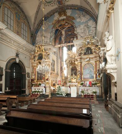 Zdjęcie nr 34: Kościół położony na południe od rynku, na placu otoczonym kamiennym murem z dwiema bramkami od zachodu i północy oraz bramką od południa. Kościół jednonawowy, dwuprzęsłowy, z węższym, niższym dwuprzęsłowym prezbiterium zamkniętym pięciobocznie. Do prezbiterium przylegają dwa aneksy, od północy dawna zakrystia (obecnie kaplica świętych Męczennic), zamknięta od wschodu dwubocznie, mająca w narożu z korpusem wieżyczkę schodową, a od południa zakrystia nowa, na planie prostokąta. Do nawy przylegają dwie kaplice: od północy kaplica Lubomirskich, założona na rzucie kwadratu, nakryta kopułą, a od południa kaplica Branickich, także na rzucie kwadratu z kopułą. Przy korpusie od zachodu piętrowa kruchta, pierwotnie otwarta w przyziemiu od północy, zachodu i południa ostrołukowymi arkadami. Arkada tęczy ostrołukowa. Sklepienie prezbiterium, zakrystii i obu kondygnacjach kruchty krzyżowo-żebrowe, w korpusie, pierwotnie trójprzęsłowym, pierwotnie sklepienie o polach trójkątnych z trójpromieniem, wsparte na dwóch dziesięciobocznych filarach, obecnie kolebkowo z lunetami. Żebra w prezbiterium i zakrystii o profilu żłobkowym, w kruchcie - gruszkowym. W prezbiterium służki cylindryczne, nadwieszone na oplecionych liśćmi wspornikach oraz rzeźbione zworniki z przedstawieniem Głowy Chrystusa i motywami roślinnymi. Ściany rozczłonkowane wykonanymi w czarnego marmuru arkadami, zamkniętymi łukiem półkolistymi. Okna ostrołukowe , obustronnie rozglifione z krzyżowym laskowaniem, w ścianie północnym prezbiterium ślepe. Kościół opięty przyporami. Elewacje na cokole, z profilowanymi gzymsami cokołowymi, kapnikowym i koronującym. Szczyty zwieńczone kwiatonami, z których zachodnie z krzyżem. Portale kamienne, ostrołukowe: zachodni profilowany, z ażurowym maswerkiem; drugi w prezbiterium do zakrystii, profilowany; trzeci do wieżyczki schodowej.