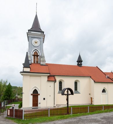 Zdjęcie nr 7: Kościół murowany, tynkowany, jednonawowy. Prezbiterium prostokątne, zamknięte prosto, z obu stron przy nawie prostokątne, piętrowe lokalności (zakrystia i skarbiec, empory). Nawa szersza od prezbiterium, na rzucie prostokąta, od frontu przylega wieża na planie kwadratu z dwoma aneksami po bokach. Prezbiterium dwuprzęsłowe, podzielone wewnątrz pilastrami, sklepione żagielkowo na gurtach. Empory flankowane parami półkolumienek, z oknami w formie leżącego prostokąta zamkniętego łukiem odcinkowym, nad lewą herb Odrowąż z inicjałami „JG”. Nawa nakryta pozornym, spłaszczonym sklepieniem kolebkowym. Otwór tęczowy w formie półkolistej arkady wspartej na pilastrach, z belką o fantazyjnym kształcie. Chór muzyczny dwukondygnacyjny, wsparty na dwóch filarach i dwóch półfilarach, pomiędzy którymi arkady ostrołukowe, kondygnacja zamknięta profilowanym gzymsem. Druga kondygnacja z trzema arkadami, w środkowej organ z wklęsło-wypukłą, ażurową balustradą. Posadzka z płyt ceramicznych. 
Fasada trójosiowa, dwukondygnacyjna. Pierwsza kondygnacja wydzielona pilastrami dekorowanymi blendami, zwieńczona profilowanym gzymsem z fryzem arkadkowym. Nad pilastrami osi bocznych dwie stylizowane wieżyczki, zakończone krzyżami. 
Na każdej osi ostrołukowe arkady, w środkowej wejście, dwie boczne wypełnione stylizowanymi blendami; nad nimi otwory okienne. Na osi środkowej, w drugiej kondygnacji wieża, ujęta w narożach czterema wieżyczkami, ścianki flankowane lizenami, zakończona profilowanym gzymsem z kostkowaniem. Na ściankach z czterech stron tarcze zegarowe oraz otwory dzwonne w formie ostrołukowych arkad w opaskach tynkowych. Wieża nakryta dachem ostrosłupowym. 
Elewacje gładkie, tynkowane zakończone profilowanym gzymsem. Wyodrębnione aneksy elewacji bocznych ujęte grubymi lizenami, z ostrołukowymi arkadami w polu, ujętymi opaskami tynkowymi. Od strony fasady w partiach aneksów bocznych wejścia do kościoła, od strony prezbiterium ostrołukowe okienka. Na każdej elewacji bocznej po trzy okna w formie stojącego prostokąta zamkniętego łukiem półkolistym, o szerokich rozglifieniach, po dwa w nawie i jednym w prezbiterium. Elewacja zamykająca prezbiterium trójosiowa, wydzielona lizenami, z głębokimi wnękami w formie stojącego prostokąta zamkniętego łukiem półkolistym, z namalowanym wizerunkiem Ukrzyżowanego Chrystusa i dwóch łotrów na krzyżach. Elewacja zakończona profilowanym gzymsem, z daszkiem pulpitowym oraz trójkątnym szczytem z czterema cokołami. Nawa i prezbiterium nakryte osobnymi  dachami dwuspadowymi. Na połączeniu nawy i aneksów przy prezbiterium wieżyczka na sygnaturkę z latarnią, nakryta dachem ostrosłupowym. 


