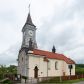 Zdjęcie nr 1: Kościół murowany, tynkowany, jednonawowy. Prezbiterium prostokątne, zamknięte prosto, z obu stron przy nawie prostokątne, piętrowe lokalności (zakrystia i skarbiec, empory). Nawa szersza od prezbiterium, na rzucie prostokąta, od frontu przylega wieża na planie kwadratu z dwoma aneksami po bokach. Prezbiterium dwuprzęsłowe, podzielone wewnątrz pilastrami, sklepione żagielkowo na gurtach. Empory flankowane parami półkolumienek, z oknami w formie leżącego prostokąta zamkniętego łukiem odcinkowym, nad lewą herb Odrowąż z inicjałami „JG”. Nawa nakryta pozornym, spłaszczonym sklepieniem kolebkowym. Otwór tęczowy w formie półkolistej arkady wspartej na pilastrach, z belką o fantazyjnym kształcie. Chór muzyczny dwukondygnacyjny, wsparty na dwóch filarach i dwóch półfilarach, pomiędzy którymi arkady ostrołukowe, kondygnacja zamknięta profilowanym gzymsem. Druga kondygnacja z trzema arkadami, w środkowej organ z wklęsło-wypukłą, ażurową balustradą. Posadzka z płyt ceramicznych. 
Fasada trójosiowa, dwukondygnacyjna. Pierwsza kondygnacja wydzielona pilastrami dekorowanymi blendami, zwieńczona profilowanym gzymsem z fryzem arkadkowym. Nad pilastrami osi bocznych dwie stylizowane wieżyczki, zakończone krzyżami. 
Na każdej osi ostrołukowe arkady, w środkowej wejście, dwie boczne wypełnione stylizowanymi blendami; nad nimi otwory okienne. Na osi środkowej, w drugiej kondygnacji wieża, ujęta w narożach czterema wieżyczkami, ścianki flankowane lizenami, zakończona profilowanym gzymsem z kostkowaniem. Na ściankach z czterech stron tarcze zegarowe oraz otwory dzwonne w formie ostrołukowych arkad w opaskach tynkowych. Wieża nakryta dachem ostrosłupowym. 
Elewacje gładkie, tynkowane zakończone profilowanym gzymsem. Wyodrębnione aneksy elewacji bocznych ujęte grubymi lizenami, z ostrołukowymi arkadami w polu, ujętymi opaskami tynkowymi. Od strony fasady w partiach aneksów bocznych wejścia do kościoła, od strony prezbiterium ostrołukowe okienka. Na każdej elewacji bocznej po trzy okna w formie stojącego prostokąta zamkniętego łukiem półkolistym, o szerokich rozglifieniach, po dwa w nawie i jednym w prezbiterium. Elewacja zamykająca prezbiterium trójosiowa, wydzielona lizenami, z głębokimi wnękami w formie stojącego prostokąta zamkniętego łukiem półkolistym, z namalowanym wizerunkiem Ukrzyżowanego Chrystusa i dwóch łotrów na krzyżach. Elewacja zakończona profilowanym gzymsem, z daszkiem pulpitowym oraz trójkątnym szczytem z czterema cokołami. Nawa i prezbiterium nakryte osobnymi  dachami dwuspadowymi. Na połączeniu nawy i aneksów przy prezbiterium wieżyczka na sygnaturkę z latarnią, nakryta dachem ostrosłupowym. 


