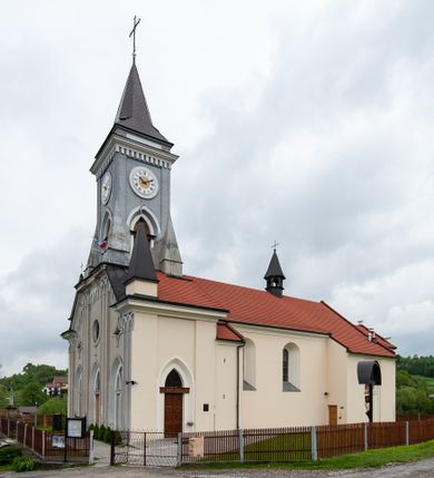 Zdjęcie nr 1: Kościół murowany, tynkowany, jednonawowy. Prezbiterium prostokątne, zamknięte prosto, z obu stron przy nawie prostokątne, piętrowe lokalności (zakrystia i skarbiec, empory). Nawa szersza od prezbiterium, na rzucie prostokąta, od frontu przylega wieża na planie kwadratu z dwoma aneksami po bokach. Prezbiterium dwuprzęsłowe, podzielone wewnątrz pilastrami, sklepione żagielkowo na gurtach. Empory flankowane parami półkolumienek, z oknami w formie leżącego prostokąta zamkniętego łukiem odcinkowym, nad lewą herb Odrowąż z inicjałami „JG”. Nawa nakryta pozornym, spłaszczonym sklepieniem kolebkowym. Otwór tęczowy w formie półkolistej arkady wspartej na pilastrach, z belką o fantazyjnym kształcie. Chór muzyczny dwukondygnacyjny, wsparty na dwóch filarach i dwóch półfilarach, pomiędzy którymi arkady ostrołukowe, kondygnacja zamknięta profilowanym gzymsem. Druga kondygnacja z trzema arkadami, w środkowej organ z wklęsło-wypukłą, ażurową balustradą. Posadzka z płyt ceramicznych. 
Fasada trójosiowa, dwukondygnacyjna. Pierwsza kondygnacja wydzielona pilastrami dekorowanymi blendami, zwieńczona profilowanym gzymsem z fryzem arkadkowym. Nad pilastrami osi bocznych dwie stylizowane wieżyczki, zakończone krzyżami. 
Na każdej osi ostrołukowe arkady, w środkowej wejście, dwie boczne wypełnione stylizowanymi blendami; nad nimi otwory okienne. Na osi środkowej, w drugiej kondygnacji wieża, ujęta w narożach czterema wieżyczkami, ścianki flankowane lizenami, zakończona profilowanym gzymsem z kostkowaniem. Na ściankach z czterech stron tarcze zegarowe oraz otwory dzwonne w formie ostrołukowych arkad w opaskach tynkowych. Wieża nakryta dachem ostrosłupowym. 
Elewacje gładkie, tynkowane zakończone profilowanym gzymsem. Wyodrębnione aneksy elewacji bocznych ujęte grubymi lizenami, z ostrołukowymi arkadami w polu, ujętymi opaskami tynkowymi. Od strony fasady w partiach aneksów bocznych wejścia do kościoła, od strony prezbiterium ostrołukowe okienka. Na każdej elewacji bocznej po trzy okna w formie stojącego prostokąta zamkniętego łukiem półkolistym, o szerokich rozglifieniach, po dwa w nawie i jednym w prezbiterium. Elewacja zamykająca prezbiterium trójosiowa, wydzielona lizenami, z głębokimi wnękami w formie stojącego prostokąta zamkniętego łukiem półkolistym, z namalowanym wizerunkiem Ukrzyżowanego Chrystusa i dwóch łotrów na krzyżach. Elewacja zakończona profilowanym gzymsem, z daszkiem pulpitowym oraz trójkątnym szczytem z czterema cokołami. Nawa i prezbiterium nakryte osobnymi  dachami dwuspadowymi. Na połączeniu nawy i aneksów przy prezbiterium wieżyczka na sygnaturkę z latarnią, nakryta dachem ostrosłupowym. 


