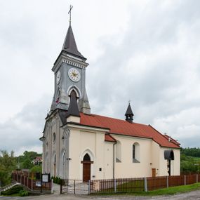 Zdjęcie nr 1: Kościół murowany, tynkowany, jednonawowy. Prezbiterium prostokątne, zamknięte prosto, z obu stron przy nawie prostokątne, piętrowe lokalności (zakrystia i skarbiec, empory). Nawa szersza od prezbiterium, na rzucie prostokąta, od frontu przylega wieża na planie kwadratu z dwoma aneksami po bokach. Prezbiterium dwuprzęsłowe, podzielone wewnątrz pilastrami, sklepione żagielkowo na gurtach. Empory flankowane parami półkolumienek, z oknami w formie leżącego prostokąta zamkniętego łukiem odcinkowym, nad lewą herb Odrowąż z inicjałami „JG”. Nawa nakryta pozornym, spłaszczonym sklepieniem kolebkowym. Otwór tęczowy w formie półkolistej arkady wspartej na pilastrach, z belką o fantazyjnym kształcie. Chór muzyczny dwukondygnacyjny, wsparty na dwóch filarach i dwóch półfilarach, pomiędzy którymi arkady ostrołukowe, kondygnacja zamknięta profilowanym gzymsem. Druga kondygnacja z trzema arkadami, w środkowej organ z wklęsło-wypukłą, ażurową balustradą. Posadzka z płyt ceramicznych. 
Fasada trójosiowa, dwukondygnacyjna. Pierwsza kondygnacja wydzielona pilastrami dekorowanymi blendami, zwieńczona profilowanym gzymsem z fryzem arkadkowym. Nad pilastrami osi bocznych dwie stylizowane wieżyczki, zakończone krzyżami. 
Na każdej osi ostrołukowe arkady, w środkowej wejście, dwie boczne wypełnione stylizowanymi blendami; nad nimi otwory okienne. Na osi środkowej, w drugiej kondygnacji wieża, ujęta w narożach czterema wieżyczkami, ścianki flankowane lizenami, zakończona profilowanym gzymsem z kostkowaniem. Na ściankach z czterech stron tarcze zegarowe oraz otwory dzwonne w formie ostrołukowych arkad w opaskach tynkowych. Wieża nakryta dachem ostrosłupowym. 
Elewacje gładkie, tynkowane zakończone profilowanym gzymsem. Wyodrębnione aneksy elewacji bocznych ujęte grubymi lizenami, z ostrołukowymi arkadami w polu, ujętymi opaskami tynkowymi. Od strony fasady w partiach aneksów bocznych wejścia do kościoła, od strony prezbiterium ostrołukowe okienka. Na każdej elewacji bocznej po trzy okna w formie stojącego prostokąta zamkniętego łukiem półkolistym, o szerokich rozglifieniach, po dwa w nawie i jednym w prezbiterium. Elewacja zamykająca prezbiterium trójosiowa, wydzielona lizenami, z głębokimi wnękami w formie stojącego prostokąta zamkniętego łukiem półkolistym, z namalowanym wizerunkiem Ukrzyżowanego Chrystusa i dwóch łotrów na krzyżach. Elewacja zakończona profilowanym gzymsem, z daszkiem pulpitowym oraz trójkątnym szczytem z czterema cokołami. Nawa i prezbiterium nakryte osobnymi  dachami dwuspadowymi. Na połączeniu nawy i aneksów przy prezbiterium wieżyczka na sygnaturkę z latarnią, nakryta dachem ostrosłupowym. 


