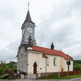 Zdjęcie nr 1: Kościół murowany, tynkowany, jednonawowy. Prezbiterium prostokątne, zamknięte prosto, z obu stron przy nawie prostokątne, piętrowe lokalności (zakrystia i skarbiec, empory). Nawa szersza od prezbiterium, na rzucie prostokąta, od frontu przylega wieża na planie kwadratu z dwoma aneksami po bokach. Prezbiterium dwuprzęsłowe, podzielone wewnątrz pilastrami, sklepione żagielkowo na gurtach. Empory flankowane parami półkolumienek, z oknami w formie leżącego prostokąta zamkniętego łukiem odcinkowym, nad lewą herb Odrowąż z inicjałami „JG”. Nawa nakryta pozornym, spłaszczonym sklepieniem kolebkowym. Otwór tęczowy w formie półkolistej arkady wspartej na pilastrach, z belką o fantazyjnym kształcie. Chór muzyczny dwukondygnacyjny, wsparty na dwóch filarach i dwóch półfilarach, pomiędzy którymi arkady ostrołukowe, kondygnacja zamknięta profilowanym gzymsem. Druga kondygnacja z trzema arkadami, w środkowej organ z wklęsło-wypukłą, ażurową balustradą. Posadzka z płyt ceramicznych. 
Fasada trójosiowa, dwukondygnacyjna. Pierwsza kondygnacja wydzielona pilastrami dekorowanymi blendami, zwieńczona profilowanym gzymsem z fryzem arkadkowym. Nad pilastrami osi bocznych dwie stylizowane wieżyczki, zakończone krzyżami. 
Na każdej osi ostrołukowe arkady, w środkowej wejście, dwie boczne wypełnione stylizowanymi blendami; nad nimi otwory okienne. Na osi środkowej, w drugiej kondygnacji wieża, ujęta w narożach czterema wieżyczkami, ścianki flankowane lizenami, zakończona profilowanym gzymsem z kostkowaniem. Na ściankach z czterech stron tarcze zegarowe oraz otwory dzwonne w formie ostrołukowych arkad w opaskach tynkowych. Wieża nakryta dachem ostrosłupowym. 
Elewacje gładkie, tynkowane zakończone profilowanym gzymsem. Wyodrębnione aneksy elewacji bocznych ujęte grubymi lizenami, z ostrołukowymi arkadami w polu, ujętymi opaskami tynkowymi. Od strony fasady w partiach aneksów bocznych wejścia do kościoła, od strony prezbiterium ostrołukowe okienka. Na każdej elewacji bocznej po trzy okna w formie stojącego prostokąta zamkniętego łukiem półkolistym, o szerokich rozglifieniach, po dwa w nawie i jednym w prezbiterium. Elewacja zamykająca prezbiterium trójosiowa, wydzielona lizenami, z głębokimi wnękami w formie stojącego prostokąta zamkniętego łukiem półkolistym, z namalowanym wizerunkiem Ukrzyżowanego Chrystusa i dwóch łotrów na krzyżach. Elewacja zakończona profilowanym gzymsem, z daszkiem pulpitowym oraz trójkątnym szczytem z czterema cokołami. Nawa i prezbiterium nakryte osobnymi  dachami dwuspadowymi. Na połączeniu nawy i aneksów przy prezbiterium wieżyczka na sygnaturkę z latarnią, nakryta dachem ostrosłupowym. 


