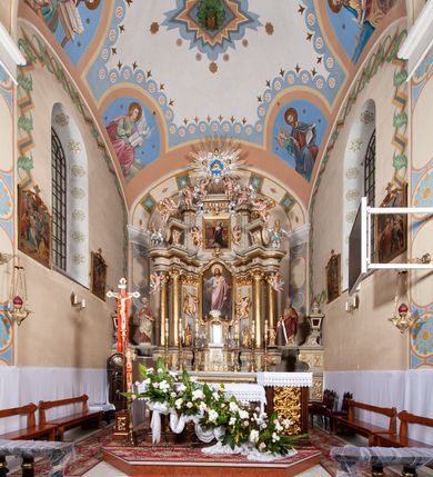 Zdjęcie nr 22: Kościół murowany, tynkowany, jednonawowy. Prezbiterium prostokątne, zamknięte prosto, z obu stron przy nawie prostokątne, piętrowe lokalności (zakrystia i skarbiec, empory). Nawa szersza od prezbiterium, na rzucie prostokąta, od frontu przylega wieża na planie kwadratu z dwoma aneksami po bokach. Prezbiterium dwuprzęsłowe, podzielone wewnątrz pilastrami, sklepione żagielkowo na gurtach. Empory flankowane parami półkolumienek, z oknami w formie leżącego prostokąta zamkniętego łukiem odcinkowym, nad lewą herb Odrowąż z inicjałami „JG”. Nawa nakryta pozornym, spłaszczonym sklepieniem kolebkowym. Otwór tęczowy w formie półkolistej arkady wspartej na pilastrach, z belką o fantazyjnym kształcie. Chór muzyczny dwukondygnacyjny, wsparty na dwóch filarach i dwóch półfilarach, pomiędzy którymi arkady ostrołukowe, kondygnacja zamknięta profilowanym gzymsem. Druga kondygnacja z trzema arkadami, w środkowej organ z wklęsło-wypukłą, ażurową balustradą. Posadzka z płyt ceramicznych. 
Fasada trójosiowa, dwukondygnacyjna. Pierwsza kondygnacja wydzielona pilastrami dekorowanymi blendami, zwieńczona profilowanym gzymsem z fryzem arkadkowym. Nad pilastrami osi bocznych dwie stylizowane wieżyczki, zakończone krzyżami. 
Na każdej osi ostrołukowe arkady, w środkowej wejście, dwie boczne wypełnione stylizowanymi blendami; nad nimi otwory okienne. Na osi środkowej, w drugiej kondygnacji wieża, ujęta w narożach czterema wieżyczkami, ścianki flankowane lizenami, zakończona profilowanym gzymsem z kostkowaniem. Na ściankach z czterech stron tarcze zegarowe oraz otwory dzwonne w formie ostrołukowych arkad w opaskach tynkowych. Wieża nakryta dachem ostrosłupowym. 
Elewacje gładkie, tynkowane zakończone profilowanym gzymsem. Wyodrębnione aneksy elewacji bocznych ujęte grubymi lizenami, z ostrołukowymi arkadami w polu, ujętymi opaskami tynkowymi. Od strony fasady w partiach aneksów bocznych wejścia do kościoła, od strony prezbiterium ostrołukowe okienka. Na każdej elewacji bocznej po trzy okna w formie stojącego prostokąta zamkniętego łukiem półkolistym, o szerokich rozglifieniach, po dwa w nawie i jednym w prezbiterium. Elewacja zamykająca prezbiterium trójosiowa, wydzielona lizenami, z głębokimi wnękami w formie stojącego prostokąta zamkniętego łukiem półkolistym, z namalowanym wizerunkiem Ukrzyżowanego Chrystusa i dwóch łotrów na krzyżach. Elewacja zakończona profilowanym gzymsem, z daszkiem pulpitowym oraz trójkątnym szczytem z czterema cokołami. Nawa i prezbiterium nakryte osobnymi  dachami dwuspadowymi. Na połączeniu nawy i aneksów przy prezbiterium wieżyczka na sygnaturkę z latarnią, nakryta dachem ostrosłupowym. 


