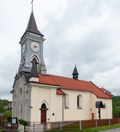 Zdjęcie nr 9: Kościół murowany, tynkowany, jednonawowy. Prezbiterium prostokątne, zamknięte prosto, z obu stron przy nawie prostokątne, piętrowe lokalności (zakrystia i skarbiec, empory). Nawa szersza od prezbiterium, na rzucie prostokąta, od frontu przylega wieża na planie kwadratu z dwoma aneksami po bokach. Prezbiterium dwuprzęsłowe, podzielone wewnątrz pilastrami, sklepione żagielkowo na gurtach. Empory flankowane parami półkolumienek, z oknami w formie leżącego prostokąta zamkniętego łukiem odcinkowym, nad lewą herb Odrowąż z inicjałami „JG”. Nawa nakryta pozornym, spłaszczonym sklepieniem kolebkowym. Otwór tęczowy w formie półkolistej arkady wspartej na pilastrach, z belką o fantazyjnym kształcie. Chór muzyczny dwukondygnacyjny, wsparty na dwóch filarach i dwóch półfilarach, pomiędzy którymi arkady ostrołukowe, kondygnacja zamknięta profilowanym gzymsem. Druga kondygnacja z trzema arkadami, w środkowej organ z wklęsło-wypukłą, ażurową balustradą. Posadzka z płyt ceramicznych. 
Fasada trójosiowa, dwukondygnacyjna. Pierwsza kondygnacja wydzielona pilastrami dekorowanymi blendami, zwieńczona profilowanym gzymsem z fryzem arkadkowym. Nad pilastrami osi bocznych dwie stylizowane wieżyczki, zakończone krzyżami. 
Na każdej osi ostrołukowe arkady, w środkowej wejście, dwie boczne wypełnione stylizowanymi blendami; nad nimi otwory okienne. Na osi środkowej, w drugiej kondygnacji wieża, ujęta w narożach czterema wieżyczkami, ścianki flankowane lizenami, zakończona profilowanym gzymsem z kostkowaniem. Na ściankach z czterech stron tarcze zegarowe oraz otwory dzwonne w formie ostrołukowych arkad w opaskach tynkowych. Wieża nakryta dachem ostrosłupowym. 
Elewacje gładkie, tynkowane zakończone profilowanym gzymsem. Wyodrębnione aneksy elewacji bocznych ujęte grubymi lizenami, z ostrołukowymi arkadami w polu, ujętymi opaskami tynkowymi. Od strony fasady w partiach aneksów bocznych wejścia do kościoła, od strony prezbiterium ostrołukowe okienka. Na każdej elewacji bocznej po trzy okna w formie stojącego prostokąta zamkniętego łukiem półkolistym, o szerokich rozglifieniach, po dwa w nawie i jednym w prezbiterium. Elewacja zamykająca prezbiterium trójosiowa, wydzielona lizenami, z głębokimi wnękami w formie stojącego prostokąta zamkniętego łukiem półkolistym, z namalowanym wizerunkiem Ukrzyżowanego Chrystusa i dwóch łotrów na krzyżach. Elewacja zakończona profilowanym gzymsem, z daszkiem pulpitowym oraz trójkątnym szczytem z czterema cokołami. Nawa i prezbiterium nakryte osobnymi  dachami dwuspadowymi. Na połączeniu nawy i aneksów przy prezbiterium wieżyczka na sygnaturkę z latarnią, nakryta dachem ostrosłupowym. 


