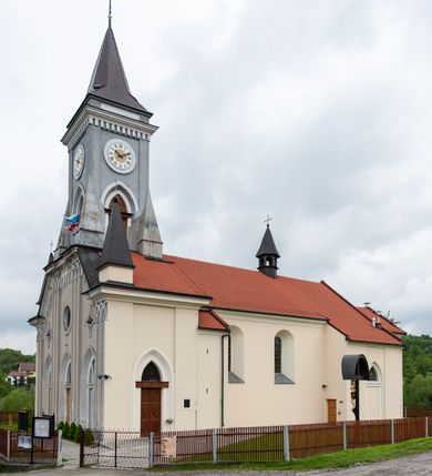 Zdjęcie nr 10: Kościół murowany, tynkowany, jednonawowy. Prezbiterium prostokątne, zamknięte prosto, z obu stron przy nawie prostokątne, piętrowe lokalności (zakrystia i skarbiec, empory). Nawa szersza od prezbiterium, na rzucie prostokąta, od frontu przylega wieża na planie kwadratu z dwoma aneksami po bokach. Prezbiterium dwuprzęsłowe, podzielone wewnątrz pilastrami, sklepione żagielkowo na gurtach. Empory flankowane parami półkolumienek, z oknami w formie leżącego prostokąta zamkniętego łukiem odcinkowym, nad lewą herb Odrowąż z inicjałami „JG”. Nawa nakryta pozornym, spłaszczonym sklepieniem kolebkowym. Otwór tęczowy w formie półkolistej arkady wspartej na pilastrach, z belką o fantazyjnym kształcie. Chór muzyczny dwukondygnacyjny, wsparty na dwóch filarach i dwóch półfilarach, pomiędzy którymi arkady ostrołukowe, kondygnacja zamknięta profilowanym gzymsem. Druga kondygnacja z trzema arkadami, w środkowej organ z wklęsło-wypukłą, ażurową balustradą. Posadzka z płyt ceramicznych. 
Fasada trójosiowa, dwukondygnacyjna. Pierwsza kondygnacja wydzielona pilastrami dekorowanymi blendami, zwieńczona profilowanym gzymsem z fryzem arkadkowym. Nad pilastrami osi bocznych dwie stylizowane wieżyczki, zakończone krzyżami. 
Na każdej osi ostrołukowe arkady, w środkowej wejście, dwie boczne wypełnione stylizowanymi blendami; nad nimi otwory okienne. Na osi środkowej, w drugiej kondygnacji wieża, ujęta w narożach czterema wieżyczkami, ścianki flankowane lizenami, zakończona profilowanym gzymsem z kostkowaniem. Na ściankach z czterech stron tarcze zegarowe oraz otwory dzwonne w formie ostrołukowych arkad w opaskach tynkowych. Wieża nakryta dachem ostrosłupowym. 
Elewacje gładkie, tynkowane zakończone profilowanym gzymsem. Wyodrębnione aneksy elewacji bocznych ujęte grubymi lizenami, z ostrołukowymi arkadami w polu, ujętymi opaskami tynkowymi. Od strony fasady w partiach aneksów bocznych wejścia do kościoła, od strony prezbiterium ostrołukowe okienka. Na każdej elewacji bocznej po trzy okna w formie stojącego prostokąta zamkniętego łukiem półkolistym, o szerokich rozglifieniach, po dwa w nawie i jednym w prezbiterium. Elewacja zamykająca prezbiterium trójosiowa, wydzielona lizenami, z głębokimi wnękami w formie stojącego prostokąta zamkniętego łukiem półkolistym, z namalowanym wizerunkiem Ukrzyżowanego Chrystusa i dwóch łotrów na krzyżach. Elewacja zakończona profilowanym gzymsem, z daszkiem pulpitowym oraz trójkątnym szczytem z czterema cokołami. Nawa i prezbiterium nakryte osobnymi  dachami dwuspadowymi. Na połączeniu nawy i aneksów przy prezbiterium wieżyczka na sygnaturkę z latarnią, nakryta dachem ostrosłupowym. 


