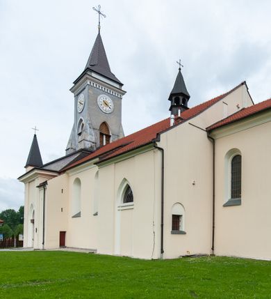 Zdjęcie nr 13: Kościół murowany, tynkowany, jednonawowy. Prezbiterium prostokątne, zamknięte prosto, z obu stron przy nawie prostokątne, piętrowe lokalności (zakrystia i skarbiec, empory). Nawa szersza od prezbiterium, na rzucie prostokąta, od frontu przylega wieża na planie kwadratu z dwoma aneksami po bokach. Prezbiterium dwuprzęsłowe, podzielone wewnątrz pilastrami, sklepione żagielkowo na gurtach. Empory flankowane parami półkolumienek, z oknami w formie leżącego prostokąta zamkniętego łukiem odcinkowym, nad lewą herb Odrowąż z inicjałami „JG”. Nawa nakryta pozornym, spłaszczonym sklepieniem kolebkowym. Otwór tęczowy w formie półkolistej arkady wspartej na pilastrach, z belką o fantazyjnym kształcie. Chór muzyczny dwukondygnacyjny, wsparty na dwóch filarach i dwóch półfilarach, pomiędzy którymi arkady ostrołukowe, kondygnacja zamknięta profilowanym gzymsem. Druga kondygnacja z trzema arkadami, w środkowej organ z wklęsło-wypukłą, ażurową balustradą. Posadzka z płyt ceramicznych. 
Fasada trójosiowa, dwukondygnacyjna. Pierwsza kondygnacja wydzielona pilastrami dekorowanymi blendami, zwieńczona profilowanym gzymsem z fryzem arkadkowym. Nad pilastrami osi bocznych dwie stylizowane wieżyczki, zakończone krzyżami. 
Na każdej osi ostrołukowe arkady, w środkowej wejście, dwie boczne wypełnione stylizowanymi blendami; nad nimi otwory okienne. Na osi środkowej, w drugiej kondygnacji wieża, ujęta w narożach czterema wieżyczkami, ścianki flankowane lizenami, zakończona profilowanym gzymsem z kostkowaniem. Na ściankach z czterech stron tarcze zegarowe oraz otwory dzwonne w formie ostrołukowych arkad w opaskach tynkowych. Wieża nakryta dachem ostrosłupowym. 
Elewacje gładkie, tynkowane zakończone profilowanym gzymsem. Wyodrębnione aneksy elewacji bocznych ujęte grubymi lizenami, z ostrołukowymi arkadami w polu, ujętymi opaskami tynkowymi. Od strony fasady w partiach aneksów bocznych wejścia do kościoła, od strony prezbiterium ostrołukowe okienka. Na każdej elewacji bocznej po trzy okna w formie stojącego prostokąta zamkniętego łukiem półkolistym, o szerokich rozglifieniach, po dwa w nawie i jednym w prezbiterium. Elewacja zamykająca prezbiterium trójosiowa, wydzielona lizenami, z głębokimi wnękami w formie stojącego prostokąta zamkniętego łukiem półkolistym, z namalowanym wizerunkiem Ukrzyżowanego Chrystusa i dwóch łotrów na krzyżach. Elewacja zakończona profilowanym gzymsem, z daszkiem pulpitowym oraz trójkątnym szczytem z czterema cokołami. Nawa i prezbiterium nakryte osobnymi  dachami dwuspadowymi. Na połączeniu nawy i aneksów przy prezbiterium wieżyczka na sygnaturkę z latarnią, nakryta dachem ostrosłupowym. 


