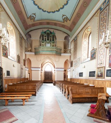 Zdjęcie nr 27: Kościół murowany, tynkowany, jednonawowy. Prezbiterium prostokątne, zamknięte prosto, z obu stron przy nawie prostokątne, piętrowe lokalności (zakrystia i skarbiec, empory). Nawa szersza od prezbiterium, na rzucie prostokąta, od frontu przylega wieża na planie kwadratu z dwoma aneksami po bokach. Prezbiterium dwuprzęsłowe, podzielone wewnątrz pilastrami, sklepione żagielkowo na gurtach. Empory flankowane parami półkolumienek, z oknami w formie leżącego prostokąta zamkniętego łukiem odcinkowym, nad lewą herb Odrowąż z inicjałami „JG”. Nawa nakryta pozornym, spłaszczonym sklepieniem kolebkowym. Otwór tęczowy w formie półkolistej arkady wspartej na pilastrach, z belką o fantazyjnym kształcie. Chór muzyczny dwukondygnacyjny, wsparty na dwóch filarach i dwóch półfilarach, pomiędzy którymi arkady ostrołukowe, kondygnacja zamknięta profilowanym gzymsem. Druga kondygnacja z trzema arkadami, w środkowej organ z wklęsło-wypukłą, ażurową balustradą. Posadzka z płyt ceramicznych. 
Fasada trójosiowa, dwukondygnacyjna. Pierwsza kondygnacja wydzielona pilastrami dekorowanymi blendami, zwieńczona profilowanym gzymsem z fryzem arkadkowym. Nad pilastrami osi bocznych dwie stylizowane wieżyczki, zakończone krzyżami. 
Na każdej osi ostrołukowe arkady, w środkowej wejście, dwie boczne wypełnione stylizowanymi blendami; nad nimi otwory okienne. Na osi środkowej, w drugiej kondygnacji wieża, ujęta w narożach czterema wieżyczkami, ścianki flankowane lizenami, zakończona profilowanym gzymsem z kostkowaniem. Na ściankach z czterech stron tarcze zegarowe oraz otwory dzwonne w formie ostrołukowych arkad w opaskach tynkowych. Wieża nakryta dachem ostrosłupowym. 
Elewacje gładkie, tynkowane zakończone profilowanym gzymsem. Wyodrębnione aneksy elewacji bocznych ujęte grubymi lizenami, z ostrołukowymi arkadami w polu, ujętymi opaskami tynkowymi. Od strony fasady w partiach aneksów bocznych wejścia do kościoła, od strony prezbiterium ostrołukowe okienka. Na każdej elewacji bocznej po trzy okna w formie stojącego prostokąta zamkniętego łukiem półkolistym, o szerokich rozglifieniach, po dwa w nawie i jednym w prezbiterium. Elewacja zamykająca prezbiterium trójosiowa, wydzielona lizenami, z głębokimi wnękami w formie stojącego prostokąta zamkniętego łukiem półkolistym, z namalowanym wizerunkiem Ukrzyżowanego Chrystusa i dwóch łotrów na krzyżach. Elewacja zakończona profilowanym gzymsem, z daszkiem pulpitowym oraz trójkątnym szczytem z czterema cokołami. Nawa i prezbiterium nakryte osobnymi  dachami dwuspadowymi. Na połączeniu nawy i aneksów przy prezbiterium wieżyczka na sygnaturkę z latarnią, nakryta dachem ostrosłupowym. 


