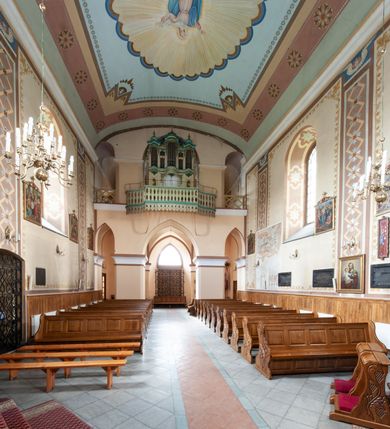 Zdjęcie nr 31: Kościół murowany, tynkowany, jednonawowy. Prezbiterium prostokątne, zamknięte prosto, z obu stron przy nawie prostokątne, piętrowe lokalności (zakrystia i skarbiec, empory). Nawa szersza od prezbiterium, na rzucie prostokąta, od frontu przylega wieża na planie kwadratu z dwoma aneksami po bokach. Prezbiterium dwuprzęsłowe, podzielone wewnątrz pilastrami, sklepione żagielkowo na gurtach. Empory flankowane parami półkolumienek, z oknami w formie leżącego prostokąta zamkniętego łukiem odcinkowym, nad lewą herb Odrowąż z inicjałami „JG”. Nawa nakryta pozornym, spłaszczonym sklepieniem kolebkowym. Otwór tęczowy w formie półkolistej arkady wspartej na pilastrach, z belką o fantazyjnym kształcie. Chór muzyczny dwukondygnacyjny, wsparty na dwóch filarach i dwóch półfilarach, pomiędzy którymi arkady ostrołukowe, kondygnacja zamknięta profilowanym gzymsem. Druga kondygnacja z trzema arkadami, w środkowej organ z wklęsło-wypukłą, ażurową balustradą. Posadzka z płyt ceramicznych. 
Fasada trójosiowa, dwukondygnacyjna. Pierwsza kondygnacja wydzielona pilastrami dekorowanymi blendami, zwieńczona profilowanym gzymsem z fryzem arkadkowym. Nad pilastrami osi bocznych dwie stylizowane wieżyczki, zakończone krzyżami. 
Na każdej osi ostrołukowe arkady, w środkowej wejście, dwie boczne wypełnione stylizowanymi blendami; nad nimi otwory okienne. Na osi środkowej, w drugiej kondygnacji wieża, ujęta w narożach czterema wieżyczkami, ścianki flankowane lizenami, zakończona profilowanym gzymsem z kostkowaniem. Na ściankach z czterech stron tarcze zegarowe oraz otwory dzwonne w formie ostrołukowych arkad w opaskach tynkowych. Wieża nakryta dachem ostrosłupowym. 
Elewacje gładkie, tynkowane zakończone profilowanym gzymsem. Wyodrębnione aneksy elewacji bocznych ujęte grubymi lizenami, z ostrołukowymi arkadami w polu, ujętymi opaskami tynkowymi. Od strony fasady w partiach aneksów bocznych wejścia do kościoła, od strony prezbiterium ostrołukowe okienka. Na każdej elewacji bocznej po trzy okna w formie stojącego prostokąta zamkniętego łukiem półkolistym, o szerokich rozglifieniach, po dwa w nawie i jednym w prezbiterium. Elewacja zamykająca prezbiterium trójosiowa, wydzielona lizenami, z głębokimi wnękami w formie stojącego prostokąta zamkniętego łukiem półkolistym, z namalowanym wizerunkiem Ukrzyżowanego Chrystusa i dwóch łotrów na krzyżach. Elewacja zakończona profilowanym gzymsem, z daszkiem pulpitowym oraz trójkątnym szczytem z czterema cokołami. Nawa i prezbiterium nakryte osobnymi  dachami dwuspadowymi. Na połączeniu nawy i aneksów przy prezbiterium wieżyczka na sygnaturkę z latarnią, nakryta dachem ostrosłupowym. 


