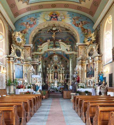 Zdjęcie nr 25: Kościół murowany, tynkowany, jednonawowy. Prezbiterium prostokątne, zamknięte prosto, z obu stron przy nawie prostokątne, piętrowe lokalności (zakrystia i skarbiec, empory). Nawa szersza od prezbiterium, na rzucie prostokąta, od frontu przylega wieża na planie kwadratu z dwoma aneksami po bokach. Prezbiterium dwuprzęsłowe, podzielone wewnątrz pilastrami, sklepione żagielkowo na gurtach. Empory flankowane parami półkolumienek, z oknami w formie leżącego prostokąta zamkniętego łukiem odcinkowym, nad lewą herb Odrowąż z inicjałami „JG”. Nawa nakryta pozornym, spłaszczonym sklepieniem kolebkowym. Otwór tęczowy w formie półkolistej arkady wspartej na pilastrach, z belką o fantazyjnym kształcie. Chór muzyczny dwukondygnacyjny, wsparty na dwóch filarach i dwóch półfilarach, pomiędzy którymi arkady ostrołukowe, kondygnacja zamknięta profilowanym gzymsem. Druga kondygnacja z trzema arkadami, w środkowej organ z wklęsło-wypukłą, ażurową balustradą. Posadzka z płyt ceramicznych. 
Fasada trójosiowa, dwukondygnacyjna. Pierwsza kondygnacja wydzielona pilastrami dekorowanymi blendami, zwieńczona profilowanym gzymsem z fryzem arkadkowym. Nad pilastrami osi bocznych dwie stylizowane wieżyczki, zakończone krzyżami. 
Na każdej osi ostrołukowe arkady, w środkowej wejście, dwie boczne wypełnione stylizowanymi blendami; nad nimi otwory okienne. Na osi środkowej, w drugiej kondygnacji wieża, ujęta w narożach czterema wieżyczkami, ścianki flankowane lizenami, zakończona profilowanym gzymsem z kostkowaniem. Na ściankach z czterech stron tarcze zegarowe oraz otwory dzwonne w formie ostrołukowych arkad w opaskach tynkowych. Wieża nakryta dachem ostrosłupowym. 
Elewacje gładkie, tynkowane zakończone profilowanym gzymsem. Wyodrębnione aneksy elewacji bocznych ujęte grubymi lizenami, z ostrołukowymi arkadami w polu, ujętymi opaskami tynkowymi. Od strony fasady w partiach aneksów bocznych wejścia do kościoła, od strony prezbiterium ostrołukowe okienka. Na każdej elewacji bocznej po trzy okna w formie stojącego prostokąta zamkniętego łukiem półkolistym, o szerokich rozglifieniach, po dwa w nawie i jednym w prezbiterium. Elewacja zamykająca prezbiterium trójosiowa, wydzielona lizenami, z głębokimi wnękami w formie stojącego prostokąta zamkniętego łukiem półkolistym, z namalowanym wizerunkiem Ukrzyżowanego Chrystusa i dwóch łotrów na krzyżach. Elewacja zakończona profilowanym gzymsem, z daszkiem pulpitowym oraz trójkątnym szczytem z czterema cokołami. Nawa i prezbiterium nakryte osobnymi  dachami dwuspadowymi. Na połączeniu nawy i aneksów przy prezbiterium wieżyczka na sygnaturkę z latarnią, nakryta dachem ostrosłupowym. 


