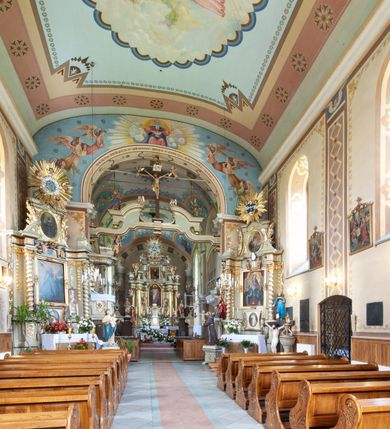 Zdjęcie nr 26: Kościół murowany, tynkowany, jednonawowy. Prezbiterium prostokątne, zamknięte prosto, z obu stron przy nawie prostokątne, piętrowe lokalności (zakrystia i skarbiec, empory). Nawa szersza od prezbiterium, na rzucie prostokąta, od frontu przylega wieża na planie kwadratu z dwoma aneksami po bokach. Prezbiterium dwuprzęsłowe, podzielone wewnątrz pilastrami, sklepione żagielkowo na gurtach. Empory flankowane parami półkolumienek, z oknami w formie leżącego prostokąta zamkniętego łukiem odcinkowym, nad lewą herb Odrowąż z inicjałami „JG”. Nawa nakryta pozornym, spłaszczonym sklepieniem kolebkowym. Otwór tęczowy w formie półkolistej arkady wspartej na pilastrach, z belką o fantazyjnym kształcie. Chór muzyczny dwukondygnacyjny, wsparty na dwóch filarach i dwóch półfilarach, pomiędzy którymi arkady ostrołukowe, kondygnacja zamknięta profilowanym gzymsem. Druga kondygnacja z trzema arkadami, w środkowej organ z wklęsło-wypukłą, ażurową balustradą. Posadzka z płyt ceramicznych. 
Fasada trójosiowa, dwukondygnacyjna. Pierwsza kondygnacja wydzielona pilastrami dekorowanymi blendami, zwieńczona profilowanym gzymsem z fryzem arkadkowym. Nad pilastrami osi bocznych dwie stylizowane wieżyczki, zakończone krzyżami. 
Na każdej osi ostrołukowe arkady, w środkowej wejście, dwie boczne wypełnione stylizowanymi blendami; nad nimi otwory okienne. Na osi środkowej, w drugiej kondygnacji wieża, ujęta w narożach czterema wieżyczkami, ścianki flankowane lizenami, zakończona profilowanym gzymsem z kostkowaniem. Na ściankach z czterech stron tarcze zegarowe oraz otwory dzwonne w formie ostrołukowych arkad w opaskach tynkowych. Wieża nakryta dachem ostrosłupowym. 
Elewacje gładkie, tynkowane zakończone profilowanym gzymsem. Wyodrębnione aneksy elewacji bocznych ujęte grubymi lizenami, z ostrołukowymi arkadami w polu, ujętymi opaskami tynkowymi. Od strony fasady w partiach aneksów bocznych wejścia do kościoła, od strony prezbiterium ostrołukowe okienka. Na każdej elewacji bocznej po trzy okna w formie stojącego prostokąta zamkniętego łukiem półkolistym, o szerokich rozglifieniach, po dwa w nawie i jednym w prezbiterium. Elewacja zamykająca prezbiterium trójosiowa, wydzielona lizenami, z głębokimi wnękami w formie stojącego prostokąta zamkniętego łukiem półkolistym, z namalowanym wizerunkiem Ukrzyżowanego Chrystusa i dwóch łotrów na krzyżach. Elewacja zakończona profilowanym gzymsem, z daszkiem pulpitowym oraz trójkątnym szczytem z czterema cokołami. Nawa i prezbiterium nakryte osobnymi  dachami dwuspadowymi. Na połączeniu nawy i aneksów przy prezbiterium wieżyczka na sygnaturkę z latarnią, nakryta dachem ostrosłupowym. 


