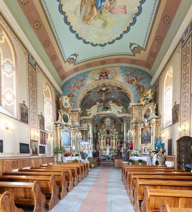 Zdjęcie nr 24: Kościół murowany, tynkowany, jednonawowy. Prezbiterium prostokątne, zamknięte prosto, z obu stron przy nawie prostokątne, piętrowe lokalności (zakrystia i skarbiec, empory). Nawa szersza od prezbiterium, na rzucie prostokąta, od frontu przylega wieża na planie kwadratu z dwoma aneksami po bokach. Prezbiterium dwuprzęsłowe, podzielone wewnątrz pilastrami, sklepione żagielkowo na gurtach. Empory flankowane parami półkolumienek, z oknami w formie leżącego prostokąta zamkniętego łukiem odcinkowym, nad lewą herb Odrowąż z inicjałami „JG”. Nawa nakryta pozornym, spłaszczonym sklepieniem kolebkowym. Otwór tęczowy w formie półkolistej arkady wspartej na pilastrach, z belką o fantazyjnym kształcie. Chór muzyczny dwukondygnacyjny, wsparty na dwóch filarach i dwóch półfilarach, pomiędzy którymi arkady ostrołukowe, kondygnacja zamknięta profilowanym gzymsem. Druga kondygnacja z trzema arkadami, w środkowej organ z wklęsło-wypukłą, ażurową balustradą. Posadzka z płyt ceramicznych. 
Fasada trójosiowa, dwukondygnacyjna. Pierwsza kondygnacja wydzielona pilastrami dekorowanymi blendami, zwieńczona profilowanym gzymsem z fryzem arkadkowym. Nad pilastrami osi bocznych dwie stylizowane wieżyczki, zakończone krzyżami. 
Na każdej osi ostrołukowe arkady, w środkowej wejście, dwie boczne wypełnione stylizowanymi blendami; nad nimi otwory okienne. Na osi środkowej, w drugiej kondygnacji wieża, ujęta w narożach czterema wieżyczkami, ścianki flankowane lizenami, zakończona profilowanym gzymsem z kostkowaniem. Na ściankach z czterech stron tarcze zegarowe oraz otwory dzwonne w formie ostrołukowych arkad w opaskach tynkowych. Wieża nakryta dachem ostrosłupowym. 
Elewacje gładkie, tynkowane zakończone profilowanym gzymsem. Wyodrębnione aneksy elewacji bocznych ujęte grubymi lizenami, z ostrołukowymi arkadami w polu, ujętymi opaskami tynkowymi. Od strony fasady w partiach aneksów bocznych wejścia do kościoła, od strony prezbiterium ostrołukowe okienka. Na każdej elewacji bocznej po trzy okna w formie stojącego prostokąta zamkniętego łukiem półkolistym, o szerokich rozglifieniach, po dwa w nawie i jednym w prezbiterium. Elewacja zamykająca prezbiterium trójosiowa, wydzielona lizenami, z głębokimi wnękami w formie stojącego prostokąta zamkniętego łukiem półkolistym, z namalowanym wizerunkiem Ukrzyżowanego Chrystusa i dwóch łotrów na krzyżach. Elewacja zakończona profilowanym gzymsem, z daszkiem pulpitowym oraz trójkątnym szczytem z czterema cokołami. Nawa i prezbiterium nakryte osobnymi  dachami dwuspadowymi. Na połączeniu nawy i aneksów przy prezbiterium wieżyczka na sygnaturkę z latarnią, nakryta dachem ostrosłupowym. 


