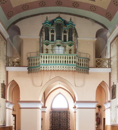 Zdjęcie nr 29: Kościół murowany, tynkowany, jednonawowy. Prezbiterium prostokątne, zamknięte prosto, z obu stron przy nawie prostokątne, piętrowe lokalności (zakrystia i skarbiec, empory). Nawa szersza od prezbiterium, na rzucie prostokąta, od frontu przylega wieża na planie kwadratu z dwoma aneksami po bokach. Prezbiterium dwuprzęsłowe, podzielone wewnątrz pilastrami, sklepione żagielkowo na gurtach. Empory flankowane parami półkolumienek, z oknami w formie leżącego prostokąta zamkniętego łukiem odcinkowym, nad lewą herb Odrowąż z inicjałami „JG”. Nawa nakryta pozornym, spłaszczonym sklepieniem kolebkowym. Otwór tęczowy w formie półkolistej arkady wspartej na pilastrach, z belką o fantazyjnym kształcie. Chór muzyczny dwukondygnacyjny, wsparty na dwóch filarach i dwóch półfilarach, pomiędzy którymi arkady ostrołukowe, kondygnacja zamknięta profilowanym gzymsem. Druga kondygnacja z trzema arkadami, w środkowej organ z wklęsło-wypukłą, ażurową balustradą. Posadzka z płyt ceramicznych. 
Fasada trójosiowa, dwukondygnacyjna. Pierwsza kondygnacja wydzielona pilastrami dekorowanymi blendami, zwieńczona profilowanym gzymsem z fryzem arkadkowym. Nad pilastrami osi bocznych dwie stylizowane wieżyczki, zakończone krzyżami. 
Na każdej osi ostrołukowe arkady, w środkowej wejście, dwie boczne wypełnione stylizowanymi blendami; nad nimi otwory okienne. Na osi środkowej, w drugiej kondygnacji wieża, ujęta w narożach czterema wieżyczkami, ścianki flankowane lizenami, zakończona profilowanym gzymsem z kostkowaniem. Na ściankach z czterech stron tarcze zegarowe oraz otwory dzwonne w formie ostrołukowych arkad w opaskach tynkowych. Wieża nakryta dachem ostrosłupowym. 
Elewacje gładkie, tynkowane zakończone profilowanym gzymsem. Wyodrębnione aneksy elewacji bocznych ujęte grubymi lizenami, z ostrołukowymi arkadami w polu, ujętymi opaskami tynkowymi. Od strony fasady w partiach aneksów bocznych wejścia do kościoła, od strony prezbiterium ostrołukowe okienka. Na każdej elewacji bocznej po trzy okna w formie stojącego prostokąta zamkniętego łukiem półkolistym, o szerokich rozglifieniach, po dwa w nawie i jednym w prezbiterium. Elewacja zamykająca prezbiterium trójosiowa, wydzielona lizenami, z głębokimi wnękami w formie stojącego prostokąta zamkniętego łukiem półkolistym, z namalowanym wizerunkiem Ukrzyżowanego Chrystusa i dwóch łotrów na krzyżach. Elewacja zakończona profilowanym gzymsem, z daszkiem pulpitowym oraz trójkątnym szczytem z czterema cokołami. Nawa i prezbiterium nakryte osobnymi  dachami dwuspadowymi. Na połączeniu nawy i aneksów przy prezbiterium wieżyczka na sygnaturkę z latarnią, nakryta dachem ostrosłupowym. 


