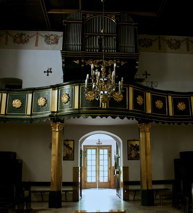 Zdjęcie nr 27: Kościół jest usytuowany w centrum wsi Rudawa, na północ od głównej drogi z Zabierzowa do Chrzanowa. Teren wokół niego jest otoczony wysokim, kamiennym murem z nieregularnych ciosów kamienia, oszkarpowanym, tynkowanym, z wyjątkiem zewnętrznej części muru na zachód od południowej bramki. W murze znajdują się trzy wejścia, od wschodu, południa i zachodu. W części wschodniej muru znajduje się trójosiowa brama wjazdowa, zwieńczona łukiem wklęsło-wypukłym, z trzema przelotami: środkowym wyższym i szerszym, zamkniętym łukiem odcinkowym i bocznymi węższymi i niższymi, zamkniętymi łukiem półkolistym (północne zamurowane). Część środkowa jest flankowana zdwojonymi pilastrami, podtrzymującymi profilowane uskokowe belkowanie z przyczółkiem o profilowanym łuku falistym, zwieńczonym równoramiennym krzyżem. W przyczółku wnęka z figurą św. Floriana. Bramki od strony zachodniej i południowej prostokątne, z przejściem zakończonym płaskim łukiem odcinkowym, z profilowanym gzymsem, zwieńczonym trójkątnym przyczółkiem. Przejścia zamykane drewnianymi ażurowymi i pomalowanymi na ciemnobrązowo jednoskrzydłowymi drzwiami. Poprzez bramkę od zachodu zejście kamiennymi schodami poprowadzonymi wzdłuż muru na dziedziniec plebański, usytuowany poniżej terenu kościelnego. 
W północno-wschodnim narożniku muru niewielka murowana i tynkowana kostnica na planie kwadratu, nakryta dachem namiotowym, łamanym, zakończonym ośmioboczną ślepą latarnią.

Po stronie południowej, poniżej placu kościelnego, do muru przylega murowana, tynkowana, prostokątna i dwukondygnacyjna „zegarowa” wieża bramna nakryta namiotowym dachem z wysoką drewnianą ośmioboczną latarnią o cebulastym hełmie. W wieży znajduje się przejazd wiodący na dziedziniec plebański, z sienią otwartą na przestrzał w dolnej kondygnacji i z lamusem dostępnym od strony placu kościelnego w górnej. 

W południowej części muru, w pobliżu południowo-wschodniego narożnika placu kościelnego, nadbudowana kamienna dzwonnica parawanowa z zawieszonymi czterema dzwonami.  

We wschodniej części placu kościelnego pomiędzy bramką wschodnią a kostnicą znajduje się kamienna ambona, o ośmiobocznej podstawie przechodzącej w szerszy, również ośmioboczny korpus, zakończony kamiennym parapetem, z kamiennymi schodami prowadzącymi na ambonę od strony wschodniej. 

Kościół jest orientowany, prawie w całości zbudowany z cegły, otynkowany z wyjątkiem prezbiterium. Wnętrze kościoła tworzy niewielkie, prostokątne, jednoprzęsłowe prezbiterium zakończone prostą ścianą i nakryte pozornym sklepieniem krzyżowo-żebrowym. Nawa jest szersza, prawie kwadratowa, nakryta drewnianym stropem. Prezbiterium z nawą są połączone szeroką, ostrołukową arkadą w ścianie tęczowej. Od północy do prezbiterium przylega założona na planie prostokąta dwuprzęsłowa zakrystia, nakryta sklepieniem krzyżowym. Wejście do zakrystii zaznaczone gotyckim, kamiennym, sfazowanym portalem zamkniętym łukiem ostrym. Od zachodu do zakrystii przylega niewielkie pomieszczenie gospodarcze, do którego z zakrystii prowadzą ostrołukowe drzwi. Zakrystia oświetlona ostrołukowym oknem w ścianie wschodniej, wypełnionym witrażem z tafelek w kształcie sześciokąta foremnego, ze szkła surowego, tzw. katedralnego. 

Od południa do nawy przylega kaplica o formach renesansowych, dwukondygnacyjna, założona na planie kwadratu. W dolnej kondygnacji sklepiona krzyżowo-żebrowo kruchta otwarta do nawy szeroką, zamkniętą półkoliście arkadą.

Ponad kruchtą kaplica św. Kazimierza, nakryta wspartą na pendentywach kopułą z latarnią. Z kruchty do kaplicy prowadzą kręte kamienne schody umieszczone od zachodu w półkolistej wieżyczce. Prostokątne wejście z krypty na klatkę schodową ujęte kamiennym profilowanym portalem. Kaplica otwarta do nawy szeroką, zamkniętą półkoliście arkadą, o kształcie i wymiarach analogicznych do arkady znajdującej się poniżej. Kaplicę, prócz latarni, oświetla prostokątne okno w ścianie południowej, wypełnione witrażem z tafelek w kształcie gomółek, ze szkła surowego, tzw. katedralnego. Na zachodniej ścianie nawy chór muzyczny, dostępny klatką schodową ukrytą w zewnętrznym aneksie przylegającym do zachodniej elewacji nawy i południowej elewacji wieży-dzwonnicy. 

Nawę i prezbiterium oświetlają umieszczone w południowych ścianach prostokątne, rozglifione okna: jedno w prezbiterium, dwa w nawie. Wszystkie wypełnione witrażami z tafelek w kształcie gomółek, ze szkła surowego, tzw. katedralnego. 

Do kościoła prowadzą dwa wejścia: poprzez arkadę z kruchty południowej oraz szerokie wejście główne prostokątne, zamknięte łukiem odcinkowym, prowadzące do kościoła z obszernej kruchty od strony zachodniej, znajdującej się w murowanym przyziemiu wieży - dzwonnicy. Kruchta, założona na planie kwadratu i nakryta murowanym stropem, doświetlona jest dwoma prostokątnymi oknami umieszczonymi naprzeciw siebie w ścianach północnej i południowej.
 
W zewnętrznej elewacji kościoła widoczny niewysoki kamienny cokół wykonany z nieregularnych ciosów kamienia. Prezbiterium, niższe od nawy, murowane z cegły w układzie wedyjskim, z domieszką układu polskiego. Wschodnie naroża prezbiterium zaakcentowane płaskimi lizenami. We wschodniej ścianie widoczny zarys zamurowanego wydłużonego okna zamkniętego lekko zaostrzonym łukiem, w trójkątnym szczycie znajduje się niewielkie wąskie okienko zakończone łukiem półkolistym. Południowa ściana prezbiterium ozdobiona fryzem z cegieł. Do ściany północnej prezbiterium przylega zakrystia, oszkarpowana, nakryta dachem pulpitowym, z dobudowanym od niej niewielkim aneksem, nakrytym takim samym zadaszeniem. Do wschodniej ściany prezbiterium przylega ogrójec nakryty dachem namiotowym z cebulastym zwieńczeniem, wspartym na sześciu smukłych, profilowanych drewnianych słupach z mieczami, pomiędzy którymi od północy i południa ażurowa drewniana balustrada. 

Nawa oszkarpowana w narożnikach. Elewacje bez podziałów architektonicznych. Od strony południowej do nawy dobudowana dwukondygnacyjna kaplica nakryta kopułą z latarnią, podzielona na dwie kondygnacje. W dolnej kondygnacji od południa wejście do kruchty zaznaczone kamiennym portalem o sfazowanych węgarach i lekko zaostrzonym łuku. Wejście zamykają drewniane dwuskrzydłowe drzwi ozdobione kratownicą z żelaznych listew. Od zachodu do kaplicy przylega półokrągła wieżyczka nakryta daszkiem stożkowym. 

Do zachodniej fasady kościoła dostawiona niska, założona na planie kwadratu trójkondygnacyjna wieża-dzwonnica: w dolnej części murowana, w narożach wzmocniona kamiennymi szkarpami, w górnej drewniana konstrukcji słupowo-ramowej z nadwieszoną izbicą i nakryta dachem półszczytowym. W dolnej, murowanej kondygnacji, na osi kościoła, prostokątne wejście do kruchty zaakcentowane przedsionkiem w kształcie ostrołukowej arkady i czterostopniowymi schodami. Przedsionek nakryty dachem dwuspadowym. Do zachodniej elewacji nawy i południowej elewacji dzwonnicy przylega niewielki, wysoki drewniany aneks, nakryty dachem pulpitowym, mieszczący klatkę schodową prowadzącą na górną kondygnację dzwonnicy i na chór muzyczny w nawie kościoła. Prostokątne wejście w południowej ścianie aneksu, do którego prowadzą pięciostopniowe proste schody. Ponad nimi, na wysokości drugiej kondygnacji dzwonnicy, niewielkie kwadratowe okno. 

Prezbiterium i nawa przykryte stromymi dachami dwuspadowymi, zamkniętymi od wschodu i zachodu szczytami sterczynowymi. Wieżyczka na sygnaturkę ośmioboczna, w dolnej części barokowa, w górnej części nowsza.