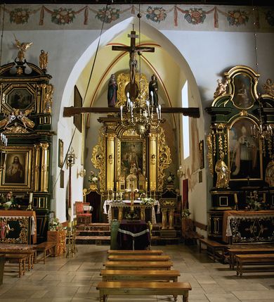 Zdjęcie nr 30: Kościół jest usytuowany w centrum wsi Rudawa, na północ od głównej drogi z Zabierzowa do Chrzanowa. Teren wokół niego jest otoczony wysokim, kamiennym murem z nieregularnych ciosów kamienia, oszkarpowanym, tynkowanym, z wyjątkiem zewnętrznej części muru na zachód od południowej bramki. W murze znajdują się trzy wejścia, od wschodu, południa i zachodu. W części wschodniej muru znajduje się trójosiowa brama wjazdowa, zwieńczona łukiem wklęsło-wypukłym, z trzema przelotami: środkowym wyższym i szerszym, zamkniętym łukiem odcinkowym i bocznymi węższymi i niższymi, zamkniętymi łukiem półkolistym (północne zamurowane). Część środkowa jest flankowana zdwojonymi pilastrami, podtrzymującymi profilowane uskokowe belkowanie z przyczółkiem o profilowanym łuku falistym, zwieńczonym równoramiennym krzyżem. W przyczółku wnęka z figurą św. Floriana. Bramki od strony zachodniej i południowej prostokątne, z przejściem zakończonym płaskim łukiem odcinkowym, z profilowanym gzymsem, zwieńczonym trójkątnym przyczółkiem. Przejścia zamykane drewnianymi ażurowymi i pomalowanymi na ciemnobrązowo jednoskrzydłowymi drzwiami. Poprzez bramkę od zachodu zejście kamiennymi schodami poprowadzonymi wzdłuż muru na dziedziniec plebański, usytuowany poniżej terenu kościelnego. 
W północno-wschodnim narożniku muru niewielka murowana i tynkowana kostnica na planie kwadratu, nakryta dachem namiotowym, łamanym, zakończonym ośmioboczną ślepą latarnią.

Po stronie południowej, poniżej placu kościelnego, do muru przylega murowana, tynkowana, prostokątna i dwukondygnacyjna „zegarowa” wieża bramna nakryta namiotowym dachem z wysoką drewnianą ośmioboczną latarnią o cebulastym hełmie. W wieży znajduje się przejazd wiodący na dziedziniec plebański, z sienią otwartą na przestrzał w dolnej kondygnacji i z lamusem dostępnym od strony placu kościelnego w górnej. 

W południowej części muru, w pobliżu południowo-wschodniego narożnika placu kościelnego, nadbudowana kamienna dzwonnica parawanowa z zawieszonymi czterema dzwonami.  

We wschodniej części placu kościelnego pomiędzy bramką wschodnią a kostnicą znajduje się kamienna ambona, o ośmiobocznej podstawie przechodzącej w szerszy, również ośmioboczny korpus, zakończony kamiennym parapetem, z kamiennymi schodami prowadzącymi na ambonę od strony wschodniej. 

Kościół jest orientowany, prawie w całości zbudowany z cegły, otynkowany z wyjątkiem prezbiterium. Wnętrze kościoła tworzy niewielkie, prostokątne, jednoprzęsłowe prezbiterium zakończone prostą ścianą i nakryte pozornym sklepieniem krzyżowo-żebrowym. Nawa jest szersza, prawie kwadratowa, nakryta drewnianym stropem. Prezbiterium z nawą są połączone szeroką, ostrołukową arkadą w ścianie tęczowej. Od północy do prezbiterium przylega założona na planie prostokąta dwuprzęsłowa zakrystia, nakryta sklepieniem krzyżowym. Wejście do zakrystii zaznaczone gotyckim, kamiennym, sfazowanym portalem zamkniętym łukiem ostrym. Od zachodu do zakrystii przylega niewielkie pomieszczenie gospodarcze, do którego z zakrystii prowadzą ostrołukowe drzwi. Zakrystia oświetlona ostrołukowym oknem w ścianie wschodniej, wypełnionym witrażem z tafelek w kształcie sześciokąta foremnego, ze szkła surowego, tzw. katedralnego. 

Od południa do nawy przylega kaplica o formach renesansowych, dwukondygnacyjna, założona na planie kwadratu. W dolnej kondygnacji sklepiona krzyżowo-żebrowo kruchta otwarta do nawy szeroką, zamkniętą półkoliście arkadą.

Ponad kruchtą kaplica św. Kazimierza, nakryta wspartą na pendentywach kopułą z latarnią. Z kruchty do kaplicy prowadzą kręte kamienne schody umieszczone od zachodu w półkolistej wieżyczce. Prostokątne wejście z krypty na klatkę schodową ujęte kamiennym profilowanym portalem. Kaplica otwarta do nawy szeroką, zamkniętą półkoliście arkadą, o kształcie i wymiarach analogicznych do arkady znajdującej się poniżej. Kaplicę, prócz latarni, oświetla prostokątne okno w ścianie południowej, wypełnione witrażem z tafelek w kształcie gomółek, ze szkła surowego, tzw. katedralnego. Na zachodniej ścianie nawy chór muzyczny, dostępny klatką schodową ukrytą w zewnętrznym aneksie przylegającym do zachodniej elewacji nawy i południowej elewacji wieży-dzwonnicy. 

Nawę i prezbiterium oświetlają umieszczone w południowych ścianach prostokątne, rozglifione okna: jedno w prezbiterium, dwa w nawie. Wszystkie wypełnione witrażami z tafelek w kształcie gomółek, ze szkła surowego, tzw. katedralnego. 

Do kościoła prowadzą dwa wejścia: poprzez arkadę z kruchty południowej oraz szerokie wejście główne prostokątne, zamknięte łukiem odcinkowym, prowadzące do kościoła z obszernej kruchty od strony zachodniej, znajdującej się w murowanym przyziemiu wieży - dzwonnicy. Kruchta, założona na planie kwadratu i nakryta murowanym stropem, doświetlona jest dwoma prostokątnymi oknami umieszczonymi naprzeciw siebie w ścianach północnej i południowej.
 
W zewnętrznej elewacji kościoła widoczny niewysoki kamienny cokół wykonany z nieregularnych ciosów kamienia. Prezbiterium, niższe od nawy, murowane z cegły w układzie wedyjskim, z domieszką układu polskiego. Wschodnie naroża prezbiterium zaakcentowane płaskimi lizenami. We wschodniej ścianie widoczny zarys zamurowanego wydłużonego okna zamkniętego lekko zaostrzonym łukiem, w trójkątnym szczycie znajduje się niewielkie wąskie okienko zakończone łukiem półkolistym. Południowa ściana prezbiterium ozdobiona fryzem z cegieł. Do ściany północnej prezbiterium przylega zakrystia, oszkarpowana, nakryta dachem pulpitowym, z dobudowanym od niej niewielkim aneksem, nakrytym takim samym zadaszeniem. Do wschodniej ściany prezbiterium przylega ogrójec nakryty dachem namiotowym z cebulastym zwieńczeniem, wspartym na sześciu smukłych, profilowanych drewnianych słupach z mieczami, pomiędzy którymi od północy i południa ażurowa drewniana balustrada. 

Nawa oszkarpowana w narożnikach. Elewacje bez podziałów architektonicznych. Od strony południowej do nawy dobudowana dwukondygnacyjna kaplica nakryta kopułą z latarnią, podzielona na dwie kondygnacje. W dolnej kondygnacji od południa wejście do kruchty zaznaczone kamiennym portalem o sfazowanych węgarach i lekko zaostrzonym łuku. Wejście zamykają drewniane dwuskrzydłowe drzwi ozdobione kratownicą z żelaznych listew. Od zachodu do kaplicy przylega półokrągła wieżyczka nakryta daszkiem stożkowym. 

Do zachodniej fasady kościoła dostawiona niska, założona na planie kwadratu trójkondygnacyjna wieża-dzwonnica: w dolnej części murowana, w narożach wzmocniona kamiennymi szkarpami, w górnej drewniana konstrukcji słupowo-ramowej z nadwieszoną izbicą i nakryta dachem półszczytowym. W dolnej, murowanej kondygnacji, na osi kościoła, prostokątne wejście do kruchty zaakcentowane przedsionkiem w kształcie ostrołukowej arkady i czterostopniowymi schodami. Przedsionek nakryty dachem dwuspadowym. Do zachodniej elewacji nawy i południowej elewacji dzwonnicy przylega niewielki, wysoki drewniany aneks, nakryty dachem pulpitowym, mieszczący klatkę schodową prowadzącą na górną kondygnację dzwonnicy i na chór muzyczny w nawie kościoła. Prostokątne wejście w południowej ścianie aneksu, do którego prowadzą pięciostopniowe proste schody. Ponad nimi, na wysokości drugiej kondygnacji dzwonnicy, niewielkie kwadratowe okno. 

Prezbiterium i nawa przykryte stromymi dachami dwuspadowymi, zamkniętymi od wschodu i zachodu szczytami sterczynowymi. Wieżyczka na sygnaturkę ośmioboczna, w dolnej części barokowa, w górnej części nowsza.