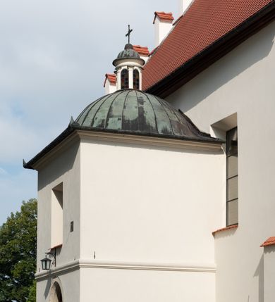 Zdjęcie nr 71: Kościół jest usytuowany w centrum wsi Rudawa, na północ od głównej drogi z Zabierzowa do Chrzanowa. Teren wokół niego jest otoczony wysokim, kamiennym murem z nieregularnych ciosów kamienia, oszkarpowanym, tynkowanym, z wyjątkiem zewnętrznej części muru na zachód od południowej bramki. W murze znajdują się trzy wejścia, od wschodu, południa i zachodu. W części wschodniej muru znajduje się trójosiowa brama wjazdowa, zwieńczona łukiem wklęsło-wypukłym, z trzema przelotami: środkowym wyższym i szerszym, zamkniętym łukiem odcinkowym i bocznymi węższymi i niższymi, zamkniętymi łukiem półkolistym (północne zamurowane). Część środkowa jest flankowana zdwojonymi pilastrami, podtrzymującymi profilowane uskokowe belkowanie z przyczółkiem o profilowanym łuku falistym, zwieńczonym równoramiennym krzyżem. W przyczółku wnęka z figurą św. Floriana. Bramki od strony zachodniej i południowej prostokątne, z przejściem zakończonym płaskim łukiem odcinkowym, z profilowanym gzymsem, zwieńczonym trójkątnym przyczółkiem. Przejścia zamykane drewnianymi ażurowymi i pomalowanymi na ciemnobrązowo jednoskrzydłowymi drzwiami. Poprzez bramkę od zachodu zejście kamiennymi schodami poprowadzonymi wzdłuż muru na dziedziniec plebański, usytuowany poniżej terenu kościelnego. 
W północno-wschodnim narożniku muru niewielka murowana i tynkowana kostnica na planie kwadratu, nakryta dachem namiotowym, łamanym, zakończonym ośmioboczną ślepą latarnią.

Po stronie południowej, poniżej placu kościelnego, do muru przylega murowana, tynkowana, prostokątna i dwukondygnacyjna „zegarowa” wieża bramna nakryta namiotowym dachem z wysoką drewnianą ośmioboczną latarnią o cebulastym hełmie. W wieży znajduje się przejazd wiodący na dziedziniec plebański, z sienią otwartą na przestrzał w dolnej kondygnacji i z lamusem dostępnym od strony placu kościelnego w górnej. 

W południowej części muru, w pobliżu południowo-wschodniego narożnika placu kościelnego, nadbudowana kamienna dzwonnica parawanowa z zawieszonymi czterema dzwonami.  

We wschodniej części placu kościelnego pomiędzy bramką wschodnią a kostnicą znajduje się kamienna ambona, o ośmiobocznej podstawie przechodzącej w szerszy, również ośmioboczny korpus, zakończony kamiennym parapetem, z kamiennymi schodami prowadzącymi na ambonę od strony wschodniej. 

Kościół jest orientowany, prawie w całości zbudowany z cegły, otynkowany z wyjątkiem prezbiterium. Wnętrze kościoła tworzy niewielkie, prostokątne, jednoprzęsłowe prezbiterium zakończone prostą ścianą i nakryte pozornym sklepieniem krzyżowo-żebrowym. Nawa jest szersza, prawie kwadratowa, nakryta drewnianym stropem. Prezbiterium z nawą są połączone szeroką, ostrołukową arkadą w ścianie tęczowej. Od północy do prezbiterium przylega założona na planie prostokąta dwuprzęsłowa zakrystia, nakryta sklepieniem krzyżowym. Wejście do zakrystii zaznaczone gotyckim, kamiennym, sfazowanym portalem zamkniętym łukiem ostrym. Od zachodu do zakrystii przylega niewielkie pomieszczenie gospodarcze, do którego z zakrystii prowadzą ostrołukowe drzwi. Zakrystia oświetlona ostrołukowym oknem w ścianie wschodniej, wypełnionym witrażem z tafelek w kształcie sześciokąta foremnego, ze szkła surowego, tzw. katedralnego. 

Od południa do nawy przylega kaplica o formach renesansowych, dwukondygnacyjna, założona na planie kwadratu. W dolnej kondygnacji sklepiona krzyżowo-żebrowo kruchta otwarta do nawy szeroką, zamkniętą półkoliście arkadą.

Ponad kruchtą kaplica św. Kazimierza, nakryta wspartą na pendentywach kopułą z latarnią. Z kruchty do kaplicy prowadzą kręte kamienne schody umieszczone od zachodu w półkolistej wieżyczce. Prostokątne wejście z krypty na klatkę schodową ujęte kamiennym profilowanym portalem. Kaplica otwarta do nawy szeroką, zamkniętą półkoliście arkadą, o kształcie i wymiarach analogicznych do arkady znajdującej się poniżej. Kaplicę, prócz latarni, oświetla prostokątne okno w ścianie południowej, wypełnione witrażem z tafelek w kształcie gomółek, ze szkła surowego, tzw. katedralnego. Na zachodniej ścianie nawy chór muzyczny, dostępny klatką schodową ukrytą w zewnętrznym aneksie przylegającym do zachodniej elewacji nawy i południowej elewacji wieży-dzwonnicy. 

Nawę i prezbiterium oświetlają umieszczone w południowych ścianach prostokątne, rozglifione okna: jedno w prezbiterium, dwa w nawie. Wszystkie wypełnione witrażami z tafelek w kształcie gomółek, ze szkła surowego, tzw. katedralnego. 

Do kościoła prowadzą dwa wejścia: poprzez arkadę z kruchty południowej oraz szerokie wejście główne prostokątne, zamknięte łukiem odcinkowym, prowadzące do kościoła z obszernej kruchty od strony zachodniej, znajdującej się w murowanym przyziemiu wieży - dzwonnicy. Kruchta, założona na planie kwadratu i nakryta murowanym stropem, doświetlona jest dwoma prostokątnymi oknami umieszczonymi naprzeciw siebie w ścianach północnej i południowej.
 
W zewnętrznej elewacji kościoła widoczny niewysoki kamienny cokół wykonany z nieregularnych ciosów kamienia. Prezbiterium, niższe od nawy, murowane z cegły w układzie wedyjskim, z domieszką układu polskiego. Wschodnie naroża prezbiterium zaakcentowane płaskimi lizenami. We wschodniej ścianie widoczny zarys zamurowanego wydłużonego okna zamkniętego lekko zaostrzonym łukiem, w trójkątnym szczycie znajduje się niewielkie wąskie okienko zakończone łukiem półkolistym. Południowa ściana prezbiterium ozdobiona fryzem z cegieł. Do ściany północnej prezbiterium przylega zakrystia, oszkarpowana, nakryta dachem pulpitowym, z dobudowanym od niej niewielkim aneksem, nakrytym takim samym zadaszeniem. Do wschodniej ściany prezbiterium przylega ogrójec nakryty dachem namiotowym z cebulastym zwieńczeniem, wspartym na sześciu smukłych, profilowanych drewnianych słupach z mieczami, pomiędzy którymi od północy i południa ażurowa drewniana balustrada. 

Nawa oszkarpowana w narożnikach. Elewacje bez podziałów architektonicznych. Od strony południowej do nawy dobudowana dwukondygnacyjna kaplica nakryta kopułą z latarnią, podzielona na dwie kondygnacje. W dolnej kondygnacji od południa wejście do kruchty zaznaczone kamiennym portalem o sfazowanych węgarach i lekko zaostrzonym łuku. Wejście zamykają drewniane dwuskrzydłowe drzwi ozdobione kratownicą z żelaznych listew. Od zachodu do kaplicy przylega półokrągła wieżyczka nakryta daszkiem stożkowym. 

Do zachodniej fasady kościoła dostawiona niska, założona na planie kwadratu trójkondygnacyjna wieża-dzwonnica: w dolnej części murowana, w narożach wzmocniona kamiennymi szkarpami, w górnej drewniana konstrukcji słupowo-ramowej z nadwieszoną izbicą i nakryta dachem półszczytowym. W dolnej, murowanej kondygnacji, na osi kościoła, prostokątne wejście do kruchty zaakcentowane przedsionkiem w kształcie ostrołukowej arkady i czterostopniowymi schodami. Przedsionek nakryty dachem dwuspadowym. Do zachodniej elewacji nawy i południowej elewacji dzwonnicy przylega niewielki, wysoki drewniany aneks, nakryty dachem pulpitowym, mieszczący klatkę schodową prowadzącą na górną kondygnację dzwonnicy i na chór muzyczny w nawie kościoła. Prostokątne wejście w południowej ścianie aneksu, do którego prowadzą pięciostopniowe proste schody. Ponad nimi, na wysokości drugiej kondygnacji dzwonnicy, niewielkie kwadratowe okno. 

Prezbiterium i nawa przykryte stromymi dachami dwuspadowymi, zamkniętymi od wschodu i zachodu szczytami sterczynowymi. Wieżyczka na sygnaturkę ośmioboczna, w dolnej części barokowa, w górnej części nowsza.