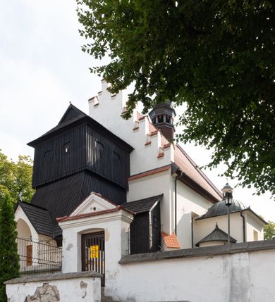 Zdjęcie nr 15: Kościół jest usytuowany w centrum wsi Rudawa, na północ od głównej drogi z Zabierzowa do Chrzanowa. Teren wokół niego jest otoczony wysokim, kamiennym murem z nieregularnych ciosów kamienia, oszkarpowanym, tynkowanym, z wyjątkiem zewnętrznej części muru na zachód od południowej bramki. W murze znajdują się trzy wejścia, od wschodu, południa i zachodu. W części wschodniej muru znajduje się trójosiowa brama wjazdowa, zwieńczona łukiem wklęsło-wypukłym, z trzema przelotami: środkowym wyższym i szerszym, zamkniętym łukiem odcinkowym i bocznymi węższymi i niższymi, zamkniętymi łukiem półkolistym (północne zamurowane). Część środkowa jest flankowana zdwojonymi pilastrami, podtrzymującymi profilowane uskokowe belkowanie z przyczółkiem o profilowanym łuku falistym, zwieńczonym równoramiennym krzyżem. W przyczółku wnęka z figurą św. Floriana. Bramki od strony zachodniej i południowej prostokątne, z przejściem zakończonym płaskim łukiem odcinkowym, z profilowanym gzymsem, zwieńczonym trójkątnym przyczółkiem. Przejścia zamykane drewnianymi ażurowymi i pomalowanymi na ciemnobrązowo jednoskrzydłowymi drzwiami. Poprzez bramkę od zachodu zejście kamiennymi schodami poprowadzonymi wzdłuż muru na dziedziniec plebański, usytuowany poniżej terenu kościelnego. 
W północno-wschodnim narożniku muru niewielka murowana i tynkowana kostnica na planie kwadratu, nakryta dachem namiotowym, łamanym, zakończonym ośmioboczną ślepą latarnią.

Po stronie południowej, poniżej placu kościelnego, do muru przylega murowana, tynkowana, prostokątna i dwukondygnacyjna „zegarowa” wieża bramna nakryta namiotowym dachem z wysoką drewnianą ośmioboczną latarnią o cebulastym hełmie. W wieży znajduje się przejazd wiodący na dziedziniec plebański, z sienią otwartą na przestrzał w dolnej kondygnacji i z lamusem dostępnym od strony placu kościelnego w górnej. 

W południowej części muru, w pobliżu południowo-wschodniego narożnika placu kościelnego, nadbudowana kamienna dzwonnica parawanowa z zawieszonymi czterema dzwonami.  

We wschodniej części placu kościelnego pomiędzy bramką wschodnią a kostnicą znajduje się kamienna ambona, o ośmiobocznej podstawie przechodzącej w szerszy, również ośmioboczny korpus, zakończony kamiennym parapetem, z kamiennymi schodami prowadzącymi na ambonę od strony wschodniej. 

Kościół jest orientowany, prawie w całości zbudowany z cegły, otynkowany z wyjątkiem prezbiterium. Wnętrze kościoła tworzy niewielkie, prostokątne, jednoprzęsłowe prezbiterium zakończone prostą ścianą i nakryte pozornym sklepieniem krzyżowo-żebrowym. Nawa jest szersza, prawie kwadratowa, nakryta drewnianym stropem. Prezbiterium z nawą są połączone szeroką, ostrołukową arkadą w ścianie tęczowej. Od północy do prezbiterium przylega założona na planie prostokąta dwuprzęsłowa zakrystia, nakryta sklepieniem krzyżowym. Wejście do zakrystii zaznaczone gotyckim, kamiennym, sfazowanym portalem zamkniętym łukiem ostrym. Od zachodu do zakrystii przylega niewielkie pomieszczenie gospodarcze, do którego z zakrystii prowadzą ostrołukowe drzwi. Zakrystia oświetlona ostrołukowym oknem w ścianie wschodniej, wypełnionym witrażem z tafelek w kształcie sześciokąta foremnego, ze szkła surowego, tzw. katedralnego. 

Od południa do nawy przylega kaplica o formach renesansowych, dwukondygnacyjna, założona na planie kwadratu. W dolnej kondygnacji sklepiona krzyżowo-żebrowo kruchta otwarta do nawy szeroką, zamkniętą półkoliście arkadą.

Ponad kruchtą kaplica św. Kazimierza, nakryta wspartą na pendentywach kopułą z latarnią. Z kruchty do kaplicy prowadzą kręte kamienne schody umieszczone od zachodu w półkolistej wieżyczce. Prostokątne wejście z krypty na klatkę schodową ujęte kamiennym profilowanym portalem. Kaplica otwarta do nawy szeroką, zamkniętą półkoliście arkadą, o kształcie i wymiarach analogicznych do arkady znajdującej się poniżej. Kaplicę, prócz latarni, oświetla prostokątne okno w ścianie południowej, wypełnione witrażem z tafelek w kształcie gomółek, ze szkła surowego, tzw. katedralnego. Na zachodniej ścianie nawy chór muzyczny, dostępny klatką schodową ukrytą w zewnętrznym aneksie przylegającym do zachodniej elewacji nawy i południowej elewacji wieży-dzwonnicy. 

Nawę i prezbiterium oświetlają umieszczone w południowych ścianach prostokątne, rozglifione okna: jedno w prezbiterium, dwa w nawie. Wszystkie wypełnione witrażami z tafelek w kształcie gomółek, ze szkła surowego, tzw. katedralnego. 

Do kościoła prowadzą dwa wejścia: poprzez arkadę z kruchty południowej oraz szerokie wejście główne prostokątne, zamknięte łukiem odcinkowym, prowadzące do kościoła z obszernej kruchty od strony zachodniej, znajdującej się w murowanym przyziemiu wieży - dzwonnicy. Kruchta, założona na planie kwadratu i nakryta murowanym stropem, doświetlona jest dwoma prostokątnymi oknami umieszczonymi naprzeciw siebie w ścianach północnej i południowej.
 
W zewnętrznej elewacji kościoła widoczny niewysoki kamienny cokół wykonany z nieregularnych ciosów kamienia. Prezbiterium, niższe od nawy, murowane z cegły w układzie wedyjskim, z domieszką układu polskiego. Wschodnie naroża prezbiterium zaakcentowane płaskimi lizenami. We wschodniej ścianie widoczny zarys zamurowanego wydłużonego okna zamkniętego lekko zaostrzonym łukiem, w trójkątnym szczycie znajduje się niewielkie wąskie okienko zakończone łukiem półkolistym. Południowa ściana prezbiterium ozdobiona fryzem z cegieł. Do ściany północnej prezbiterium przylega zakrystia, oszkarpowana, nakryta dachem pulpitowym, z dobudowanym od niej niewielkim aneksem, nakrytym takim samym zadaszeniem. Do wschodniej ściany prezbiterium przylega ogrójec nakryty dachem namiotowym z cebulastym zwieńczeniem, wspartym na sześciu smukłych, profilowanych drewnianych słupach z mieczami, pomiędzy którymi od północy i południa ażurowa drewniana balustrada. 

Nawa oszkarpowana w narożnikach. Elewacje bez podziałów architektonicznych. Od strony południowej do nawy dobudowana dwukondygnacyjna kaplica nakryta kopułą z latarnią, podzielona na dwie kondygnacje. W dolnej kondygnacji od południa wejście do kruchty zaznaczone kamiennym portalem o sfazowanych węgarach i lekko zaostrzonym łuku. Wejście zamykają drewniane dwuskrzydłowe drzwi ozdobione kratownicą z żelaznych listew. Od zachodu do kaplicy przylega półokrągła wieżyczka nakryta daszkiem stożkowym. 

Do zachodniej fasady kościoła dostawiona niska, założona na planie kwadratu trójkondygnacyjna wieża-dzwonnica: w dolnej części murowana, w narożach wzmocniona kamiennymi szkarpami, w górnej drewniana konstrukcji słupowo-ramowej z nadwieszoną izbicą i nakryta dachem półszczytowym. W dolnej, murowanej kondygnacji, na osi kościoła, prostokątne wejście do kruchty zaakcentowane przedsionkiem w kształcie ostrołukowej arkady i czterostopniowymi schodami. Przedsionek nakryty dachem dwuspadowym. Do zachodniej elewacji nawy i południowej elewacji dzwonnicy przylega niewielki, wysoki drewniany aneks, nakryty dachem pulpitowym, mieszczący klatkę schodową prowadzącą na górną kondygnację dzwonnicy i na chór muzyczny w nawie kościoła. Prostokątne wejście w południowej ścianie aneksu, do którego prowadzą pięciostopniowe proste schody. Ponad nimi, na wysokości drugiej kondygnacji dzwonnicy, niewielkie kwadratowe okno. 

Prezbiterium i nawa przykryte stromymi dachami dwuspadowymi, zamkniętymi od wschodu i zachodu szczytami sterczynowymi. Wieżyczka na sygnaturkę ośmioboczna, w dolnej części barokowa, w górnej części nowsza.