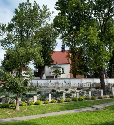 Zdjęcie nr 26: Kościół jest usytuowany w centrum wsi Rudawa, na północ od głównej drogi z Zabierzowa do Chrzanowa. Teren wokół niego jest otoczony wysokim, kamiennym murem z nieregularnych ciosów kamienia, oszkarpowanym, tynkowanym, z wyjątkiem zewnętrznej części muru na zachód od południowej bramki. W murze znajdują się trzy wejścia, od wschodu, południa i zachodu. W części wschodniej muru znajduje się trójosiowa brama wjazdowa, zwieńczona łukiem wklęsło-wypukłym, z trzema przelotami: środkowym wyższym i szerszym, zamkniętym łukiem odcinkowym i bocznymi węższymi i niższymi, zamkniętymi łukiem półkolistym (północne zamurowane). Część środkowa jest flankowana zdwojonymi pilastrami, podtrzymującymi profilowane uskokowe belkowanie z przyczółkiem o profilowanym łuku falistym, zwieńczonym równoramiennym krzyżem. W przyczółku wnęka z figurą św. Floriana. Bramki od strony zachodniej i południowej prostokątne, z przejściem zakończonym płaskim łukiem odcinkowym, z profilowanym gzymsem, zwieńczonym trójkątnym przyczółkiem. Przejścia zamykane drewnianymi ażurowymi i pomalowanymi na ciemnobrązowo jednoskrzydłowymi drzwiami. Poprzez bramkę od zachodu zejście kamiennymi schodami poprowadzonymi wzdłuż muru na dziedziniec plebański, usytuowany poniżej terenu kościelnego. 
W północno-wschodnim narożniku muru niewielka murowana i tynkowana kostnica na planie kwadratu, nakryta dachem namiotowym, łamanym, zakończonym ośmioboczną ślepą latarnią.

Po stronie południowej, poniżej placu kościelnego, do muru przylega murowana, tynkowana, prostokątna i dwukondygnacyjna „zegarowa” wieża bramna nakryta namiotowym dachem z wysoką drewnianą ośmioboczną latarnią o cebulastym hełmie. W wieży znajduje się przejazd wiodący na dziedziniec plebański, z sienią otwartą na przestrzał w dolnej kondygnacji i z lamusem dostępnym od strony placu kościelnego w górnej. 

W południowej części muru, w pobliżu południowo-wschodniego narożnika placu kościelnego, nadbudowana kamienna dzwonnica parawanowa z zawieszonymi czterema dzwonami.  

We wschodniej części placu kościelnego pomiędzy bramką wschodnią a kostnicą znajduje się kamienna ambona, o ośmiobocznej podstawie przechodzącej w szerszy, również ośmioboczny korpus, zakończony kamiennym parapetem, z kamiennymi schodami prowadzącymi na ambonę od strony wschodniej. 

Kościół jest orientowany, prawie w całości zbudowany z cegły, otynkowany z wyjątkiem prezbiterium. Wnętrze kościoła tworzy niewielkie, prostokątne, jednoprzęsłowe prezbiterium zakończone prostą ścianą i nakryte pozornym sklepieniem krzyżowo-żebrowym. Nawa jest szersza, prawie kwadratowa, nakryta drewnianym stropem. Prezbiterium z nawą są połączone szeroką, ostrołukową arkadą w ścianie tęczowej. Od północy do prezbiterium przylega założona na planie prostokąta dwuprzęsłowa zakrystia, nakryta sklepieniem krzyżowym. Wejście do zakrystii zaznaczone gotyckim, kamiennym, sfazowanym portalem zamkniętym łukiem ostrym. Od zachodu do zakrystii przylega niewielkie pomieszczenie gospodarcze, do którego z zakrystii prowadzą ostrołukowe drzwi. Zakrystia oświetlona ostrołukowym oknem w ścianie wschodniej, wypełnionym witrażem z tafelek w kształcie sześciokąta foremnego, ze szkła surowego, tzw. katedralnego. 

Od południa do nawy przylega kaplica o formach renesansowych, dwukondygnacyjna, założona na planie kwadratu. W dolnej kondygnacji sklepiona krzyżowo-żebrowo kruchta otwarta do nawy szeroką, zamkniętą półkoliście arkadą.

Ponad kruchtą kaplica św. Kazimierza, nakryta wspartą na pendentywach kopułą z latarnią. Z kruchty do kaplicy prowadzą kręte kamienne schody umieszczone od zachodu w półkolistej wieżyczce. Prostokątne wejście z krypty na klatkę schodową ujęte kamiennym profilowanym portalem. Kaplica otwarta do nawy szeroką, zamkniętą półkoliście arkadą, o kształcie i wymiarach analogicznych do arkady znajdującej się poniżej. Kaplicę, prócz latarni, oświetla prostokątne okno w ścianie południowej, wypełnione witrażem z tafelek w kształcie gomółek, ze szkła surowego, tzw. katedralnego. Na zachodniej ścianie nawy chór muzyczny, dostępny klatką schodową ukrytą w zewnętrznym aneksie przylegającym do zachodniej elewacji nawy i południowej elewacji wieży-dzwonnicy. 

Nawę i prezbiterium oświetlają umieszczone w południowych ścianach prostokątne, rozglifione okna: jedno w prezbiterium, dwa w nawie. Wszystkie wypełnione witrażami z tafelek w kształcie gomółek, ze szkła surowego, tzw. katedralnego. 

Do kościoła prowadzą dwa wejścia: poprzez arkadę z kruchty południowej oraz szerokie wejście główne prostokątne, zamknięte łukiem odcinkowym, prowadzące do kościoła z obszernej kruchty od strony zachodniej, znajdującej się w murowanym przyziemiu wieży - dzwonnicy. Kruchta, założona na planie kwadratu i nakryta murowanym stropem, doświetlona jest dwoma prostokątnymi oknami umieszczonymi naprzeciw siebie w ścianach północnej i południowej.
 
W zewnętrznej elewacji kościoła widoczny niewysoki kamienny cokół wykonany z nieregularnych ciosów kamienia. Prezbiterium, niższe od nawy, murowane z cegły w układzie wedyjskim, z domieszką układu polskiego. Wschodnie naroża prezbiterium zaakcentowane płaskimi lizenami. We wschodniej ścianie widoczny zarys zamurowanego wydłużonego okna zamkniętego lekko zaostrzonym łukiem, w trójkątnym szczycie znajduje się niewielkie wąskie okienko zakończone łukiem półkolistym. Południowa ściana prezbiterium ozdobiona fryzem z cegieł. Do ściany północnej prezbiterium przylega zakrystia, oszkarpowana, nakryta dachem pulpitowym, z dobudowanym od niej niewielkim aneksem, nakrytym takim samym zadaszeniem. Do wschodniej ściany prezbiterium przylega ogrójec nakryty dachem namiotowym z cebulastym zwieńczeniem, wspartym na sześciu smukłych, profilowanych drewnianych słupach z mieczami, pomiędzy którymi od północy i południa ażurowa drewniana balustrada. 

Nawa oszkarpowana w narożnikach. Elewacje bez podziałów architektonicznych. Od strony południowej do nawy dobudowana dwukondygnacyjna kaplica nakryta kopułą z latarnią, podzielona na dwie kondygnacje. W dolnej kondygnacji od południa wejście do kruchty zaznaczone kamiennym portalem o sfazowanych węgarach i lekko zaostrzonym łuku. Wejście zamykają drewniane dwuskrzydłowe drzwi ozdobione kratownicą z żelaznych listew. Od zachodu do kaplicy przylega półokrągła wieżyczka nakryta daszkiem stożkowym. 

Do zachodniej fasady kościoła dostawiona niska, założona na planie kwadratu trójkondygnacyjna wieża-dzwonnica: w dolnej części murowana, w narożach wzmocniona kamiennymi szkarpami, w górnej drewniana konstrukcji słupowo-ramowej z nadwieszoną izbicą i nakryta dachem półszczytowym. W dolnej, murowanej kondygnacji, na osi kościoła, prostokątne wejście do kruchty zaakcentowane przedsionkiem w kształcie ostrołukowej arkady i czterostopniowymi schodami. Przedsionek nakryty dachem dwuspadowym. Do zachodniej elewacji nawy i południowej elewacji dzwonnicy przylega niewielki, wysoki drewniany aneks, nakryty dachem pulpitowym, mieszczący klatkę schodową prowadzącą na górną kondygnację dzwonnicy i na chór muzyczny w nawie kościoła. Prostokątne wejście w południowej ścianie aneksu, do którego prowadzą pięciostopniowe proste schody. Ponad nimi, na wysokości drugiej kondygnacji dzwonnicy, niewielkie kwadratowe okno. 

Prezbiterium i nawa przykryte stromymi dachami dwuspadowymi, zamkniętymi od wschodu i zachodu szczytami sterczynowymi. Wieżyczka na sygnaturkę ośmioboczna, w dolnej części barokowa, w górnej części nowsza.