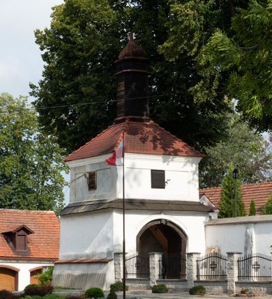Zdjęcie nr 36: Kościół jest usytuowany w centrum wsi Rudawa, na północ od głównej drogi z Zabierzowa do Chrzanowa. Teren wokół niego jest otoczony wysokim, kamiennym murem z nieregularnych ciosów kamienia, oszkarpowanym, tynkowanym, z wyjątkiem zewnętrznej części muru na zachód od południowej bramki. W murze znajdują się trzy wejścia, od wschodu, południa i zachodu. W części wschodniej muru znajduje się trójosiowa brama wjazdowa, zwieńczona łukiem wklęsło-wypukłym, z trzema przelotami: środkowym wyższym i szerszym, zamkniętym łukiem odcinkowym i bocznymi węższymi i niższymi, zamkniętymi łukiem półkolistym (północne zamurowane). Część środkowa jest flankowana zdwojonymi pilastrami, podtrzymującymi profilowane uskokowe belkowanie z przyczółkiem o profilowanym łuku falistym, zwieńczonym równoramiennym krzyżem. W przyczółku wnęka z figurą św. Floriana. Bramki od strony zachodniej i południowej prostokątne, z przejściem zakończonym płaskim łukiem odcinkowym, z profilowanym gzymsem, zwieńczonym trójkątnym przyczółkiem. Przejścia zamykane drewnianymi ażurowymi i pomalowanymi na ciemnobrązowo jednoskrzydłowymi drzwiami. Poprzez bramkę od zachodu zejście kamiennymi schodami poprowadzonymi wzdłuż muru na dziedziniec plebański, usytuowany poniżej terenu kościelnego. 
W północno-wschodnim narożniku muru niewielka murowana i tynkowana kostnica na planie kwadratu, nakryta dachem namiotowym, łamanym, zakończonym ośmioboczną ślepą latarnią.

Po stronie południowej, poniżej placu kościelnego, do muru przylega murowana, tynkowana, prostokątna i dwukondygnacyjna „zegarowa” wieża bramna nakryta namiotowym dachem z wysoką drewnianą ośmioboczną latarnią o cebulastym hełmie. W wieży znajduje się przejazd wiodący na dziedziniec plebański, z sienią otwartą na przestrzał w dolnej kondygnacji i z lamusem dostępnym od strony placu kościelnego w górnej. 

W południowej części muru, w pobliżu południowo-wschodniego narożnika placu kościelnego, nadbudowana kamienna dzwonnica parawanowa z zawieszonymi czterema dzwonami.  

We wschodniej części placu kościelnego pomiędzy bramką wschodnią a kostnicą znajduje się kamienna ambona, o ośmiobocznej podstawie przechodzącej w szerszy, również ośmioboczny korpus, zakończony kamiennym parapetem, z kamiennymi schodami prowadzącymi na ambonę od strony wschodniej. 

Kościół jest orientowany, prawie w całości zbudowany z cegły, otynkowany z wyjątkiem prezbiterium. Wnętrze kościoła tworzy niewielkie, prostokątne, jednoprzęsłowe prezbiterium zakończone prostą ścianą i nakryte pozornym sklepieniem krzyżowo-żebrowym. Nawa jest szersza, prawie kwadratowa, nakryta drewnianym stropem. Prezbiterium z nawą są połączone szeroką, ostrołukową arkadą w ścianie tęczowej. Od północy do prezbiterium przylega założona na planie prostokąta dwuprzęsłowa zakrystia, nakryta sklepieniem krzyżowym. Wejście do zakrystii zaznaczone gotyckim, kamiennym, sfazowanym portalem zamkniętym łukiem ostrym. Od zachodu do zakrystii przylega niewielkie pomieszczenie gospodarcze, do którego z zakrystii prowadzą ostrołukowe drzwi. Zakrystia oświetlona ostrołukowym oknem w ścianie wschodniej, wypełnionym witrażem z tafelek w kształcie sześciokąta foremnego, ze szkła surowego, tzw. katedralnego. 

Od południa do nawy przylega kaplica o formach renesansowych, dwukondygnacyjna, założona na planie kwadratu. W dolnej kondygnacji sklepiona krzyżowo-żebrowo kruchta otwarta do nawy szeroką, zamkniętą półkoliście arkadą.

Ponad kruchtą kaplica św. Kazimierza, nakryta wspartą na pendentywach kopułą z latarnią. Z kruchty do kaplicy prowadzą kręte kamienne schody umieszczone od zachodu w półkolistej wieżyczce. Prostokątne wejście z krypty na klatkę schodową ujęte kamiennym profilowanym portalem. Kaplica otwarta do nawy szeroką, zamkniętą półkoliście arkadą, o kształcie i wymiarach analogicznych do arkady znajdującej się poniżej. Kaplicę, prócz latarni, oświetla prostokątne okno w ścianie południowej, wypełnione witrażem z tafelek w kształcie gomółek, ze szkła surowego, tzw. katedralnego. Na zachodniej ścianie nawy chór muzyczny, dostępny klatką schodową ukrytą w zewnętrznym aneksie przylegającym do zachodniej elewacji nawy i południowej elewacji wieży-dzwonnicy. 

Nawę i prezbiterium oświetlają umieszczone w południowych ścianach prostokątne, rozglifione okna: jedno w prezbiterium, dwa w nawie. Wszystkie wypełnione witrażami z tafelek w kształcie gomółek, ze szkła surowego, tzw. katedralnego. 

Do kościoła prowadzą dwa wejścia: poprzez arkadę z kruchty południowej oraz szerokie wejście główne prostokątne, zamknięte łukiem odcinkowym, prowadzące do kościoła z obszernej kruchty od strony zachodniej, znajdującej się w murowanym przyziemiu wieży - dzwonnicy. Kruchta, założona na planie kwadratu i nakryta murowanym stropem, doświetlona jest dwoma prostokątnymi oknami umieszczonymi naprzeciw siebie w ścianach północnej i południowej.
 
W zewnętrznej elewacji kościoła widoczny niewysoki kamienny cokół wykonany z nieregularnych ciosów kamienia. Prezbiterium, niższe od nawy, murowane z cegły w układzie wedyjskim, z domieszką układu polskiego. Wschodnie naroża prezbiterium zaakcentowane płaskimi lizenami. We wschodniej ścianie widoczny zarys zamurowanego wydłużonego okna zamkniętego lekko zaostrzonym łukiem, w trójkątnym szczycie znajduje się niewielkie wąskie okienko zakończone łukiem półkolistym. Południowa ściana prezbiterium ozdobiona fryzem z cegieł. Do ściany północnej prezbiterium przylega zakrystia, oszkarpowana, nakryta dachem pulpitowym, z dobudowanym od niej niewielkim aneksem, nakrytym takim samym zadaszeniem. Do wschodniej ściany prezbiterium przylega ogrójec nakryty dachem namiotowym z cebulastym zwieńczeniem, wspartym na sześciu smukłych, profilowanych drewnianych słupach z mieczami, pomiędzy którymi od północy i południa ażurowa drewniana balustrada. 

Nawa oszkarpowana w narożnikach. Elewacje bez podziałów architektonicznych. Od strony południowej do nawy dobudowana dwukondygnacyjna kaplica nakryta kopułą z latarnią, podzielona na dwie kondygnacje. W dolnej kondygnacji od południa wejście do kruchty zaznaczone kamiennym portalem o sfazowanych węgarach i lekko zaostrzonym łuku. Wejście zamykają drewniane dwuskrzydłowe drzwi ozdobione kratownicą z żelaznych listew. Od zachodu do kaplicy przylega półokrągła wieżyczka nakryta daszkiem stożkowym. 

Do zachodniej fasady kościoła dostawiona niska, założona na planie kwadratu trójkondygnacyjna wieża-dzwonnica: w dolnej części murowana, w narożach wzmocniona kamiennymi szkarpami, w górnej drewniana konstrukcji słupowo-ramowej z nadwieszoną izbicą i nakryta dachem półszczytowym. W dolnej, murowanej kondygnacji, na osi kościoła, prostokątne wejście do kruchty zaakcentowane przedsionkiem w kształcie ostrołukowej arkady i czterostopniowymi schodami. Przedsionek nakryty dachem dwuspadowym. Do zachodniej elewacji nawy i południowej elewacji dzwonnicy przylega niewielki, wysoki drewniany aneks, nakryty dachem pulpitowym, mieszczący klatkę schodową prowadzącą na górną kondygnację dzwonnicy i na chór muzyczny w nawie kościoła. Prostokątne wejście w południowej ścianie aneksu, do którego prowadzą pięciostopniowe proste schody. Ponad nimi, na wysokości drugiej kondygnacji dzwonnicy, niewielkie kwadratowe okno. 

Prezbiterium i nawa przykryte stromymi dachami dwuspadowymi, zamkniętymi od wschodu i zachodu szczytami sterczynowymi. Wieżyczka na sygnaturkę ośmioboczna, w dolnej części barokowa, w górnej części nowsza.