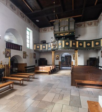 Zdjęcie nr 42: Kościół jest usytuowany w centrum wsi Rudawa, na północ od głównej drogi z Zabierzowa do Chrzanowa. Teren wokół niego jest otoczony wysokim, kamiennym murem z nieregularnych ciosów kamienia, oszkarpowanym, tynkowanym, z wyjątkiem zewnętrznej części muru na zachód od południowej bramki. W murze znajdują się trzy wejścia, od wschodu, południa i zachodu. W części wschodniej muru znajduje się trójosiowa brama wjazdowa, zwieńczona łukiem wklęsło-wypukłym, z trzema przelotami: środkowym wyższym i szerszym, zamkniętym łukiem odcinkowym i bocznymi węższymi i niższymi, zamkniętymi łukiem półkolistym (północne zamurowane). Część środkowa jest flankowana zdwojonymi pilastrami, podtrzymującymi profilowane uskokowe belkowanie z przyczółkiem o profilowanym łuku falistym, zwieńczonym równoramiennym krzyżem. W przyczółku wnęka z figurą św. Floriana. Bramki od strony zachodniej i południowej prostokątne, z przejściem zakończonym płaskim łukiem odcinkowym, z profilowanym gzymsem, zwieńczonym trójkątnym przyczółkiem. Przejścia zamykane drewnianymi ażurowymi i pomalowanymi na ciemnobrązowo jednoskrzydłowymi drzwiami. Poprzez bramkę od zachodu zejście kamiennymi schodami poprowadzonymi wzdłuż muru na dziedziniec plebański, usytuowany poniżej terenu kościelnego. 
W północno-wschodnim narożniku muru niewielka murowana i tynkowana kostnica na planie kwadratu, nakryta dachem namiotowym, łamanym, zakończonym ośmioboczną ślepą latarnią.

Po stronie południowej, poniżej placu kościelnego, do muru przylega murowana, tynkowana, prostokątna i dwukondygnacyjna „zegarowa” wieża bramna nakryta namiotowym dachem z wysoką drewnianą ośmioboczną latarnią o cebulastym hełmie. W wieży znajduje się przejazd wiodący na dziedziniec plebański, z sienią otwartą na przestrzał w dolnej kondygnacji i z lamusem dostępnym od strony placu kościelnego w górnej. 

W południowej części muru, w pobliżu południowo-wschodniego narożnika placu kościelnego, nadbudowana kamienna dzwonnica parawanowa z zawieszonymi czterema dzwonami.  

We wschodniej części placu kościelnego pomiędzy bramką wschodnią a kostnicą znajduje się kamienna ambona, o ośmiobocznej podstawie przechodzącej w szerszy, również ośmioboczny korpus, zakończony kamiennym parapetem, z kamiennymi schodami prowadzącymi na ambonę od strony wschodniej. 

Kościół jest orientowany, prawie w całości zbudowany z cegły, otynkowany z wyjątkiem prezbiterium. Wnętrze kościoła tworzy niewielkie, prostokątne, jednoprzęsłowe prezbiterium zakończone prostą ścianą i nakryte pozornym sklepieniem krzyżowo-żebrowym. Nawa jest szersza, prawie kwadratowa, nakryta drewnianym stropem. Prezbiterium z nawą są połączone szeroką, ostrołukową arkadą w ścianie tęczowej. Od północy do prezbiterium przylega założona na planie prostokąta dwuprzęsłowa zakrystia, nakryta sklepieniem krzyżowym. Wejście do zakrystii zaznaczone gotyckim, kamiennym, sfazowanym portalem zamkniętym łukiem ostrym. Od zachodu do zakrystii przylega niewielkie pomieszczenie gospodarcze, do którego z zakrystii prowadzą ostrołukowe drzwi. Zakrystia oświetlona ostrołukowym oknem w ścianie wschodniej, wypełnionym witrażem z tafelek w kształcie sześciokąta foremnego, ze szkła surowego, tzw. katedralnego. 

Od południa do nawy przylega kaplica o formach renesansowych, dwukondygnacyjna, założona na planie kwadratu. W dolnej kondygnacji sklepiona krzyżowo-żebrowo kruchta otwarta do nawy szeroką, zamkniętą półkoliście arkadą.

Ponad kruchtą kaplica św. Kazimierza, nakryta wspartą na pendentywach kopułą z latarnią. Z kruchty do kaplicy prowadzą kręte kamienne schody umieszczone od zachodu w półkolistej wieżyczce. Prostokątne wejście z krypty na klatkę schodową ujęte kamiennym profilowanym portalem. Kaplica otwarta do nawy szeroką, zamkniętą półkoliście arkadą, o kształcie i wymiarach analogicznych do arkady znajdującej się poniżej. Kaplicę, prócz latarni, oświetla prostokątne okno w ścianie południowej, wypełnione witrażem z tafelek w kształcie gomółek, ze szkła surowego, tzw. katedralnego. Na zachodniej ścianie nawy chór muzyczny, dostępny klatką schodową ukrytą w zewnętrznym aneksie przylegającym do zachodniej elewacji nawy i południowej elewacji wieży-dzwonnicy. 

Nawę i prezbiterium oświetlają umieszczone w południowych ścianach prostokątne, rozglifione okna: jedno w prezbiterium, dwa w nawie. Wszystkie wypełnione witrażami z tafelek w kształcie gomółek, ze szkła surowego, tzw. katedralnego. 

Do kościoła prowadzą dwa wejścia: poprzez arkadę z kruchty południowej oraz szerokie wejście główne prostokątne, zamknięte łukiem odcinkowym, prowadzące do kościoła z obszernej kruchty od strony zachodniej, znajdującej się w murowanym przyziemiu wieży - dzwonnicy. Kruchta, założona na planie kwadratu i nakryta murowanym stropem, doświetlona jest dwoma prostokątnymi oknami umieszczonymi naprzeciw siebie w ścianach północnej i południowej.
 
W zewnętrznej elewacji kościoła widoczny niewysoki kamienny cokół wykonany z nieregularnych ciosów kamienia. Prezbiterium, niższe od nawy, murowane z cegły w układzie wedyjskim, z domieszką układu polskiego. Wschodnie naroża prezbiterium zaakcentowane płaskimi lizenami. We wschodniej ścianie widoczny zarys zamurowanego wydłużonego okna zamkniętego lekko zaostrzonym łukiem, w trójkątnym szczycie znajduje się niewielkie wąskie okienko zakończone łukiem półkolistym. Południowa ściana prezbiterium ozdobiona fryzem z cegieł. Do ściany północnej prezbiterium przylega zakrystia, oszkarpowana, nakryta dachem pulpitowym, z dobudowanym od niej niewielkim aneksem, nakrytym takim samym zadaszeniem. Do wschodniej ściany prezbiterium przylega ogrójec nakryty dachem namiotowym z cebulastym zwieńczeniem, wspartym na sześciu smukłych, profilowanych drewnianych słupach z mieczami, pomiędzy którymi od północy i południa ażurowa drewniana balustrada. 

Nawa oszkarpowana w narożnikach. Elewacje bez podziałów architektonicznych. Od strony południowej do nawy dobudowana dwukondygnacyjna kaplica nakryta kopułą z latarnią, podzielona na dwie kondygnacje. W dolnej kondygnacji od południa wejście do kruchty zaznaczone kamiennym portalem o sfazowanych węgarach i lekko zaostrzonym łuku. Wejście zamykają drewniane dwuskrzydłowe drzwi ozdobione kratownicą z żelaznych listew. Od zachodu do kaplicy przylega półokrągła wieżyczka nakryta daszkiem stożkowym. 

Do zachodniej fasady kościoła dostawiona niska, założona na planie kwadratu trójkondygnacyjna wieża-dzwonnica: w dolnej części murowana, w narożach wzmocniona kamiennymi szkarpami, w górnej drewniana konstrukcji słupowo-ramowej z nadwieszoną izbicą i nakryta dachem półszczytowym. W dolnej, murowanej kondygnacji, na osi kościoła, prostokątne wejście do kruchty zaakcentowane przedsionkiem w kształcie ostrołukowej arkady i czterostopniowymi schodami. Przedsionek nakryty dachem dwuspadowym. Do zachodniej elewacji nawy i południowej elewacji dzwonnicy przylega niewielki, wysoki drewniany aneks, nakryty dachem pulpitowym, mieszczący klatkę schodową prowadzącą na górną kondygnację dzwonnicy i na chór muzyczny w nawie kościoła. Prostokątne wejście w południowej ścianie aneksu, do którego prowadzą pięciostopniowe proste schody. Ponad nimi, na wysokości drugiej kondygnacji dzwonnicy, niewielkie kwadratowe okno. 

Prezbiterium i nawa przykryte stromymi dachami dwuspadowymi, zamkniętymi od wschodu i zachodu szczytami sterczynowymi. Wieżyczka na sygnaturkę ośmioboczna, w dolnej części barokowa, w górnej części nowsza.