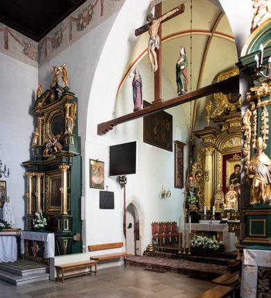 Zdjęcie nr 44: Kościół jest usytuowany w centrum wsi Rudawa, na północ od głównej drogi z Zabierzowa do Chrzanowa. Teren wokół niego jest otoczony wysokim, kamiennym murem z nieregularnych ciosów kamienia, oszkarpowanym, tynkowanym, z wyjątkiem zewnętrznej części muru na zachód od południowej bramki. W murze znajdują się trzy wejścia, od wschodu, południa i zachodu. W części wschodniej muru znajduje się trójosiowa brama wjazdowa, zwieńczona łukiem wklęsło-wypukłym, z trzema przelotami: środkowym wyższym i szerszym, zamkniętym łukiem odcinkowym i bocznymi węższymi i niższymi, zamkniętymi łukiem półkolistym (północne zamurowane). Część środkowa jest flankowana zdwojonymi pilastrami, podtrzymującymi profilowane uskokowe belkowanie z przyczółkiem o profilowanym łuku falistym, zwieńczonym równoramiennym krzyżem. W przyczółku wnęka z figurą św. Floriana. Bramki od strony zachodniej i południowej prostokątne, z przejściem zakończonym płaskim łukiem odcinkowym, z profilowanym gzymsem, zwieńczonym trójkątnym przyczółkiem. Przejścia zamykane drewnianymi ażurowymi i pomalowanymi na ciemnobrązowo jednoskrzydłowymi drzwiami. Poprzez bramkę od zachodu zejście kamiennymi schodami poprowadzonymi wzdłuż muru na dziedziniec plebański, usytuowany poniżej terenu kościelnego. 
W północno-wschodnim narożniku muru niewielka murowana i tynkowana kostnica na planie kwadratu, nakryta dachem namiotowym, łamanym, zakończonym ośmioboczną ślepą latarnią.

Po stronie południowej, poniżej placu kościelnego, do muru przylega murowana, tynkowana, prostokątna i dwukondygnacyjna „zegarowa” wieża bramna nakryta namiotowym dachem z wysoką drewnianą ośmioboczną latarnią o cebulastym hełmie. W wieży znajduje się przejazd wiodący na dziedziniec plebański, z sienią otwartą na przestrzał w dolnej kondygnacji i z lamusem dostępnym od strony placu kościelnego w górnej. 

W południowej części muru, w pobliżu południowo-wschodniego narożnika placu kościelnego, nadbudowana kamienna dzwonnica parawanowa z zawieszonymi czterema dzwonami.  

We wschodniej części placu kościelnego pomiędzy bramką wschodnią a kostnicą znajduje się kamienna ambona, o ośmiobocznej podstawie przechodzącej w szerszy, również ośmioboczny korpus, zakończony kamiennym parapetem, z kamiennymi schodami prowadzącymi na ambonę od strony wschodniej. 

Kościół jest orientowany, prawie w całości zbudowany z cegły, otynkowany z wyjątkiem prezbiterium. Wnętrze kościoła tworzy niewielkie, prostokątne, jednoprzęsłowe prezbiterium zakończone prostą ścianą i nakryte pozornym sklepieniem krzyżowo-żebrowym. Nawa jest szersza, prawie kwadratowa, nakryta drewnianym stropem. Prezbiterium z nawą są połączone szeroką, ostrołukową arkadą w ścianie tęczowej. Od północy do prezbiterium przylega założona na planie prostokąta dwuprzęsłowa zakrystia, nakryta sklepieniem krzyżowym. Wejście do zakrystii zaznaczone gotyckim, kamiennym, sfazowanym portalem zamkniętym łukiem ostrym. Od zachodu do zakrystii przylega niewielkie pomieszczenie gospodarcze, do którego z zakrystii prowadzą ostrołukowe drzwi. Zakrystia oświetlona ostrołukowym oknem w ścianie wschodniej, wypełnionym witrażem z tafelek w kształcie sześciokąta foremnego, ze szkła surowego, tzw. katedralnego. 

Od południa do nawy przylega kaplica o formach renesansowych, dwukondygnacyjna, założona na planie kwadratu. W dolnej kondygnacji sklepiona krzyżowo-żebrowo kruchta otwarta do nawy szeroką, zamkniętą półkoliście arkadą.

Ponad kruchtą kaplica św. Kazimierza, nakryta wspartą na pendentywach kopułą z latarnią. Z kruchty do kaplicy prowadzą kręte kamienne schody umieszczone od zachodu w półkolistej wieżyczce. Prostokątne wejście z krypty na klatkę schodową ujęte kamiennym profilowanym portalem. Kaplica otwarta do nawy szeroką, zamkniętą półkoliście arkadą, o kształcie i wymiarach analogicznych do arkady znajdującej się poniżej. Kaplicę, prócz latarni, oświetla prostokątne okno w ścianie południowej, wypełnione witrażem z tafelek w kształcie gomółek, ze szkła surowego, tzw. katedralnego. Na zachodniej ścianie nawy chór muzyczny, dostępny klatką schodową ukrytą w zewnętrznym aneksie przylegającym do zachodniej elewacji nawy i południowej elewacji wieży-dzwonnicy. 

Nawę i prezbiterium oświetlają umieszczone w południowych ścianach prostokątne, rozglifione okna: jedno w prezbiterium, dwa w nawie. Wszystkie wypełnione witrażami z tafelek w kształcie gomółek, ze szkła surowego, tzw. katedralnego. 

Do kościoła prowadzą dwa wejścia: poprzez arkadę z kruchty południowej oraz szerokie wejście główne prostokątne, zamknięte łukiem odcinkowym, prowadzące do kościoła z obszernej kruchty od strony zachodniej, znajdującej się w murowanym przyziemiu wieży - dzwonnicy. Kruchta, założona na planie kwadratu i nakryta murowanym stropem, doświetlona jest dwoma prostokątnymi oknami umieszczonymi naprzeciw siebie w ścianach północnej i południowej.
 
W zewnętrznej elewacji kościoła widoczny niewysoki kamienny cokół wykonany z nieregularnych ciosów kamienia. Prezbiterium, niższe od nawy, murowane z cegły w układzie wedyjskim, z domieszką układu polskiego. Wschodnie naroża prezbiterium zaakcentowane płaskimi lizenami. We wschodniej ścianie widoczny zarys zamurowanego wydłużonego okna zamkniętego lekko zaostrzonym łukiem, w trójkątnym szczycie znajduje się niewielkie wąskie okienko zakończone łukiem półkolistym. Południowa ściana prezbiterium ozdobiona fryzem z cegieł. Do ściany północnej prezbiterium przylega zakrystia, oszkarpowana, nakryta dachem pulpitowym, z dobudowanym od niej niewielkim aneksem, nakrytym takim samym zadaszeniem. Do wschodniej ściany prezbiterium przylega ogrójec nakryty dachem namiotowym z cebulastym zwieńczeniem, wspartym na sześciu smukłych, profilowanych drewnianych słupach z mieczami, pomiędzy którymi od północy i południa ażurowa drewniana balustrada. 

Nawa oszkarpowana w narożnikach. Elewacje bez podziałów architektonicznych. Od strony południowej do nawy dobudowana dwukondygnacyjna kaplica nakryta kopułą z latarnią, podzielona na dwie kondygnacje. W dolnej kondygnacji od południa wejście do kruchty zaznaczone kamiennym portalem o sfazowanych węgarach i lekko zaostrzonym łuku. Wejście zamykają drewniane dwuskrzydłowe drzwi ozdobione kratownicą z żelaznych listew. Od zachodu do kaplicy przylega półokrągła wieżyczka nakryta daszkiem stożkowym. 

Do zachodniej fasady kościoła dostawiona niska, założona na planie kwadratu trójkondygnacyjna wieża-dzwonnica: w dolnej części murowana, w narożach wzmocniona kamiennymi szkarpami, w górnej drewniana konstrukcji słupowo-ramowej z nadwieszoną izbicą i nakryta dachem półszczytowym. W dolnej, murowanej kondygnacji, na osi kościoła, prostokątne wejście do kruchty zaakcentowane przedsionkiem w kształcie ostrołukowej arkady i czterostopniowymi schodami. Przedsionek nakryty dachem dwuspadowym. Do zachodniej elewacji nawy i południowej elewacji dzwonnicy przylega niewielki, wysoki drewniany aneks, nakryty dachem pulpitowym, mieszczący klatkę schodową prowadzącą na górną kondygnację dzwonnicy i na chór muzyczny w nawie kościoła. Prostokątne wejście w południowej ścianie aneksu, do którego prowadzą pięciostopniowe proste schody. Ponad nimi, na wysokości drugiej kondygnacji dzwonnicy, niewielkie kwadratowe okno. 

Prezbiterium i nawa przykryte stromymi dachami dwuspadowymi, zamkniętymi od wschodu i zachodu szczytami sterczynowymi. Wieżyczka na sygnaturkę ośmioboczna, w dolnej części barokowa, w górnej części nowsza.