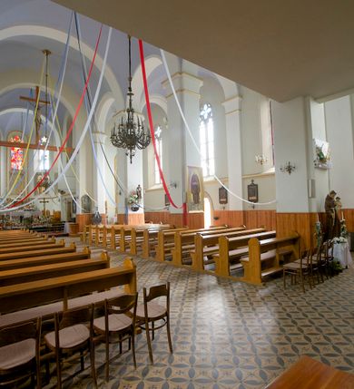 Zdjęcie nr 30: Kościół orientowany, murowany, trójnawowy, czteroprzęsłowy, z jednoprzęsłowym prezbiterium zakończonym wielobocznie. Do prezbiterium dostawione symetrycznie aneksy, od zachodu kruchta, w przyziemiu wieża flankowana dwiema klatkami schodowymi (pomieszczeniem gospodarczym?). Nawy oddzielone od siebie masywnymi filarami opilastrowanymi, z uproszczonymi kapitelami, podtrzymującymi arkady. Nawy i prezbiterium nakryte sklepieniem krzyżowym na gurtach, pięcioboczne zamknięcie prezbiterium sklepieniem parasolowatym. Nawę i prezbiterium oświetlają wysokie, prostokątne okna zakończone półkoliście z oknami trójrzędowymi dwuosiowymi, zakończonymi maswerkami. Układ komunikacyjny zaznaczony kamiennymi portalami o sfazowanych węgarach. Do kościoła prowadzą duże prostokątne drzwi, w kruchcie zakończone półkoliście. Tam też prostokątne wejścia do aneksów bocznych. W południowo-zachodniej ścianie prostokątne wejście zamknięte ściętym łukiem nadwieszonym. Takie samo wejście do aneksu południowego przy prezbiterium. Do aneksu północnego przy prezbiterium prostokątne wejście zamknięte łukiem odcinkowym, ujęte kamiennym portalem, zamkniętym półkoliście. Wejście w ścianie nawy południowej zaznaczone kamiennym portalem zamkniętym łukiem ostrym. W skrajnym przęśle nawy od zachodu chór muzyczny wsparty na dwóch filarach międzynawowych. W części chóru nad kruchtą wnęka otwarta kamienną rozetą. Fasada kościoła trójosiowa, dwukondygnacyjna, ujęta szkarpami z uskokami. Szkarpy z uskokami wydzielają także środkową oś fasady. W jej dolnej kondygnacji znajduje się kamienny portal główny, ujęty uskokowo ustawionymi półkolumnami i zakończony półkolistym tympanonem wypełnionym płaskorzeźbą ze sceną Zesłania Ducha Świętego. Powyżej wypełniona maswerkiem rozeta w profilowanej ramie. Między nią a biforium niewielki herb rodziny Potockich. Szczyt dekoruje fryz arkadkowy. W osiach bocznych wysokie, dwudzielne okna z maswerkiem. Budynek ustawiony na kamiennym cokole, oszkarpowany, z kamiennymi detalami, dekorowany fryzem arkadkowym, z otwartym od zewnątrz obejściem prezbiterium. W obejściu płaskorzeźbiona grupa Ukrzyżowania. Dachy kryte blachą – nawy i wieży dwuspadowe, przybudówek przy prezbiterium pulpitowe, nad obejściem i prezbiterium wieloboczne. Na kalenicy wieżyczka na sygnaturkę z latarnią i wielobocznym dachem. 