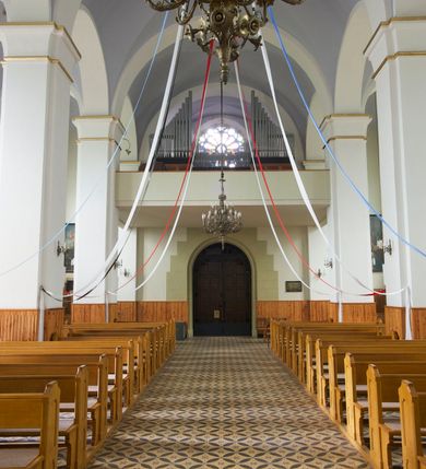 Zdjęcie nr 26: Kościół orientowany, murowany, trójnawowy, czteroprzęsłowy, z jednoprzęsłowym prezbiterium zakończonym wielobocznie. Do prezbiterium dostawione symetrycznie aneksy, od zachodu kruchta, w przyziemiu wieża flankowana dwiema klatkami schodowymi (pomieszczeniem gospodarczym?). Nawy oddzielone od siebie masywnymi filarami opilastrowanymi, z uproszczonymi kapitelami, podtrzymującymi arkady. Nawy i prezbiterium nakryte sklepieniem krzyżowym na gurtach, pięcioboczne zamknięcie prezbiterium sklepieniem parasolowatym. Nawę i prezbiterium oświetlają wysokie, prostokątne okna zakończone półkoliście z oknami trójrzędowymi dwuosiowymi, zakończonymi maswerkami. Układ komunikacyjny zaznaczony kamiennymi portalami o sfazowanych węgarach. Do kościoła prowadzą duże prostokątne drzwi, w kruchcie zakończone półkoliście. Tam też prostokątne wejścia do aneksów bocznych. W południowo-zachodniej ścianie prostokątne wejście zamknięte ściętym łukiem nadwieszonym. Takie samo wejście do aneksu południowego przy prezbiterium. Do aneksu północnego przy prezbiterium prostokątne wejście zamknięte łukiem odcinkowym, ujęte kamiennym portalem, zamkniętym półkoliście. Wejście w ścianie nawy południowej zaznaczone kamiennym portalem zamkniętym łukiem ostrym. W skrajnym przęśle nawy od zachodu chór muzyczny wsparty na dwóch filarach międzynawowych. W części chóru nad kruchtą wnęka otwarta kamienną rozetą. Fasada kościoła trójosiowa, dwukondygnacyjna, ujęta szkarpami z uskokami. Szkarpy z uskokami wydzielają także środkową oś fasady. W jej dolnej kondygnacji znajduje się kamienny portal główny, ujęty uskokowo ustawionymi półkolumnami i zakończony półkolistym tympanonem wypełnionym płaskorzeźbą ze sceną Zesłania Ducha Świętego. Powyżej wypełniona maswerkiem rozeta w profilowanej ramie. Między nią a biforium niewielki herb rodziny Potockich. Szczyt dekoruje fryz arkadkowy. W osiach bocznych wysokie, dwudzielne okna z maswerkiem. Budynek ustawiony na kamiennym cokole, oszkarpowany, z kamiennymi detalami, dekorowany fryzem arkadkowym, z otwartym od zewnątrz obejściem prezbiterium. W obejściu płaskorzeźbiona grupa Ukrzyżowania. Dachy kryte blachą – nawy i wieży dwuspadowe, przybudówek przy prezbiterium pulpitowe, nad obejściem i prezbiterium wieloboczne. Na kalenicy wieżyczka na sygnaturkę z latarnią i wielobocznym dachem. 