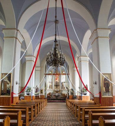 Zdjęcie nr 35: Kościół orientowany, murowany, trójnawowy, czteroprzęsłowy, z jednoprzęsłowym prezbiterium zakończonym wielobocznie. Do prezbiterium dostawione symetrycznie aneksy, od zachodu kruchta, w przyziemiu wieża flankowana dwiema klatkami schodowymi (pomieszczeniem gospodarczym?). Nawy oddzielone od siebie masywnymi filarami opilastrowanymi, z uproszczonymi kapitelami, podtrzymującymi arkady. Nawy i prezbiterium nakryte sklepieniem krzyżowym na gurtach, pięcioboczne zamknięcie prezbiterium sklepieniem parasolowatym. Nawę i prezbiterium oświetlają wysokie, prostokątne okna zakończone półkoliście z oknami trójrzędowymi dwuosiowymi, zakończonymi maswerkami. Układ komunikacyjny zaznaczony kamiennymi portalami o sfazowanych węgarach. Do kościoła prowadzą duże prostokątne drzwi, w kruchcie zakończone półkoliście. Tam też prostokątne wejścia do aneksów bocznych. W południowo-zachodniej ścianie prostokątne wejście zamknięte ściętym łukiem nadwieszonym. Takie samo wejście do aneksu południowego przy prezbiterium. Do aneksu północnego przy prezbiterium prostokątne wejście zamknięte łukiem odcinkowym, ujęte kamiennym portalem, zamkniętym półkoliście. Wejście w ścianie nawy południowej zaznaczone kamiennym portalem zamkniętym łukiem ostrym. W skrajnym przęśle nawy od zachodu chór muzyczny wsparty na dwóch filarach międzynawowych. W części chóru nad kruchtą wnęka otwarta kamienną rozetą. Fasada kościoła trójosiowa, dwukondygnacyjna, ujęta szkarpami z uskokami. Szkarpy z uskokami wydzielają także środkową oś fasady. W jej dolnej kondygnacji znajduje się kamienny portal główny, ujęty uskokowo ustawionymi półkolumnami i zakończony półkolistym tympanonem wypełnionym płaskorzeźbą ze sceną Zesłania Ducha Świętego. Powyżej wypełniona maswerkiem rozeta w profilowanej ramie. Między nią a biforium niewielki herb rodziny Potockich. Szczyt dekoruje fryz arkadkowy. W osiach bocznych wysokie, dwudzielne okna z maswerkiem. Budynek ustawiony na kamiennym cokole, oszkarpowany, z kamiennymi detalami, dekorowany fryzem arkadkowym, z otwartym od zewnątrz obejściem prezbiterium. W obejściu płaskorzeźbiona grupa Ukrzyżowania. Dachy kryte blachą – nawy i wieży dwuspadowe, przybudówek przy prezbiterium pulpitowe, nad obejściem i prezbiterium wieloboczne. Na kalenicy wieżyczka na sygnaturkę z latarnią i wielobocznym dachem. 