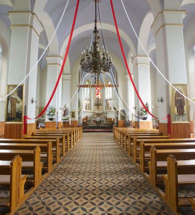 Zdjęcie nr 32: Kościół orientowany, murowany, trójnawowy, czteroprzęsłowy, z jednoprzęsłowym prezbiterium zakończonym wielobocznie. Do prezbiterium dostawione symetrycznie aneksy, od zachodu kruchta, w przyziemiu wieża flankowana dwiema klatkami schodowymi (pomieszczeniem gospodarczym?). Nawy oddzielone od siebie masywnymi filarami opilastrowanymi, z uproszczonymi kapitelami, podtrzymującymi arkady. Nawy i prezbiterium nakryte sklepieniem krzyżowym na gurtach, pięcioboczne zamknięcie prezbiterium sklepieniem parasolowatym. Nawę i prezbiterium oświetlają wysokie, prostokątne okna zakończone półkoliście z oknami trójrzędowymi dwuosiowymi, zakończonymi maswerkami. Układ komunikacyjny zaznaczony kamiennymi portalami o sfazowanych węgarach. Do kościoła prowadzą duże prostokątne drzwi, w kruchcie zakończone półkoliście. Tam też prostokątne wejścia do aneksów bocznych. W południowo-zachodniej ścianie prostokątne wejście zamknięte ściętym łukiem nadwieszonym. Takie samo wejście do aneksu południowego przy prezbiterium. Do aneksu północnego przy prezbiterium prostokątne wejście zamknięte łukiem odcinkowym, ujęte kamiennym portalem, zamkniętym półkoliście. Wejście w ścianie nawy południowej zaznaczone kamiennym portalem zamkniętym łukiem ostrym. W skrajnym przęśle nawy od zachodu chór muzyczny wsparty na dwóch filarach międzynawowych. W części chóru nad kruchtą wnęka otwarta kamienną rozetą. Fasada kościoła trójosiowa, dwukondygnacyjna, ujęta szkarpami z uskokami. Szkarpy z uskokami wydzielają także środkową oś fasady. W jej dolnej kondygnacji znajduje się kamienny portal główny, ujęty uskokowo ustawionymi półkolumnami i zakończony półkolistym tympanonem wypełnionym płaskorzeźbą ze sceną Zesłania Ducha Świętego. Powyżej wypełniona maswerkiem rozeta w profilowanej ramie. Między nią a biforium niewielki herb rodziny Potockich. Szczyt dekoruje fryz arkadkowy. W osiach bocznych wysokie, dwudzielne okna z maswerkiem. Budynek ustawiony na kamiennym cokole, oszkarpowany, z kamiennymi detalami, dekorowany fryzem arkadkowym, z otwartym od zewnątrz obejściem prezbiterium. W obejściu płaskorzeźbiona grupa Ukrzyżowania. Dachy kryte blachą – nawy i wieży dwuspadowe, przybudówek przy prezbiterium pulpitowe, nad obejściem i prezbiterium wieloboczne. Na kalenicy wieżyczka na sygnaturkę z latarnią i wielobocznym dachem. 