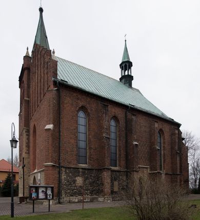 Zdjęcie nr 4: Kościół położony na obszernym placu przylegającym do wschodniej pierzei rynku, na północ od zamku. Plac otoczony ceglanym murem z filarkami. Przed kościołem wydzielony plac, dawny cmentarz, na nim figura św. Jana Kantego. W południowo-wschodnim narożu placu grobowiec księżnej Apolonii Potockiej. Kościół orientowany, halowy, trójnawowy, czteroprzęsłowy, z dwuprzęsłowym zamkniętym wielobocznie prezbiterium. Nawa główna szersza od naw bocznych. Nawy boczne zakończone od wschodu poligonalnymi kaplicami. Od strony północnej do nawy przylega kruchta. W północno-zachodnim narożniku kwadratowa wieża mieszcząca kaplicę w przyziemiu. Do zachodniego przęsła nawy głównej dostawiony głęboki ryzalit z kruchtą w przyziemiu i chórem na piętrze z prospektem organowym. Od północnej strony przylega piętrowa zakrystia, zamknięta wielobocznie. Nawa główna od bocznych oddzielona czworobocznymi filarami o ściętych narożach. Prezbiterium otwarte do korpusu ostrołukową tęczą. W korpusie sklepienie o konstrukcji żelbetowej, stylizowane na gotyckie. W kaplicy pod wieżą sklepienie kolebkowe, w kruchcie zachodniej sufit. Prezbiterium nakryte sklepieniem krzyżowo-żebrowym z żebrami spływającymi na konsole. Wnętrze oświetlają okna ostrołukowe, wypełnione witrażami; dwa w zamknięciu prezbiterium (środkowy otwór zamurowany), dwa na ścianie południowej. Portal z prezbiterium do zakrystii zamknięty łukiem w ośli grzbiet. Otwory drzwiowe prostokątne, różnej wielkości. Kaplica pod wieżą otwarta do wnętrza ostrołukowymi arkadami. Otwory okienne wąskie, prostokątne, ostrołukowe, wypełnione witrażem; cztery w ścianie północnej i południowej, jedno, szersze w ścianie zachodniej nad chórem. Wieża oświetlona małymi, wąskimi oknami zakończonymi łukiem odcinkowym i ostrołukowym. Fasada jednoosiowa, dwukondygnacyjna, zwieńczona szczytem schodkowym z ceglanymi laskami. Niesymetrycznie umieszczone wejście ujęte kamiennym, profilowanym portalem, zamkniętym ostrołukowo. Ponad nim rozglifione ostrołukowe okno. Od północy wieża wbudowana w naroże kościoła, wysunięta nieco przed lico fasady. W dolnej partii kamienna, w górnej ceglana, na rzucie prostokąta, czterokondygnacyjna. Piętro pierwsze i drugie oddzielone kamiennym gzymsem. Trzy dolne kondygnacje gotyckie, czwarta neogotycka (projektu Franciszka Marii Lanciego z 1836 r). Na osi pojedyncze okna. W parterze okno ciosowe, prostokątne, ponad nim wmurowany późnogotycki maswerk ostrołukowy z motywami rybich pęcherzy i psiego zęba, wyżej kartusz z herbem Leliwa. Na pierwszym piętrze okno ostrołukowe z parapetem na konsolkach, w opasce ceglanej zamkniętej ostrołukiem wklęsłym. Drugie piętro, okno ostrołukowe w opasce kamiennej, ponad nim okrągła tarcza zegarowa. Ostatnia kondygnacja ze ściętymi narożami, na których wysunięte przed lico muru krenelażowe wieżyczki zwieńczone kamiennymi szczytami w formie ostrosłupów. Od zachodu masywny łuk półokrągły uformowany z kształtek ceramicznych, w jego polu triforium ostrołukowe. Ponad nim okulus. Pod okapem dachu fryz z ceglanych konsolek oraz gąsiory układane w motyw rybiej łuski. Dach iglicowy. Elewacja południowa. Portal kamienny na cokole, profilowany, ostrołukowy. Archiwolty przechodzące w łuk o formie oślego grzbietu, wsparte na konsolkach zdobionych motywem roślinnym. Skrajna archiwolta z czołgankami zwieńczona pinaklem z kwiatonem. Po bokach analogiczne pinakle; W prezbiterium portal kamienny na cokole, profilowany, ostrołukowy, z dekoracją z motywem skręconego sznura; w kluczu herb Odrowąż, oraz data 1767 i litery LG OH OFP. W ścianę korpusu wmurowane kamienne epitafium ks. Pawła Gabańskiego plebana zatorskiego (zm. 1825), nad nim kartusz z herbem Łodzia.Trzy okna analogiczne jak w fasadzie, i jedno o połowę węższe. Elewacja północna. Kruchta ceglana, na cokole, opięta przyporami. Na osi portal kamienny, profilowany, ostrołukowy. Ponad nim kamienna rozeta z monogramem Marii, po bokach dwa okna o wykroju czworoliścia w okrągłych, kamiennych opaskach. Od strony północno-zachodniej zakrystia na rzucie prostokąta, zamknięta wielobocznie, piętrowa, w dolnej części kamienna (pozostałość pierwotnego kościoła), wyżej ceglana (piętro dobudowane 1915 r.). Od północy portal w opasce ceglanej, zamknięty łukiem odcinkowym. Ponad nim ostrołukowe, ceglane okno. Dwa okna analogiczne jak w fasadzie i jedno o połowę węższe. Kościół opięty przyporami, na wysokości ław okiennych gzyms kapnikowy wyłamany nad portalem północnym. Przypory z kapnikami w zwieńczeniu i na 2/3 wysokości. Pod dachem gzyms konsolkowy. Dach dwuspadowy, sygnaturka wieloboczna z ostrołukowymi prześwitami, zwieńczona hełmem iglicowym.