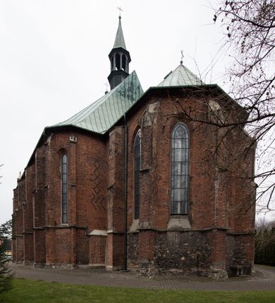 Zdjęcie nr 6: Kościół położony na obszernym placu przylegającym do wschodniej pierzei rynku, na północ od zamku. Plac otoczony ceglanym murem z filarkami. Przed kościołem wydzielony plac, dawny cmentarz, na nim figura św. Jana Kantego. W południowo-wschodnim narożu placu grobowiec księżnej Apolonii Potockiej. Kościół orientowany, halowy, trójnawowy, czteroprzęsłowy, z dwuprzęsłowym zamkniętym wielobocznie prezbiterium. Nawa główna szersza od naw bocznych. Nawy boczne zakończone od wschodu poligonalnymi kaplicami. Od strony północnej do nawy przylega kruchta. W północno-zachodnim narożniku kwadratowa wieża mieszcząca kaplicę w przyziemiu. Do zachodniego przęsła nawy głównej dostawiony głęboki ryzalit z kruchtą w przyziemiu i chórem na piętrze z prospektem organowym. Od północnej strony przylega piętrowa zakrystia, zamknięta wielobocznie. Nawa główna od bocznych oddzielona czworobocznymi filarami o ściętych narożach. Prezbiterium otwarte do korpusu ostrołukową tęczą. W korpusie sklepienie o konstrukcji żelbetowej, stylizowane na gotyckie. W kaplicy pod wieżą sklepienie kolebkowe, w kruchcie zachodniej sufit. Prezbiterium nakryte sklepieniem krzyżowo-żebrowym z żebrami spływającymi na konsole. Wnętrze oświetlają okna ostrołukowe, wypełnione witrażami; dwa w zamknięciu prezbiterium (środkowy otwór zamurowany), dwa na ścianie południowej. Portal z prezbiterium do zakrystii zamknięty łukiem w ośli grzbiet. Otwory drzwiowe prostokątne, różnej wielkości. Kaplica pod wieżą otwarta do wnętrza ostrołukowymi arkadami. Otwory okienne wąskie, prostokątne, ostrołukowe, wypełnione witrażem; cztery w ścianie północnej i południowej, jedno, szersze w ścianie zachodniej nad chórem. Wieża oświetlona małymi, wąskimi oknami zakończonymi łukiem odcinkowym i ostrołukowym. Fasada jednoosiowa, dwukondygnacyjna, zwieńczona szczytem schodkowym z ceglanymi laskami. Niesymetrycznie umieszczone wejście ujęte kamiennym, profilowanym portalem, zamkniętym ostrołukowo. Ponad nim rozglifione ostrołukowe okno. Od północy wieża wbudowana w naroże kościoła, wysunięta nieco przed lico fasady. W dolnej partii kamienna, w górnej ceglana, na rzucie prostokąta, czterokondygnacyjna. Piętro pierwsze i drugie oddzielone kamiennym gzymsem. Trzy dolne kondygnacje gotyckie, czwarta neogotycka (projektu Franciszka Marii Lanciego z 1836 r). Na osi pojedyncze okna. W parterze okno ciosowe, prostokątne, ponad nim wmurowany późnogotycki maswerk ostrołukowy z motywami rybich pęcherzy i psiego zęba, wyżej kartusz z herbem Leliwa. Na pierwszym piętrze okno ostrołukowe z parapetem na konsolkach, w opasce ceglanej zamkniętej ostrołukiem wklęsłym. Drugie piętro, okno ostrołukowe w opasce kamiennej, ponad nim okrągła tarcza zegarowa. Ostatnia kondygnacja ze ściętymi narożami, na których wysunięte przed lico muru krenelażowe wieżyczki zwieńczone kamiennymi szczytami w formie ostrosłupów. Od zachodu masywny łuk półokrągły uformowany z kształtek ceramicznych, w jego polu triforium ostrołukowe. Ponad nim okulus. Pod okapem dachu fryz z ceglanych konsolek oraz gąsiory układane w motyw rybiej łuski. Dach iglicowy. Elewacja południowa. Portal kamienny na cokole, profilowany, ostrołukowy. Archiwolty przechodzące w łuk o formie oślego grzbietu, wsparte na konsolkach zdobionych motywem roślinnym. Skrajna archiwolta z czołgankami zwieńczona pinaklem z kwiatonem. Po bokach analogiczne pinakle; W prezbiterium portal kamienny na cokole, profilowany, ostrołukowy, z dekoracją z motywem skręconego sznura; w kluczu herb Odrowąż, oraz data 1767 i litery LG OH OFP. W ścianę korpusu wmurowane kamienne epitafium ks. Pawła Gabańskiego plebana zatorskiego (zm. 1825), nad nim kartusz z herbem Łodzia.Trzy okna analogiczne jak w fasadzie, i jedno o połowę węższe. Elewacja północna. Kruchta ceglana, na cokole, opięta przyporami. Na osi portal kamienny, profilowany, ostrołukowy. Ponad nim kamienna rozeta z monogramem Marii, po bokach dwa okna o wykroju czworoliścia w okrągłych, kamiennych opaskach. Od strony północno-zachodniej zakrystia na rzucie prostokąta, zamknięta wielobocznie, piętrowa, w dolnej części kamienna (pozostałość pierwotnego kościoła), wyżej ceglana (piętro dobudowane 1915 r.). Od północy portal w opasce ceglanej, zamknięty łukiem odcinkowym. Ponad nim ostrołukowe, ceglane okno. Dwa okna analogiczne jak w fasadzie i jedno o połowę węższe. Kościół opięty przyporami, na wysokości ław okiennych gzyms kapnikowy wyłamany nad portalem północnym. Przypory z kapnikami w zwieńczeniu i na 2/3 wysokości. Pod dachem gzyms konsolkowy. Dach dwuspadowy, sygnaturka wieloboczna z ostrołukowymi prześwitami, zwieńczona hełmem iglicowym.