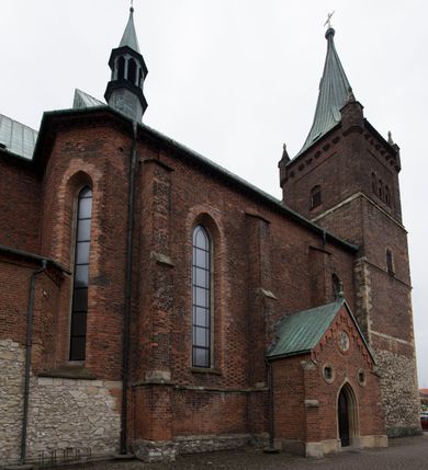 Zdjęcie nr 5: Kościół położony na obszernym placu przylegającym do wschodniej pierzei rynku, na północ od zamku. Plac otoczony ceglanym murem z filarkami. Przed kościołem wydzielony plac, dawny cmentarz, na nim figura św. Jana Kantego. W południowo-wschodnim narożu placu grobowiec księżnej Apolonii Potockiej. Kościół orientowany, halowy, trójnawowy, czteroprzęsłowy, z dwuprzęsłowym zamkniętym wielobocznie prezbiterium. Nawa główna szersza od naw bocznych. Nawy boczne zakończone od wschodu poligonalnymi kaplicami. Od strony północnej do nawy przylega kruchta. W północno-zachodnim narożniku kwadratowa wieża mieszcząca kaplicę w przyziemiu. Do zachodniego przęsła nawy głównej dostawiony głęboki ryzalit z kruchtą w przyziemiu i chórem na piętrze z prospektem organowym. Od północnej strony przylega piętrowa zakrystia, zamknięta wielobocznie. Nawa główna od bocznych oddzielona czworobocznymi filarami o ściętych narożach. Prezbiterium otwarte do korpusu ostrołukową tęczą. W korpusie sklepienie o konstrukcji żelbetowej, stylizowane na gotyckie. W kaplicy pod wieżą sklepienie kolebkowe, w kruchcie zachodniej sufit. Prezbiterium nakryte sklepieniem krzyżowo-żebrowym z żebrami spływającymi na konsole. Wnętrze oświetlają okna ostrołukowe, wypełnione witrażami; dwa w zamknięciu prezbiterium (środkowy otwór zamurowany), dwa na ścianie południowej. Portal z prezbiterium do zakrystii zamknięty łukiem w ośli grzbiet. Otwory drzwiowe prostokątne, różnej wielkości. Kaplica pod wieżą otwarta do wnętrza ostrołukowymi arkadami. Otwory okienne wąskie, prostokątne, ostrołukowe, wypełnione witrażem; cztery w ścianie północnej i południowej, jedno, szersze w ścianie zachodniej nad chórem. Wieża oświetlona małymi, wąskimi oknami zakończonymi łukiem odcinkowym i ostrołukowym. Fasada jednoosiowa, dwukondygnacyjna, zwieńczona szczytem schodkowym z ceglanymi laskami. Niesymetrycznie umieszczone wejście ujęte kamiennym, profilowanym portalem, zamkniętym ostrołukowo. Ponad nim rozglifione ostrołukowe okno. Od północy wieża wbudowana w naroże kościoła, wysunięta nieco przed lico fasady. W dolnej partii kamienna, w górnej ceglana, na rzucie prostokąta, czterokondygnacyjna. Piętro pierwsze i drugie oddzielone kamiennym gzymsem. Trzy dolne kondygnacje gotyckie, czwarta neogotycka (projektu Franciszka Marii Lanciego z 1836 r). Na osi pojedyncze okna. W parterze okno ciosowe, prostokątne, ponad nim wmurowany późnogotycki maswerk ostrołukowy z motywami rybich pęcherzy i psiego zęba, wyżej kartusz z herbem Leliwa. Na pierwszym piętrze okno ostrołukowe z parapetem na konsolkach, w opasce ceglanej zamkniętej ostrołukiem wklęsłym. Drugie piętro, okno ostrołukowe w opasce kamiennej, ponad nim okrągła tarcza zegarowa. Ostatnia kondygnacja ze ściętymi narożami, na których wysunięte przed lico muru krenelażowe wieżyczki zwieńczone kamiennymi szczytami w formie ostrosłupów. Od zachodu masywny łuk półokrągły uformowany z kształtek ceramicznych, w jego polu triforium ostrołukowe. Ponad nim okulus. Pod okapem dachu fryz z ceglanych konsolek oraz gąsiory układane w motyw rybiej łuski. Dach iglicowy. Elewacja południowa. Portal kamienny na cokole, profilowany, ostrołukowy. Archiwolty przechodzące w łuk o formie oślego grzbietu, wsparte na konsolkach zdobionych motywem roślinnym. Skrajna archiwolta z czołgankami zwieńczona pinaklem z kwiatonem. Po bokach analogiczne pinakle; W prezbiterium portal kamienny na cokole, profilowany, ostrołukowy, z dekoracją z motywem skręconego sznura; w kluczu herb Odrowąż, oraz data 1767 i litery LG OH OFP. W ścianę korpusu wmurowane kamienne epitafium ks. Pawła Gabańskiego plebana zatorskiego (zm. 1825), nad nim kartusz z herbem Łodzia.Trzy okna analogiczne jak w fasadzie, i jedno o połowę węższe. Elewacja północna. Kruchta ceglana, na cokole, opięta przyporami. Na osi portal kamienny, profilowany, ostrołukowy. Ponad nim kamienna rozeta z monogramem Marii, po bokach dwa okna o wykroju czworoliścia w okrągłych, kamiennych opaskach. Od strony północno-zachodniej zakrystia na rzucie prostokąta, zamknięta wielobocznie, piętrowa, w dolnej części kamienna (pozostałość pierwotnego kościoła), wyżej ceglana (piętro dobudowane 1915 r.). Od północy portal w opasce ceglanej, zamknięty łukiem odcinkowym. Ponad nim ostrołukowe, ceglane okno. Dwa okna analogiczne jak w fasadzie i jedno o połowę węższe. Kościół opięty przyporami, na wysokości ław okiennych gzyms kapnikowy wyłamany nad portalem północnym. Przypory z kapnikami w zwieńczeniu i na 2/3 wysokości. Pod dachem gzyms konsolkowy. Dach dwuspadowy, sygnaturka wieloboczna z ostrołukowymi prześwitami, zwieńczona hełmem iglicowym.