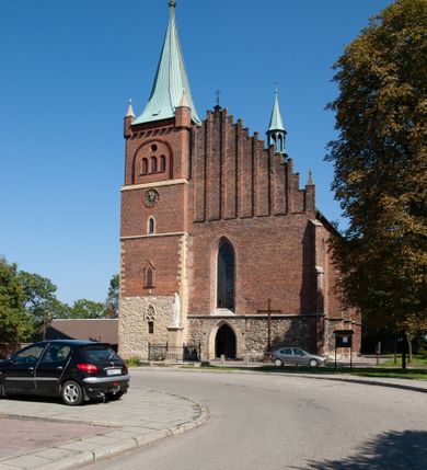 Zdjęcie nr 33: Kościół położony na obszernym placu przylegającym do wschodniej pierzei rynku, na północ od zamku. Plac otoczony ceglanym murem z filarkami. Przed kościołem wydzielony plac, dawny cmentarz, na nim figura św. Jana Kantego. W południowo-wschodnim narożu placu grobowiec księżnej Apolonii Potockiej. Kościół orientowany, halowy, trójnawowy, czteroprzęsłowy, z dwuprzęsłowym zamkniętym wielobocznie prezbiterium. Nawa główna szersza od naw bocznych. Nawy boczne zakończone od wschodu poligonalnymi kaplicami. Od strony północnej do nawy przylega kruchta. W północno-zachodnim narożniku kwadratowa wieża mieszcząca kaplicę w przyziemiu. Do zachodniego przęsła nawy głównej dostawiony głęboki ryzalit z kruchtą w przyziemiu i chórem na piętrze z prospektem organowym. Od północnej strony przylega piętrowa zakrystia, zamknięta wielobocznie. Nawa główna od bocznych oddzielona czworobocznymi filarami o ściętych narożach. Prezbiterium otwarte do korpusu ostrołukową tęczą. W korpusie sklepienie o konstrukcji żelbetowej, stylizowane na gotyckie. W kaplicy pod wieżą sklepienie kolebkowe, w kruchcie zachodniej sufit. Prezbiterium nakryte sklepieniem krzyżowo-żebrowym z żebrami spływającymi na konsole. Wnętrze oświetlają okna ostrołukowe, wypełnione witrażami; dwa w zamknięciu prezbiterium (środkowy otwór zamurowany), dwa na ścianie południowej. Portal z prezbiterium do zakrystii zamknięty łukiem w ośli grzbiet. Otwory drzwiowe prostokątne, różnej wielkości. Kaplica pod wieżą otwarta do wnętrza ostrołukowymi arkadami. Otwory okienne wąskie, prostokątne, ostrołukowe, wypełnione witrażem; cztery w ścianie północnej i południowej, jedno, szersze w ścianie zachodniej nad chórem. Wieża oświetlona małymi, wąskimi oknami zakończonymi łukiem odcinkowym i ostrołukowym. Fasada jednoosiowa, dwukondygnacyjna, zwieńczona szczytem schodkowym z ceglanymi laskami. Niesymetrycznie umieszczone wejście ujęte kamiennym, profilowanym portalem, zamkniętym ostrołukowo. Ponad nim rozglifione ostrołukowe okno. Od północy wieża wbudowana w naroże kościoła, wysunięta nieco przed lico fasady. W dolnej partii kamienna, w górnej ceglana, na rzucie prostokąta, czterokondygnacyjna. Piętro pierwsze i drugie oddzielone kamiennym gzymsem. Trzy dolne kondygnacje gotyckie, czwarta neogotycka (projektu Franciszka Marii Lanciego z 1836 r). Na osi pojedyncze okna. W parterze okno ciosowe, prostokątne, ponad nim wmurowany późnogotycki maswerk ostrołukowy z motywami rybich pęcherzy i psiego zęba, wyżej kartusz z herbem Leliwa. Na pierwszym piętrze okno ostrołukowe z parapetem na konsolkach, w opasce ceglanej zamkniętej ostrołukiem wklęsłym. Drugie piętro, okno ostrołukowe w opasce kamiennej, ponad nim okrągła tarcza zegarowa. Ostatnia kondygnacja ze ściętymi narożami, na których wysunięte przed lico muru krenelażowe wieżyczki zwieńczone kamiennymi szczytami w formie ostrosłupów. Od zachodu masywny łuk półokrągły uformowany z kształtek ceramicznych, w jego polu triforium ostrołukowe. Ponad nim okulus. Pod okapem dachu fryz z ceglanych konsolek oraz gąsiory układane w motyw rybiej łuski. Dach iglicowy. Elewacja południowa. Portal kamienny na cokole, profilowany, ostrołukowy. Archiwolty przechodzące w łuk o formie oślego grzbietu, wsparte na konsolkach zdobionych motywem roślinnym. Skrajna archiwolta z czołgankami zwieńczona pinaklem z kwiatonem. Po bokach analogiczne pinakle; W prezbiterium portal kamienny na cokole, profilowany, ostrołukowy, z dekoracją z motywem skręconego sznura; w kluczu herb Odrowąż, oraz data 1767 i litery LG OH OFP. W ścianę korpusu wmurowane kamienne epitafium ks. Pawła Gabańskiego plebana zatorskiego (zm. 1825), nad nim kartusz z herbem Łodzia.Trzy okna analogiczne jak w fasadzie, i jedno o połowę węższe. Elewacja północna. Kruchta ceglana, na cokole, opięta przyporami. Na osi portal kamienny, profilowany, ostrołukowy. Ponad nim kamienna rozeta z monogramem Marii, po bokach dwa okna o wykroju czworoliścia w okrągłych, kamiennych opaskach. Od strony północno-zachodniej zakrystia na rzucie prostokąta, zamknięta wielobocznie, piętrowa, w dolnej części kamienna (pozostałość pierwotnego kościoła), wyżej ceglana (piętro dobudowane 1915 r.). Od północy portal w opasce ceglanej, zamknięty łukiem odcinkowym. Ponad nim ostrołukowe, ceglane okno. Dwa okna analogiczne jak w fasadzie i jedno o połowę węższe. Kościół opięty przyporami, na wysokości ław okiennych gzyms kapnikowy wyłamany nad portalem północnym. Przypory z kapnikami w zwieńczeniu i na 2/3 wysokości. Pod dachem gzyms konsolkowy. Dach dwuspadowy, sygnaturka wieloboczna z ostrołukowymi prześwitami, zwieńczona hełmem iglicowym.