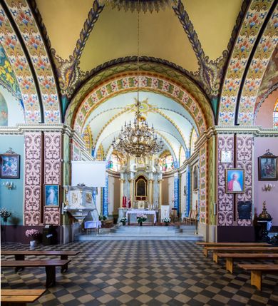 Zdjęcie nr 20: Kościół murowany, jednonawowy, z wieżą częściowo wtopioną w elewację zachodnią składający się z nawy, transeptu, zakrystii od północy z mieszczącym się na piętrze skarbcem i przystawionej od wschodu wieżyczki klatki schodowej oraz kruchty od południa. Prezbiterium dwuprzęsłowe, zamknięte trójbocznie. Nawa główna podzielona masywnymi opilastrowanymi filarami. Sklepienie prezbiterium i nawy kolebkowe z lunetami, skrzyżowania z transeptem. Od południa chór muzyczny mieszczący się między pierwszymi filarami i powyżej kruchty wejściowej. W prezbiterium okna w każdym przęśle, po każdej stronie nawy po dwa, w transepcie po trzy, w kruchcie dwa. Główne wejście od zachodu, kolejne do zakrystii i od południa. Ściany i sklepienia kościoła pokrywa polichromia złożona z geometryzujących dekoracji floralnych. 
Wschodnią elewację frontową kościoła tworzy trójosiowa, wieżowa fasada. Oś kompozycji stanowi wysunięta ryzalitowo dwukondygnacyjna wieża ze ściętymi narożami, które zaakcentowane są poprzez pilastry. Ściana czołowa wieży wypełniona w pierwszej kondygnacji wklęsłą płyciną, z portalem o wykroju prostokątnym, z odcinkiem gzymsu w zwieńczeniu. Ponad nim prostokątne okno zakończone łukiem pełnym. Kondygnacje rozdzielone za pomocą masywnego gzymsu. Druga kondygnacja wieży wypełniona analogicznie prostokątną płyciną, w którą wkomponowany jest wypukły panel w kształcie leżącego prostokąta. Nad nim okno o obramieniu i wykroju identycznym jak w kondygnacji niższej. Całość zwieńczona za pomocą gzymsu podokapowego i baniastego hełmu wieżowego o ściętych narożach, na które nałożona jest kopułka w formie cebulastej. Osie boczne cofnięte w stosunku do wysuniętej wieży i zrytmizowane podziałem ramowym. Tak jak w osi głównej pierwsza kondygnacja wypełniona jest wklęsłą płyciną w formie wydłużonego, stojącego prostokąta. Nad gzymsem trójkątny spływ przysłonięty wieżą. Elewacje boczne i tylna ukształtowane jednorodnie. Zrytmizowane podziałem ramowym i przeprute oknami umieszczonymi w prostokątnych płycinach. Ramiona transeptu oraz prezbiterium zrytmizowane są za pomocą pilastrów załamanych na narożach. Od południa do korpusu przylega niska kruchta. Prowadzi do niej wejście o wykroju prostokątnym z profilowanym w tynku portalem i z odcinkiem gzymsu w zwieńczeniu. Od północy pomiędzy prezbiterium, a ramieniem transeptu wprowadzona została piętrowa przybudówka zakrystii. W elewacji tej partii kościoła brak jest znaczących podziałów. Okna i drzwi tam się znajdujące mają formę stojącego prostokąta i pozbawione są jakichkolwiek obramień. Kościół pokryty dwuspadowym, jednokalenicowym dachem, nad zakrystią i kruchtami umieszczono daszki dwuspadowe. Wieża nakryta jest hełmem cebulastym. Całość pokryta została malowaną blachą.
