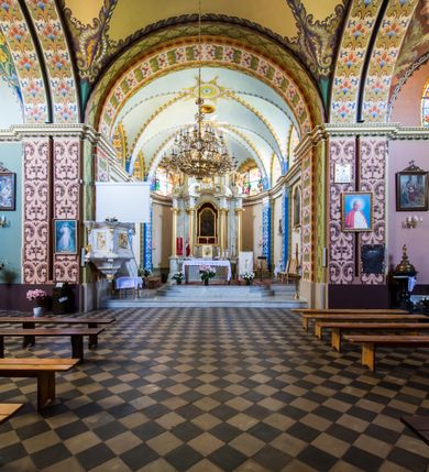 Zdjęcie nr 22: Kościół murowany, jednonawowy, z wieżą częściowo wtopioną w elewację zachodnią składający się z nawy, transeptu, zakrystii od północy z mieszczącym się na piętrze skarbcem i przystawionej od wschodu wieżyczki klatki schodowej oraz kruchty od południa. Prezbiterium dwuprzęsłowe, zamknięte trójbocznie. Nawa główna podzielona masywnymi opilastrowanymi filarami. Sklepienie prezbiterium i nawy kolebkowe z lunetami, skrzyżowania z transeptem. Od południa chór muzyczny mieszczący się między pierwszymi filarami i powyżej kruchty wejściowej. W prezbiterium okna w każdym przęśle, po każdej stronie nawy po dwa, w transepcie po trzy, w kruchcie dwa. Główne wejście od zachodu, kolejne do zakrystii i od południa. Ściany i sklepienia kościoła pokrywa polichromia złożona z geometryzujących dekoracji floralnych. 
Wschodnią elewację frontową kościoła tworzy trójosiowa, wieżowa fasada. Oś kompozycji stanowi wysunięta ryzalitowo dwukondygnacyjna wieża ze ściętymi narożami, które zaakcentowane są poprzez pilastry. Ściana czołowa wieży wypełniona w pierwszej kondygnacji wklęsłą płyciną, z portalem o wykroju prostokątnym, z odcinkiem gzymsu w zwieńczeniu. Ponad nim prostokątne okno zakończone łukiem pełnym. Kondygnacje rozdzielone za pomocą masywnego gzymsu. Druga kondygnacja wieży wypełniona analogicznie prostokątną płyciną, w którą wkomponowany jest wypukły panel w kształcie leżącego prostokąta. Nad nim okno o obramieniu i wykroju identycznym jak w kondygnacji niższej. Całość zwieńczona za pomocą gzymsu podokapowego i baniastego hełmu wieżowego o ściętych narożach, na które nałożona jest kopułka w formie cebulastej. Osie boczne cofnięte w stosunku do wysuniętej wieży i zrytmizowane podziałem ramowym. Tak jak w osi głównej pierwsza kondygnacja wypełniona jest wklęsłą płyciną w formie wydłużonego, stojącego prostokąta. Nad gzymsem trójkątny spływ przysłonięty wieżą. Elewacje boczne i tylna ukształtowane jednorodnie. Zrytmizowane podziałem ramowym i przeprute oknami umieszczonymi w prostokątnych płycinach. Ramiona transeptu oraz prezbiterium zrytmizowane są za pomocą pilastrów załamanych na narożach. Od południa do korpusu przylega niska kruchta. Prowadzi do niej wejście o wykroju prostokątnym z profilowanym w tynku portalem i z odcinkiem gzymsu w zwieńczeniu. Od północy pomiędzy prezbiterium, a ramieniem transeptu wprowadzona została piętrowa przybudówka zakrystii. W elewacji tej partii kościoła brak jest znaczących podziałów. Okna i drzwi tam się znajdujące mają formę stojącego prostokąta i pozbawione są jakichkolwiek obramień. Kościół pokryty dwuspadowym, jednokalenicowym dachem, nad zakrystią i kruchtami umieszczono daszki dwuspadowe. Wieża nakryta jest hełmem cebulastym. Całość pokryta została malowaną blachą.
