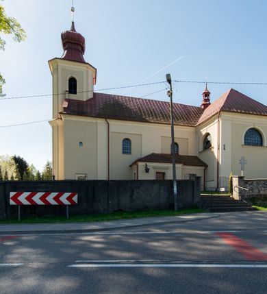 Zdjęcie nr 19: Kościół murowany, jednonawowy, z wieżą częściowo wtopioną w elewację zachodnią składający się z nawy, transeptu, zakrystii od północy z mieszczącym się na piętrze skarbcem i przystawionej od wschodu wieżyczki klatki schodowej oraz kruchty od południa. Prezbiterium dwuprzęsłowe, zamknięte trójbocznie. Nawa główna podzielona masywnymi opilastrowanymi filarami. Sklepienie prezbiterium i nawy kolebkowe z lunetami, skrzyżowania z transeptem. Od południa chór muzyczny mieszczący się między pierwszymi filarami i powyżej kruchty wejściowej. W prezbiterium okna w każdym przęśle, po każdej stronie nawy po dwa, w transepcie po trzy, w kruchcie dwa. Główne wejście od zachodu, kolejne do zakrystii i od południa. Ściany i sklepienia kościoła pokrywa polichromia złożona z geometryzujących dekoracji floralnych. 
Wschodnią elewację frontową kościoła tworzy trójosiowa, wieżowa fasada. Oś kompozycji stanowi wysunięta ryzalitowo dwukondygnacyjna wieża ze ściętymi narożami, które zaakcentowane są poprzez pilastry. Ściana czołowa wieży wypełniona w pierwszej kondygnacji wklęsłą płyciną, z portalem o wykroju prostokątnym, z odcinkiem gzymsu w zwieńczeniu. Ponad nim prostokątne okno zakończone łukiem pełnym. Kondygnacje rozdzielone za pomocą masywnego gzymsu. Druga kondygnacja wieży wypełniona analogicznie prostokątną płyciną, w którą wkomponowany jest wypukły panel w kształcie leżącego prostokąta. Nad nim okno o obramieniu i wykroju identycznym jak w kondygnacji niższej. Całość zwieńczona za pomocą gzymsu podokapowego i baniastego hełmu wieżowego o ściętych narożach, na które nałożona jest kopułka w formie cebulastej. Osie boczne cofnięte w stosunku do wysuniętej wieży i zrytmizowane podziałem ramowym. Tak jak w osi głównej pierwsza kondygnacja wypełniona jest wklęsłą płyciną w formie wydłużonego, stojącego prostokąta. Nad gzymsem trójkątny spływ przysłonięty wieżą. Elewacje boczne i tylna ukształtowane jednorodnie. Zrytmizowane podziałem ramowym i przeprute oknami umieszczonymi w prostokątnych płycinach. Ramiona transeptu oraz prezbiterium zrytmizowane są za pomocą pilastrów załamanych na narożach. Od południa do korpusu przylega niska kruchta. Prowadzi do niej wejście o wykroju prostokątnym z profilowanym w tynku portalem i z odcinkiem gzymsu w zwieńczeniu. Od północy pomiędzy prezbiterium, a ramieniem transeptu wprowadzona została piętrowa przybudówka zakrystii. W elewacji tej partii kościoła brak jest znaczących podziałów. Okna i drzwi tam się znajdujące mają formę stojącego prostokąta i pozbawione są jakichkolwiek obramień. Kościół pokryty dwuspadowym, jednokalenicowym dachem, nad zakrystią i kruchtami umieszczono daszki dwuspadowe. Wieża nakryta jest hełmem cebulastym. Całość pokryta została malowaną blachą.
