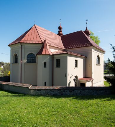 Zdjęcie nr 16: Kościół murowany, jednonawowy, z wieżą częściowo wtopioną w elewację zachodnią składający się z nawy, transeptu, zakrystii od północy z mieszczącym się na piętrze skarbcem i przystawionej od wschodu wieżyczki klatki schodowej oraz kruchty od południa. Prezbiterium dwuprzęsłowe, zamknięte trójbocznie. Nawa główna podzielona masywnymi opilastrowanymi filarami. Sklepienie prezbiterium i nawy kolebkowe z lunetami, skrzyżowania z transeptem. Od południa chór muzyczny mieszczący się między pierwszymi filarami i powyżej kruchty wejściowej. W prezbiterium okna w każdym przęśle, po każdej stronie nawy po dwa, w transepcie po trzy, w kruchcie dwa. Główne wejście od zachodu, kolejne do zakrystii i od południa. Ściany i sklepienia kościoła pokrywa polichromia złożona z geometryzujących dekoracji floralnych. 
Wschodnią elewację frontową kościoła tworzy trójosiowa, wieżowa fasada. Oś kompozycji stanowi wysunięta ryzalitowo dwukondygnacyjna wieża ze ściętymi narożami, które zaakcentowane są poprzez pilastry. Ściana czołowa wieży wypełniona w pierwszej kondygnacji wklęsłą płyciną, z portalem o wykroju prostokątnym, z odcinkiem gzymsu w zwieńczeniu. Ponad nim prostokątne okno zakończone łukiem pełnym. Kondygnacje rozdzielone za pomocą masywnego gzymsu. Druga kondygnacja wieży wypełniona analogicznie prostokątną płyciną, w którą wkomponowany jest wypukły panel w kształcie leżącego prostokąta. Nad nim okno o obramieniu i wykroju identycznym jak w kondygnacji niższej. Całość zwieńczona za pomocą gzymsu podokapowego i baniastego hełmu wieżowego o ściętych narożach, na które nałożona jest kopułka w formie cebulastej. Osie boczne cofnięte w stosunku do wysuniętej wieży i zrytmizowane podziałem ramowym. Tak jak w osi głównej pierwsza kondygnacja wypełniona jest wklęsłą płyciną w formie wydłużonego, stojącego prostokąta. Nad gzymsem trójkątny spływ przysłonięty wieżą. Elewacje boczne i tylna ukształtowane jednorodnie. Zrytmizowane podziałem ramowym i przeprute oknami umieszczonymi w prostokątnych płycinach. Ramiona transeptu oraz prezbiterium zrytmizowane są za pomocą pilastrów załamanych na narożach. Od południa do korpusu przylega niska kruchta. Prowadzi do niej wejście o wykroju prostokątnym z profilowanym w tynku portalem i z odcinkiem gzymsu w zwieńczeniu. Od północy pomiędzy prezbiterium, a ramieniem transeptu wprowadzona została piętrowa przybudówka zakrystii. W elewacji tej partii kościoła brak jest znaczących podziałów. Okna i drzwi tam się znajdujące mają formę stojącego prostokąta i pozbawione są jakichkolwiek obramień. Kościół pokryty dwuspadowym, jednokalenicowym dachem, nad zakrystią i kruchtami umieszczono daszki dwuspadowe. Wieża nakryta jest hełmem cebulastym. Całość pokryta została malowaną blachą.
