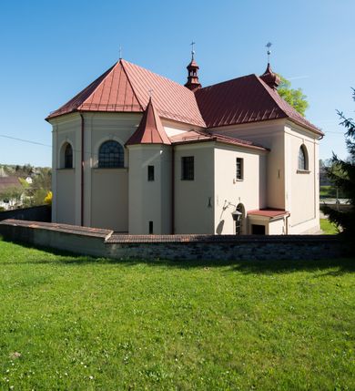 Zdjęcie nr 13: Kościół murowany, jednonawowy, z wieżą częściowo wtopioną w elewację zachodnią składający się z nawy, transeptu, zakrystii od północy z mieszczącym się na piętrze skarbcem i przystawionej od wschodu wieżyczki klatki schodowej oraz kruchty od południa. Prezbiterium dwuprzęsłowe, zamknięte trójbocznie. Nawa główna podzielona masywnymi opilastrowanymi filarami. Sklepienie prezbiterium i nawy kolebkowe z lunetami, skrzyżowania z transeptem. Od południa chór muzyczny mieszczący się między pierwszymi filarami i powyżej kruchty wejściowej. W prezbiterium okna w każdym przęśle, po każdej stronie nawy po dwa, w transepcie po trzy, w kruchcie dwa. Główne wejście od zachodu, kolejne do zakrystii i od południa. Ściany i sklepienia kościoła pokrywa polichromia złożona z geometryzujących dekoracji floralnych. 
Wschodnią elewację frontową kościoła tworzy trójosiowa, wieżowa fasada. Oś kompozycji stanowi wysunięta ryzalitowo dwukondygnacyjna wieża ze ściętymi narożami, które zaakcentowane są poprzez pilastry. Ściana czołowa wieży wypełniona w pierwszej kondygnacji wklęsłą płyciną, z portalem o wykroju prostokątnym, z odcinkiem gzymsu w zwieńczeniu. Ponad nim prostokątne okno zakończone łukiem pełnym. Kondygnacje rozdzielone za pomocą masywnego gzymsu. Druga kondygnacja wieży wypełniona analogicznie prostokątną płyciną, w którą wkomponowany jest wypukły panel w kształcie leżącego prostokąta. Nad nim okno o obramieniu i wykroju identycznym jak w kondygnacji niższej. Całość zwieńczona za pomocą gzymsu podokapowego i baniastego hełmu wieżowego o ściętych narożach, na które nałożona jest kopułka w formie cebulastej. Osie boczne cofnięte w stosunku do wysuniętej wieży i zrytmizowane podziałem ramowym. Tak jak w osi głównej pierwsza kondygnacja wypełniona jest wklęsłą płyciną w formie wydłużonego, stojącego prostokąta. Nad gzymsem trójkątny spływ przysłonięty wieżą. Elewacje boczne i tylna ukształtowane jednorodnie. Zrytmizowane podziałem ramowym i przeprute oknami umieszczonymi w prostokątnych płycinach. Ramiona transeptu oraz prezbiterium zrytmizowane są za pomocą pilastrów załamanych na narożach. Od południa do korpusu przylega niska kruchta. Prowadzi do niej wejście o wykroju prostokątnym z profilowanym w tynku portalem i z odcinkiem gzymsu w zwieńczeniu. Od północy pomiędzy prezbiterium, a ramieniem transeptu wprowadzona została piętrowa przybudówka zakrystii. W elewacji tej partii kościoła brak jest znaczących podziałów. Okna i drzwi tam się znajdujące mają formę stojącego prostokąta i pozbawione są jakichkolwiek obramień. Kościół pokryty dwuspadowym, jednokalenicowym dachem, nad zakrystią i kruchtami umieszczono daszki dwuspadowe. Wieża nakryta jest hełmem cebulastym. Całość pokryta została malowaną blachą.
