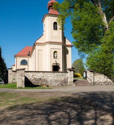 Zdjęcie nr 6: Kościół murowany, jednonawowy, z wieżą częściowo wtopioną w elewację zachodnią składający się z nawy, transeptu, zakrystii od północy z mieszczącym się na piętrze skarbcem i przystawionej od wschodu wieżyczki klatki schodowej oraz kruchty od południa. Prezbiterium dwuprzęsłowe, zamknięte trójbocznie. Nawa główna podzielona masywnymi opilastrowanymi filarami. Sklepienie prezbiterium i nawy kolebkowe z lunetami, skrzyżowania z transeptem. Od południa chór muzyczny mieszczący się między pierwszymi filarami i powyżej kruchty wejściowej. W prezbiterium okna w każdym przęśle, po każdej stronie nawy po dwa, w transepcie po trzy, w kruchcie dwa. Główne wejście od zachodu, kolejne do zakrystii i od południa. Ściany i sklepienia kościoła pokrywa polichromia złożona z geometryzujących dekoracji floralnych. 
Wschodnią elewację frontową kościoła tworzy trójosiowa, wieżowa fasada. Oś kompozycji stanowi wysunięta ryzalitowo dwukondygnacyjna wieża ze ściętymi narożami, które zaakcentowane są poprzez pilastry. Ściana czołowa wieży wypełniona w pierwszej kondygnacji wklęsłą płyciną, z portalem o wykroju prostokątnym, z odcinkiem gzymsu w zwieńczeniu. Ponad nim prostokątne okno zakończone łukiem pełnym. Kondygnacje rozdzielone za pomocą masywnego gzymsu. Druga kondygnacja wieży wypełniona analogicznie prostokątną płyciną, w którą wkomponowany jest wypukły panel w kształcie leżącego prostokąta. Nad nim okno o obramieniu i wykroju identycznym jak w kondygnacji niższej. Całość zwieńczona za pomocą gzymsu podokapowego i baniastego hełmu wieżowego o ściętych narożach, na które nałożona jest kopułka w formie cebulastej. Osie boczne cofnięte w stosunku do wysuniętej wieży i zrytmizowane podziałem ramowym. Tak jak w osi głównej pierwsza kondygnacja wypełniona jest wklęsłą płyciną w formie wydłużonego, stojącego prostokąta. Nad gzymsem trójkątny spływ przysłonięty wieżą. Elewacje boczne i tylna ukształtowane jednorodnie. Zrytmizowane podziałem ramowym i przeprute oknami umieszczonymi w prostokątnych płycinach. Ramiona transeptu oraz prezbiterium zrytmizowane są za pomocą pilastrów załamanych na narożach. Od południa do korpusu przylega niska kruchta. Prowadzi do niej wejście o wykroju prostokątnym z profilowanym w tynku portalem i z odcinkiem gzymsu w zwieńczeniu. Od północy pomiędzy prezbiterium, a ramieniem transeptu wprowadzona została piętrowa przybudówka zakrystii. W elewacji tej partii kościoła brak jest znaczących podziałów. Okna i drzwi tam się znajdujące mają formę stojącego prostokąta i pozbawione są jakichkolwiek obramień. Kościół pokryty dwuspadowym, jednokalenicowym dachem, nad zakrystią i kruchtami umieszczono daszki dwuspadowe. Wieża nakryta jest hełmem cebulastym. Całość pokryta została malowaną blachą.
