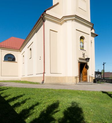 Zdjęcie nr 11: Kościół murowany, jednonawowy, z wieżą częściowo wtopioną w elewację zachodnią składający się z nawy, transeptu, zakrystii od północy z mieszczącym się na piętrze skarbcem i przystawionej od wschodu wieżyczki klatki schodowej oraz kruchty od południa. Prezbiterium dwuprzęsłowe, zamknięte trójbocznie. Nawa główna podzielona masywnymi opilastrowanymi filarami. Sklepienie prezbiterium i nawy kolebkowe z lunetami, skrzyżowania z transeptem. Od południa chór muzyczny mieszczący się między pierwszymi filarami i powyżej kruchty wejściowej. W prezbiterium okna w każdym przęśle, po każdej stronie nawy po dwa, w transepcie po trzy, w kruchcie dwa. Główne wejście od zachodu, kolejne do zakrystii i od południa. Ściany i sklepienia kościoła pokrywa polichromia złożona z geometryzujących dekoracji floralnych. 
Wschodnią elewację frontową kościoła tworzy trójosiowa, wieżowa fasada. Oś kompozycji stanowi wysunięta ryzalitowo dwukondygnacyjna wieża ze ściętymi narożami, które zaakcentowane są poprzez pilastry. Ściana czołowa wieży wypełniona w pierwszej kondygnacji wklęsłą płyciną, z portalem o wykroju prostokątnym, z odcinkiem gzymsu w zwieńczeniu. Ponad nim prostokątne okno zakończone łukiem pełnym. Kondygnacje rozdzielone za pomocą masywnego gzymsu. Druga kondygnacja wieży wypełniona analogicznie prostokątną płyciną, w którą wkomponowany jest wypukły panel w kształcie leżącego prostokąta. Nad nim okno o obramieniu i wykroju identycznym jak w kondygnacji niższej. Całość zwieńczona za pomocą gzymsu podokapowego i baniastego hełmu wieżowego o ściętych narożach, na które nałożona jest kopułka w formie cebulastej. Osie boczne cofnięte w stosunku do wysuniętej wieży i zrytmizowane podziałem ramowym. Tak jak w osi głównej pierwsza kondygnacja wypełniona jest wklęsłą płyciną w formie wydłużonego, stojącego prostokąta. Nad gzymsem trójkątny spływ przysłonięty wieżą. Elewacje boczne i tylna ukształtowane jednorodnie. Zrytmizowane podziałem ramowym i przeprute oknami umieszczonymi w prostokątnych płycinach. Ramiona transeptu oraz prezbiterium zrytmizowane są za pomocą pilastrów załamanych na narożach. Od południa do korpusu przylega niska kruchta. Prowadzi do niej wejście o wykroju prostokątnym z profilowanym w tynku portalem i z odcinkiem gzymsu w zwieńczeniu. Od północy pomiędzy prezbiterium, a ramieniem transeptu wprowadzona została piętrowa przybudówka zakrystii. W elewacji tej partii kościoła brak jest znaczących podziałów. Okna i drzwi tam się znajdujące mają formę stojącego prostokąta i pozbawione są jakichkolwiek obramień. Kościół pokryty dwuspadowym, jednokalenicowym dachem, nad zakrystią i kruchtami umieszczono daszki dwuspadowe. Wieża nakryta jest hełmem cebulastym. Całość pokryta została malowaną blachą.
