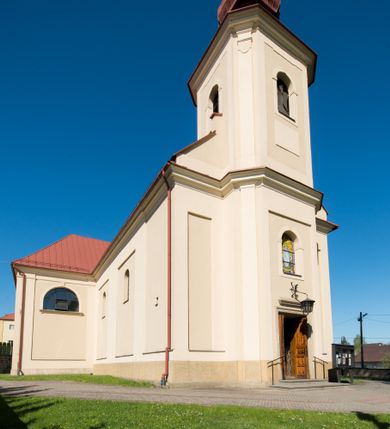 Zdjęcie nr 9: Kościół murowany, jednonawowy, z wieżą częściowo wtopioną w elewację zachodnią składający się z nawy, transeptu, zakrystii od północy z mieszczącym się na piętrze skarbcem i przystawionej od wschodu wieżyczki klatki schodowej oraz kruchty od południa. Prezbiterium dwuprzęsłowe, zamknięte trójbocznie. Nawa główna podzielona masywnymi opilastrowanymi filarami. Sklepienie prezbiterium i nawy kolebkowe z lunetami, skrzyżowania z transeptem. Od południa chór muzyczny mieszczący się między pierwszymi filarami i powyżej kruchty wejściowej. W prezbiterium okna w każdym przęśle, po każdej stronie nawy po dwa, w transepcie po trzy, w kruchcie dwa. Główne wejście od zachodu, kolejne do zakrystii i od południa. Ściany i sklepienia kościoła pokrywa polichromia złożona z geometryzujących dekoracji floralnych. 
Wschodnią elewację frontową kościoła tworzy trójosiowa, wieżowa fasada. Oś kompozycji stanowi wysunięta ryzalitowo dwukondygnacyjna wieża ze ściętymi narożami, które zaakcentowane są poprzez pilastry. Ściana czołowa wieży wypełniona w pierwszej kondygnacji wklęsłą płyciną, z portalem o wykroju prostokątnym, z odcinkiem gzymsu w zwieńczeniu. Ponad nim prostokątne okno zakończone łukiem pełnym. Kondygnacje rozdzielone za pomocą masywnego gzymsu. Druga kondygnacja wieży wypełniona analogicznie prostokątną płyciną, w którą wkomponowany jest wypukły panel w kształcie leżącego prostokąta. Nad nim okno o obramieniu i wykroju identycznym jak w kondygnacji niższej. Całość zwieńczona za pomocą gzymsu podokapowego i baniastego hełmu wieżowego o ściętych narożach, na które nałożona jest kopułka w formie cebulastej. Osie boczne cofnięte w stosunku do wysuniętej wieży i zrytmizowane podziałem ramowym. Tak jak w osi głównej pierwsza kondygnacja wypełniona jest wklęsłą płyciną w formie wydłużonego, stojącego prostokąta. Nad gzymsem trójkątny spływ przysłonięty wieżą. Elewacje boczne i tylna ukształtowane jednorodnie. Zrytmizowane podziałem ramowym i przeprute oknami umieszczonymi w prostokątnych płycinach. Ramiona transeptu oraz prezbiterium zrytmizowane są za pomocą pilastrów załamanych na narożach. Od południa do korpusu przylega niska kruchta. Prowadzi do niej wejście o wykroju prostokątnym z profilowanym w tynku portalem i z odcinkiem gzymsu w zwieńczeniu. Od północy pomiędzy prezbiterium, a ramieniem transeptu wprowadzona została piętrowa przybudówka zakrystii. W elewacji tej partii kościoła brak jest znaczących podziałów. Okna i drzwi tam się znajdujące mają formę stojącego prostokąta i pozbawione są jakichkolwiek obramień. Kościół pokryty dwuspadowym, jednokalenicowym dachem, nad zakrystią i kruchtami umieszczono daszki dwuspadowe. Wieża nakryta jest hełmem cebulastym. Całość pokryta została malowaną blachą.
