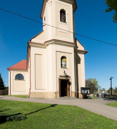 Zdjęcie nr 10: Kościół murowany, jednonawowy, z wieżą częściowo wtopioną w elewację zachodnią składający się z nawy, transeptu, zakrystii od północy z mieszczącym się na piętrze skarbcem i przystawionej od wschodu wieżyczki klatki schodowej oraz kruchty od południa. Prezbiterium dwuprzęsłowe, zamknięte trójbocznie. Nawa główna podzielona masywnymi opilastrowanymi filarami. Sklepienie prezbiterium i nawy kolebkowe z lunetami, skrzyżowania z transeptem. Od południa chór muzyczny mieszczący się między pierwszymi filarami i powyżej kruchty wejściowej. W prezbiterium okna w każdym przęśle, po każdej stronie nawy po dwa, w transepcie po trzy, w kruchcie dwa. Główne wejście od zachodu, kolejne do zakrystii i od południa. Ściany i sklepienia kościoła pokrywa polichromia złożona z geometryzujących dekoracji floralnych. 
Wschodnią elewację frontową kościoła tworzy trójosiowa, wieżowa fasada. Oś kompozycji stanowi wysunięta ryzalitowo dwukondygnacyjna wieża ze ściętymi narożami, które zaakcentowane są poprzez pilastry. Ściana czołowa wieży wypełniona w pierwszej kondygnacji wklęsłą płyciną, z portalem o wykroju prostokątnym, z odcinkiem gzymsu w zwieńczeniu. Ponad nim prostokątne okno zakończone łukiem pełnym. Kondygnacje rozdzielone za pomocą masywnego gzymsu. Druga kondygnacja wieży wypełniona analogicznie prostokątną płyciną, w którą wkomponowany jest wypukły panel w kształcie leżącego prostokąta. Nad nim okno o obramieniu i wykroju identycznym jak w kondygnacji niższej. Całość zwieńczona za pomocą gzymsu podokapowego i baniastego hełmu wieżowego o ściętych narożach, na które nałożona jest kopułka w formie cebulastej. Osie boczne cofnięte w stosunku do wysuniętej wieży i zrytmizowane podziałem ramowym. Tak jak w osi głównej pierwsza kondygnacja wypełniona jest wklęsłą płyciną w formie wydłużonego, stojącego prostokąta. Nad gzymsem trójkątny spływ przysłonięty wieżą. Elewacje boczne i tylna ukształtowane jednorodnie. Zrytmizowane podziałem ramowym i przeprute oknami umieszczonymi w prostokątnych płycinach. Ramiona transeptu oraz prezbiterium zrytmizowane są za pomocą pilastrów załamanych na narożach. Od południa do korpusu przylega niska kruchta. Prowadzi do niej wejście o wykroju prostokątnym z profilowanym w tynku portalem i z odcinkiem gzymsu w zwieńczeniu. Od północy pomiędzy prezbiterium, a ramieniem transeptu wprowadzona została piętrowa przybudówka zakrystii. W elewacji tej partii kościoła brak jest znaczących podziałów. Okna i drzwi tam się znajdujące mają formę stojącego prostokąta i pozbawione są jakichkolwiek obramień. Kościół pokryty dwuspadowym, jednokalenicowym dachem, nad zakrystią i kruchtami umieszczono daszki dwuspadowe. Wieża nakryta jest hełmem cebulastym. Całość pokryta została malowaną blachą.
