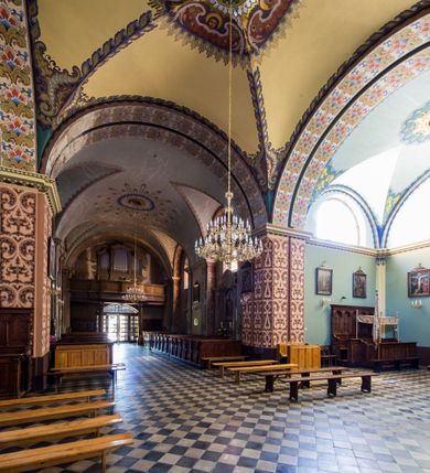 Zdjęcie nr 28: Kościół murowany, jednonawowy, z wieżą częściowo wtopioną w elewację zachodnią składający się z nawy, transeptu, zakrystii od północy z mieszczącym się na piętrze skarbcem i przystawionej od wschodu wieżyczki klatki schodowej oraz kruchty od południa. Prezbiterium dwuprzęsłowe, zamknięte trójbocznie. Nawa główna podzielona masywnymi opilastrowanymi filarami. Sklepienie prezbiterium i nawy kolebkowe z lunetami, skrzyżowania z transeptem. Od południa chór muzyczny mieszczący się między pierwszymi filarami i powyżej kruchty wejściowej. W prezbiterium okna w każdym przęśle, po każdej stronie nawy po dwa, w transepcie po trzy, w kruchcie dwa. Główne wejście od zachodu, kolejne do zakrystii i od południa. Ściany i sklepienia kościoła pokrywa polichromia złożona z geometryzujących dekoracji floralnych. 
Wschodnią elewację frontową kościoła tworzy trójosiowa, wieżowa fasada. Oś kompozycji stanowi wysunięta ryzalitowo dwukondygnacyjna wieża ze ściętymi narożami, które zaakcentowane są poprzez pilastry. Ściana czołowa wieży wypełniona w pierwszej kondygnacji wklęsłą płyciną, z portalem o wykroju prostokątnym, z odcinkiem gzymsu w zwieńczeniu. Ponad nim prostokątne okno zakończone łukiem pełnym. Kondygnacje rozdzielone za pomocą masywnego gzymsu. Druga kondygnacja wieży wypełniona analogicznie prostokątną płyciną, w którą wkomponowany jest wypukły panel w kształcie leżącego prostokąta. Nad nim okno o obramieniu i wykroju identycznym jak w kondygnacji niższej. Całość zwieńczona za pomocą gzymsu podokapowego i baniastego hełmu wieżowego o ściętych narożach, na które nałożona jest kopułka w formie cebulastej. Osie boczne cofnięte w stosunku do wysuniętej wieży i zrytmizowane podziałem ramowym. Tak jak w osi głównej pierwsza kondygnacja wypełniona jest wklęsłą płyciną w formie wydłużonego, stojącego prostokąta. Nad gzymsem trójkątny spływ przysłonięty wieżą. Elewacje boczne i tylna ukształtowane jednorodnie. Zrytmizowane podziałem ramowym i przeprute oknami umieszczonymi w prostokątnych płycinach. Ramiona transeptu oraz prezbiterium zrytmizowane są za pomocą pilastrów załamanych na narożach. Od południa do korpusu przylega niska kruchta. Prowadzi do niej wejście o wykroju prostokątnym z profilowanym w tynku portalem i z odcinkiem gzymsu w zwieńczeniu. Od północy pomiędzy prezbiterium, a ramieniem transeptu wprowadzona została piętrowa przybudówka zakrystii. W elewacji tej partii kościoła brak jest znaczących podziałów. Okna i drzwi tam się znajdujące mają formę stojącego prostokąta i pozbawione są jakichkolwiek obramień. Kościół pokryty dwuspadowym, jednokalenicowym dachem, nad zakrystią i kruchtami umieszczono daszki dwuspadowe. Wieża nakryta jest hełmem cebulastym. Całość pokryta została malowaną blachą.
