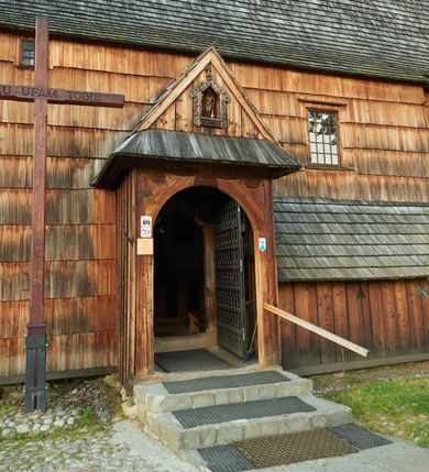 Zdjęcie nr 18: Orientowany, jednoprzestrzenny, nawa na rzucie prostokąta, z węższym, prostokątnym prezbiterium, przy którym od północy wąska zakrystia. Od zachodu przy nawie wieża na rzucie kwadratu, od południa kruchta. Wnętrze nakryte stropem, w nawie z zaskrzynieniem. Portale zachodni i do zakrystii ostrołukowe, fazowane; portal południowy zamknięty łukiem kotarowym. Okna prostokątne, w prezbiterium od południa okno bliźnie, od wschodu zamknięte łukiem kotarowym.  Wokół podcienia, obecnie zaszalowane. Więźba dachowa jętkowa, ze znakami montażowymi.  Dach nad nawą i prezbiterium jednokalenicowy, dwuspadowy, nad nawą z połaciami przedłużonymi na zaskrzynienia i od północy nad zakrystię. Na kalenicy wieżyczka na sygnaturkę z baniastym hełmem.  Wieża o ścianach pochyłych, z nadwieszoną izbicą, zwieńczona ostrosłupowym hełmem. Wokół kościoła ogrodzenie belek układanych na zrąb, z dwiema bramkami. 