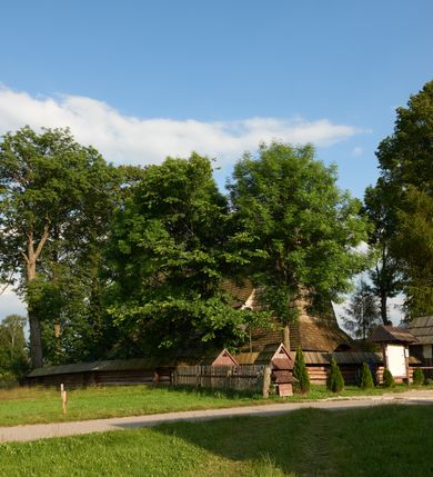Zdjęcie nr 6: Orientowany, jednoprzestrzenny, nawa na rzucie prostokąta, z węższym, prostokątnym prezbiterium, przy którym od północy wąska zakrystia. Od zachodu przy nawie wieża na rzucie kwadratu, od południa kruchta. Wnętrze nakryte stropem, w nawie z zaskrzynieniem. Portale zachodni i do zakrystii ostrołukowe, fazowane; portal południowy zamknięty łukiem kotarowym. Okna prostokątne, w prezbiterium od południa okno bliźnie, od wschodu zamknięte łukiem kotarowym.  Wokół podcienia, obecnie zaszalowane. Więźba dachowa jętkowa, ze znakami montażowymi.  Dach nad nawą i prezbiterium jednokalenicowy, dwuspadowy, nad nawą z połaciami przedłużonymi na zaskrzynienia i od północy nad zakrystię. Na kalenicy wieżyczka na sygnaturkę z baniastym hełmem.  Wieża o ścianach pochyłych, z nadwieszoną izbicą, zwieńczona ostrosłupowym hełmem. Wokół kościoła ogrodzenie belek układanych na zrąb, z dwiema bramkami. 