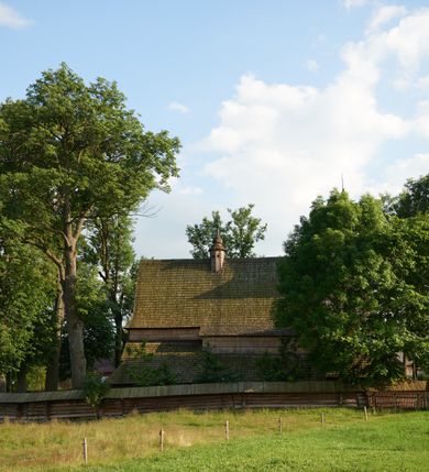 Zdjęcie nr 7: Orientowany, jednoprzestrzenny, nawa na rzucie prostokąta, z węższym, prostokątnym prezbiterium, przy którym od północy wąska zakrystia. Od zachodu przy nawie wieża na rzucie kwadratu, od południa kruchta. Wnętrze nakryte stropem, w nawie z zaskrzynieniem. Portale zachodni i do zakrystii ostrołukowe, fazowane; portal południowy zamknięty łukiem kotarowym. Okna prostokątne, w prezbiterium od południa okno bliźnie, od wschodu zamknięte łukiem kotarowym.  Wokół podcienia, obecnie zaszalowane. Więźba dachowa jętkowa, ze znakami montażowymi.  Dach nad nawą i prezbiterium jednokalenicowy, dwuspadowy, nad nawą z połaciami przedłużonymi na zaskrzynienia i od północy nad zakrystię. Na kalenicy wieżyczka na sygnaturkę z baniastym hełmem.  Wieża o ścianach pochyłych, z nadwieszoną izbicą, zwieńczona ostrosłupowym hełmem. Wokół kościoła ogrodzenie belek układanych na zrąb, z dwiema bramkami. 