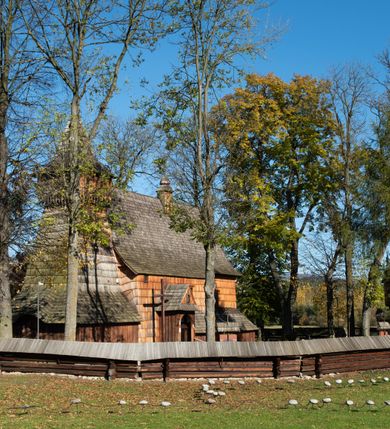 Zdjęcie nr 20: Orientowany, jednoprzestrzenny, nawa na rzucie prostokąta, z węższym, prostokątnym prezbiterium, przy którym od północy wąska zakrystia. Od zachodu przy nawie wieża na rzucie kwadratu, od południa kruchta. Wnętrze nakryte stropem, w nawie z zaskrzynieniem. Portale zachodni i do zakrystii ostrołukowe, fazowane; portal południowy zamknięty łukiem kotarowym. Okna prostokątne, w prezbiterium od południa okno bliźnie, od wschodu zamknięte łukiem kotarowym.  Wokół podcienia, obecnie zaszalowane. Więźba dachowa jętkowa, ze znakami montażowymi.  Dach nad nawą i prezbiterium jednokalenicowy, dwuspadowy, nad nawą z połaciami przedłużonymi na zaskrzynienia i od północy nad zakrystię. Na kalenicy wieżyczka na sygnaturkę z baniastym hełmem.  Wieża o ścianach pochyłych, z nadwieszoną izbicą, zwieńczona ostrosłupowym hełmem. Wokół kościoła ogrodzenie belek układanych na zrąb, z dwiema bramkami. 