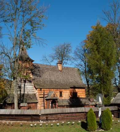 Zdjęcie nr 22: Orientowany, jednoprzestrzenny, nawa na rzucie prostokąta, z węższym, prostokątnym prezbiterium, przy którym od północy wąska zakrystia. Od zachodu przy nawie wieża na rzucie kwadratu, od południa kruchta. Wnętrze nakryte stropem, w nawie z zaskrzynieniem. Portale zachodni i do zakrystii ostrołukowe, fazowane; portal południowy zamknięty łukiem kotarowym. Okna prostokątne, w prezbiterium od południa okno bliźnie, od wschodu zamknięte łukiem kotarowym.  Wokół podcienia, obecnie zaszalowane. Więźba dachowa jętkowa, ze znakami montażowymi.  Dach nad nawą i prezbiterium jednokalenicowy, dwuspadowy, nad nawą z połaciami przedłużonymi na zaskrzynienia i od północy nad zakrystię. Na kalenicy wieżyczka na sygnaturkę z baniastym hełmem.  Wieża o ścianach pochyłych, z nadwieszoną izbicą, zwieńczona ostrosłupowym hełmem. Wokół kościoła ogrodzenie belek układanych na zrąb, z dwiema bramkami. 