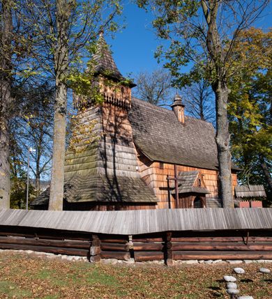 Zdjęcie nr 5: Orientowany, jednoprzestrzenny, nawa na rzucie prostokąta, z węższym, prostokątnym prezbiterium, przy którym od północy wąska zakrystia. Od zachodu przy nawie wieża na rzucie kwadratu, od południa kruchta. Wnętrze nakryte stropem, w nawie z zaskrzynieniem. Portale zachodni i do zakrystii ostrołukowe, fazowane; portal południowy zamknięty łukiem kotarowym. Okna prostokątne, w prezbiterium od południa okno bliźnie, od wschodu zamknięte łukiem kotarowym.  Wokół podcienia, obecnie zaszalowane. Więźba dachowa jętkowa, ze znakami montażowymi.  Dach nad nawą i prezbiterium jednokalenicowy, dwuspadowy, nad nawą z połaciami przedłużonymi na zaskrzynienia i od północy nad zakrystię. Na kalenicy wieżyczka na sygnaturkę z baniastym hełmem.  Wieża o ścianach pochyłych, z nadwieszoną izbicą, zwieńczona ostrosłupowym hełmem. Wokół kościoła ogrodzenie belek układanych na zrąb, z dwiema bramkami. 