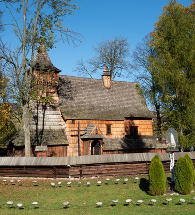 Zdjęcie nr 3: Orientowany, jednoprzestrzenny, nawa na rzucie prostokąta, z węższym, prostokątnym prezbiterium, przy którym od północy wąska zakrystia. Od zachodu przy nawie wieża na rzucie kwadratu, od południa kruchta. Wnętrze nakryte stropem, w nawie z zaskrzynieniem. Portale zachodni i do zakrystii ostrołukowe, fazowane; portal południowy zamknięty łukiem kotarowym. Okna prostokątne, w prezbiterium od południa okno bliźnie, od wschodu zamknięte łukiem kotarowym.  Wokół podcienia, obecnie zaszalowane. Więźba dachowa jętkowa, ze znakami montażowymi.  Dach nad nawą i prezbiterium jednokalenicowy, dwuspadowy, nad nawą z połaciami przedłużonymi na zaskrzynienia i od północy nad zakrystię. Na kalenicy wieżyczka na sygnaturkę z baniastym hełmem.  Wieża o ścianach pochyłych, z nadwieszoną izbicą, zwieńczona ostrosłupowym hełmem. Wokół kościoła ogrodzenie belek układanych na zrąb, z dwiema bramkami. 