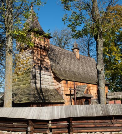 Zdjęcie nr 4: Orientowany, jednoprzestrzenny, nawa na rzucie prostokąta, z węższym, prostokątnym prezbiterium, przy którym od północy wąska zakrystia. Od zachodu przy nawie wieża na rzucie kwadratu, od południa kruchta. Wnętrze nakryte stropem, w nawie z zaskrzynieniem. Portale zachodni i do zakrystii ostrołukowe, fazowane; portal południowy zamknięty łukiem kotarowym. Okna prostokątne, w prezbiterium od południa okno bliźnie, od wschodu zamknięte łukiem kotarowym.  Wokół podcienia, obecnie zaszalowane. Więźba dachowa jętkowa, ze znakami montażowymi.  Dach nad nawą i prezbiterium jednokalenicowy, dwuspadowy, nad nawą z połaciami przedłużonymi na zaskrzynienia i od północy nad zakrystię. Na kalenicy wieżyczka na sygnaturkę z baniastym hełmem.  Wieża o ścianach pochyłych, z nadwieszoną izbicą, zwieńczona ostrosłupowym hełmem. Wokół kościoła ogrodzenie belek układanych na zrąb, z dwiema bramkami. 